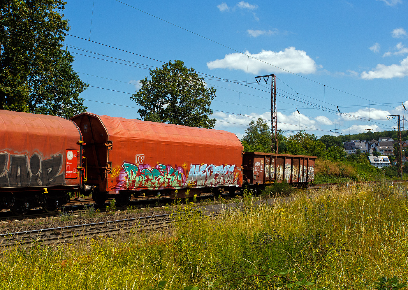 2-achsiger Flachwagen mit öffnungsfähigem Planendach und Stoßverzehreinrichtung zum Schutz vor Rangierstößen, 41 80 3384 088-5 D-DB, der Gattung Kijls 450, der DB Cargo AG (leider wie viele solcher Wagen sehr beschmiert), am 11 Juni 2024 im Zugverband bei einer Zugdurchfahrt durch Rudersdorf (Kreis Siegen) in Richtung Siegen bzw. Kreuztal.

Der Wagen wurde 2001 von ALSTOM LHB (vormals Linke-Hofmann-Busch GmbH in Salzgitter-Watenstedt gebaut.

Der Wagen lässt an sich einiges abprallen, er ist mit einer Stoßverzehreinrichtung zum Schutz vor Rangierstößen ausgestattet. So eignet sich dieser Wagen besonders zum Transport von stoßempfindlichen Gütern (z. B. Komponenten für die Automobilindustrie, Motoren, Getriebe, Maschinen, Trafos). Aufgrund des geschlossenen und verriegelten Planendachs gewährt er auch Schutz für nässeempfindliche Güter. Zusätzliche Zug-Spannsysteme gewährleisten eine schnellere Ladesicherung. Bei einer Ladelänge von über 14 Meter bietet der Wagen einen Laderaum von 109 m³.

Der Wagen besitzt einen unter dem Wagenkasten durchlaufenden, hydraulischen Stoßbalken, der die im Wagen befindlichen Güter weitgehend vor Rangierstößen schützt. Dadurch wird die auf die Ladung wirkende rechnerische Beschleunigung bei Auflaufgeschwindigkeiten bis 9 km/h auf 1 g (9,81 m/s²) begrenzt.

Die Stirnwände bestehen aus zwei schrägen Stirnwandsäulen, zwei Querträgern und einem Rahmen, der gleichzeitig das Dichtsystem aufnimmt. Die Dicke der Beblechung beträgt 2 mm. An den Stirnwänden sind die robusten 4-Punkt-Zentralverriegelungen angeordnet, mit der das Planendach zuverlässig gesichert werden kann. Die Betätigungseinrichtungen sind so angeordnet, dass das Ent- und Verriegeln des Planendaches sowohl vom Erdboden als auch von einer Rampe aus möglich ist. Die insgesamt 4 Verriegelungshaken (je Längseite) einschließlich der beiden Betätigungshebel sind über drehbar gelagerte Wellen untereinander verbunden. Dadurch ist ein Betätigen der Zentralverriegelung von jeder Wagenseite aus möglich.

Das Planendach besteht aus 2 End- und 10 Mittelspriegeln mit einer PVC-Beschichteten Gewebeplane. Die Spriegel ruhen auf Laufwagen, die wiederum selbst auf an den Langträgern angeordneten Fahrschienen stehen. Unter die Fahrschienen greifende Rollen an den Laufwagen wirken als Sicherungen und verhindern so ein Abheben der Hauben bei Auflaufstößen oder Windbelastung.

Das Planendach lässt sich mit geringem Kraftaufwand jeweils zu einem Wagenende hin verfahren und so weit zusammenschieben, dass ca. 3/4 der Ladelänge zur uneingeschränkten Beladung zur Verfügung stehen.

TECHNISCHE DATEN des Wagens:
Gattung: Gattung Kijls 450 (Gattungskennzahl 3384)
Erstes Baujahr: 2001
Spurweite: 1.435 mm (Normalspur)
Achsanzahl: 2
Länge über Puffer: 16.500 mm
Achsabstand: 10.000 mm
Ladelänge: 14.150 mm
Ladebreite: 2.850 mm
Ladefläche: 40,3 m²
Laderaum: 109 m³
Fußbodenhöhe über SOK: 1.2430 mm
Höchstgeschwindigkeit: 100 km/h (beladen) / 120 km/h (leer)
Eigengewicht: 17.450 kg
max. Zuladung: 27,5 t (ab Streckenklasse D) / DB Netz CM 24,5 t
Bauart der Bremse: KE-GP-A
Handbremse: nein
Intern. Verwendungsfähigkeit: nein
