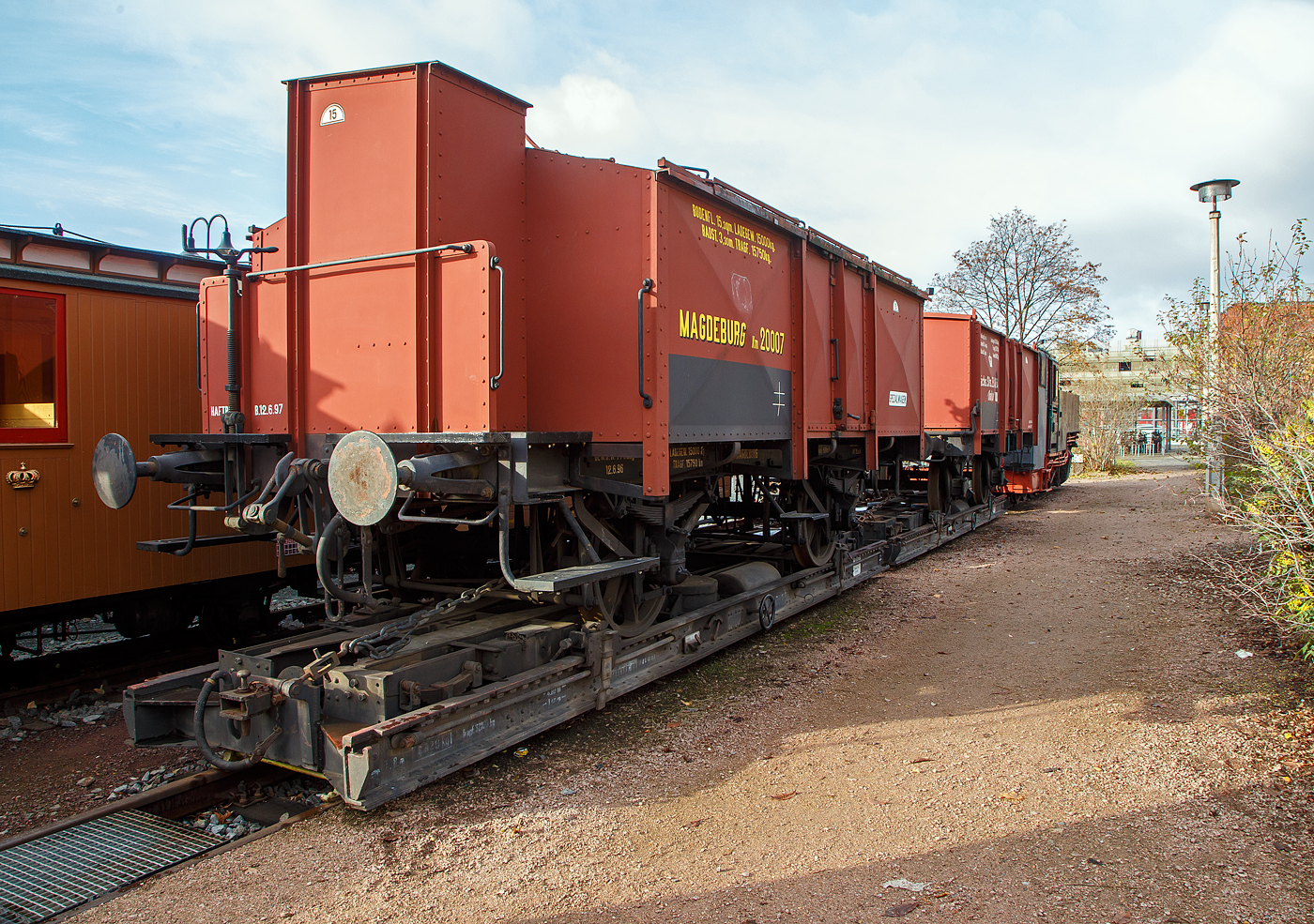 2-achsiger normalspuriger kurzer preußischer Klappdeckelwagen, eiserne Bauart mit Bremserhaus, der Königlich Preußischen Eisenbahn-Verwaltung (KPEV) Magdeburg Km 20007, (Güterwagen der Verbandsbauart), verladen auf dem 4-achsigen schmalspurigen 7,8 m Rollbockwagen ex DR 97-08-73, der Gattung Rf 4 (Sächs. Gattung 816), von der Traditionsbahn Radebeul e.V. derzeit (hier am 07.12.2022) aufgestellt am Museumsgleis 6 in Radebeul Ost. Der historische Regelspur-Güterwagen ist Eigentum vom Verkehrsmuseums Dresden.

Der Regelspur-Güterwagen der Verbandsbauart ist ein 2-achsige kurzer Klappdeckelwagen der eisernen Bauart  mit Bremserhaus, der Königlich Preußischen Eisenbahn-Verwaltung (KPEV) der Gattung Km. Die Wagen der Verbandsbauart  wurden zwischen 1910 - 1924 nach Plänen des Deutschen Staatsbahnwagen-Verbandes gebaut. Die Bezeichnung der Bauart beruht auf den Bestrebungen nach Vereinheitlichung im Güterwagenbau durch den Deutschen Staatsbahnwagenverband (DWV), dem alle acht damaligen Staatseisenbahnen (Länderbahnen) angehörten.

Diese Km Klappdeckelwagen mit 6 Klappdeckeln, Bremserhaus und Speichenrädern, waren für den Transport von nässeempfindlichen Schüttgütern (meist Kalk). Sie entsprachen weitgehend den Kalkwagen nach Musterblatt IId4. Das preußische Bremserhaus ist einseitig offen ausgeführt. Diese Wagen hatten eine Ladelänge von 5.295 mm, eine Ladebreite von 2.812 mm, ein Ladegewicht von 15 Tonnen und ein Ladevolumen von 18,6 m³. Diese geschlossenen Wagen waren so konstruiert das die Dachklappen und Seitentüren sehr dicht waren um das Transportgut gegen Sonne und Regen zu schützen, die sechs Dachklappen waren mittig an dem durchgehenden Dachfirst des Satteldachs befestigt, was das Beladen vereinfachte.

Die Wagen ohne Handbremse hatten eine Länge über Puffer von 6.600 mm und bis 1917 einen Achsstand von 3.000 mm. Die Wagen mit Handbremse (wie dieser) verfügten über ein geschlossenes Bremserhaus, eine Kunze-Knorr-Bremse, hatten eine Länge über Puffer von 7.300 mm, bis 1917 betrug ihr Achsstand 3.300 mm. Ab 1918 wurde der Achsstand für beide Wagenarten auf 3.500 mm festgelegt.

TECHNISCHE DATEN vom Wagen Magdeburg Km 20007:
Spurweite: 1.435 mm (Normalspur)
Anzahl der Achsen: 2
Länge über Puffer: 7.760 mm
Achsstand: 3.300 mm
Ladelänge: 5.295 mm
Ladebreite: 2.812 mm
Leergewicht: 8.720 kg
Ladegewicht: 15.000 kg (Tragfähigkeit 15.750 kg)
Ladefläche: 15,3 m²
Ladevolumen:18,6 m³.

Der Rollwagen:
Im Eisenbahnwesen ist der Rollwagen ein Nebenfahrzeug, mit dem Regelspurwagen auf Schmalspurbahnen befördert werden. 

Die Tatsache, die hauptsächlich verantwortlich für das Aufkommen von Rollwagen in Deutschland war, war das Fehlen eines zusammenhängenden Schmalspurnetzes. Daraus ergab sich, dass die Schmalspurstrecken in viele Inselbetriebe zerfielen, weswegen die Betriebsvorschriften nicht einheitlich waren. Während bei der Deutschen Reichsbahn pro Rollwagen nur ein zweiachsiger Normalspurwagen zugelassen war, verlud die Mittelbadische Eisenbahngesellschaft auch vierachsige Mineralölkesselwagen auf einzelne Rollwagen, die dementsprechend lang ausgestaltet waren. Bei der Reichsbahn verlud man Drehgestellwagen, sofern zulässig, auf zwei Rollwagen.
Rollwagen der Königlich Sächsischen Staatseisenbahnen.

Die Rollwagen der Königlich Sächsischen Staatseisenbahnen hatten alle eine Spurweite von 750 mm. Es gab sie in 8 unterschiedlichen Gattungen, Anzahl der Achsen und Längen, hier ist die sächsische Gattung 816 (Rf 4, ex Rf 6). Es ist ein vierachsiger Wagen mit einer Fahrbühnenhöhe von 400 mm und Fahrbühnenlänge von 7.800 mm.

TECHNISCHE DATEN vom Rollwagen:
Fahrzeugnummer: 97-08-73, Gattung Rf4
Spurweite: 750 mm 
Anzahl der Achsen: 4 (in 2 Drehgestellen)
Anzahl der Achsen: 4
Länge über Puffer: 7.800 mm (wie Fahrbühnenlänge)
Drehzapfenabstand: 4.800 mm
Achsabstand im Drehgestell: 1.400 mm
Eigengewicht: 6.920 kg
Tragfähigkeit: 32.000 kg
