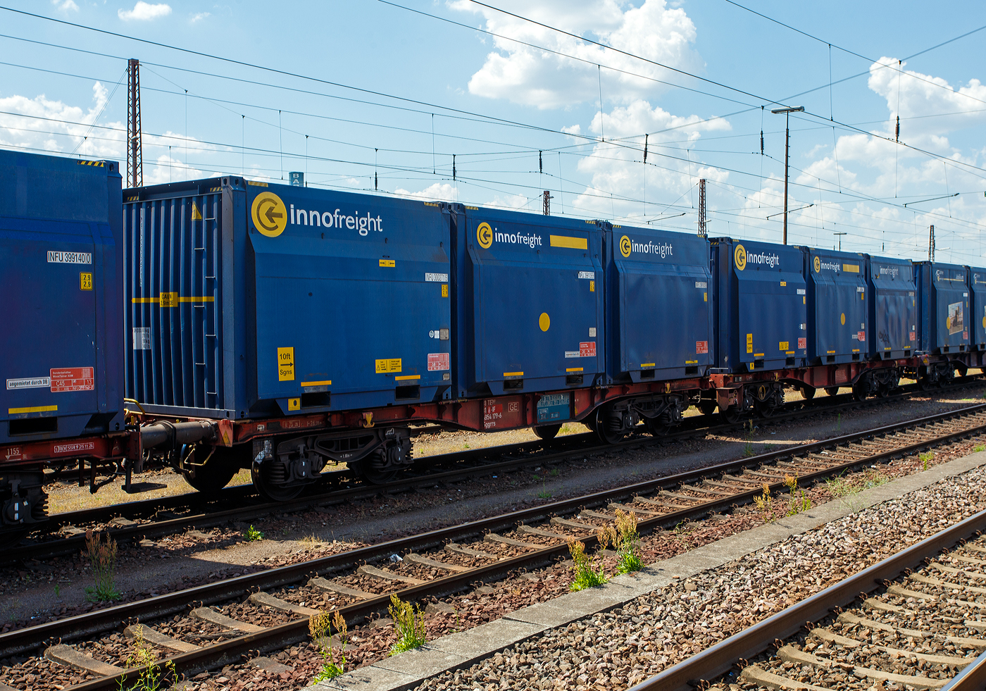 2 x 4-achsiger Flachwagen in Sonderbauart (Doppelwagen) bzw. ein 8-achsiger Containertragwagen, 31 81 4854 179-6 A-IF, der Gattung Sggrrs 80 ft, der �sterreichischen INNOFREIGHT hier als Wagon der Variante D02 - WoodTainer XXM mit sechs aufgesetzten WoodTainer XXM (2 x 3) mit einer L�nge von je 13' (KV Profil C45) vermietet an die DB Cargo AG, am 01 Juli 2025 abgestellt im Zugverband in Dillingen/Saar.

Grunds�tzlich besteht ein InnoWaggon aus zwei kurzgekuppelten Einzelwagen. Leichtbauweise und hohe Belastbarkeit differenzieren diese Waggons dabei klar von anderen und erm�glichen deutlich h�here Zuladung f�r den Transport von unterschiedlichsten G�tern. Der InnoWaggon vereint den Tragwagen und die auswechselbaren Beh�lter zu einem innovativen Konzept, das eine flexible Nutzung verspricht. Der Einsatz der Spezialbeh�lter wird dabei der jeweiligen Branche angepasst, da die Beh�lter je nach Anforderung wie spezifisches Sch�ttgewicht oder Entladestation eingesetzt werden.


TECHNISCHE DATEN des 2x40 ft InnoWaggon:
Gattung: Sggrrs
Gattungskennzahl: 4854
Hersteller: Tatravagonka Poprad (Slowakei), 
Spurweite: 1.435 mm (Normalspur)
Achsenanzahl: 8 pro Doppelwagen (in 4 Drehgestellen)
L�nge �ber Puffer: 26.710 mm 
Breite: 2.878 mm
Drehzapfenabstand: 2 x 8.070 mm
Achsabstand in den Drehgestellen: 1.800 mm
Raddurchmesser: 920 mm (neu)
L�nge Ladefl�che: 2 x 12.370 mm (2 x 40 ft)
H�he der Ladefl�che �ber SOK: 1.155 mm
Eigengewicht: 42.300 kg
Max. Geschwindigkeit: 100 km/h (beladen) / 120 km/h (leer)
Max. Zuladung pro Doppelwagen: 137,7 t (ab Streckenklasse D 3)
Bremse: KE-GP-A (K)
Bremssohle: C 810
Kleinster befahrbarer Gleisbogen: R 75m
Intern. Verwendungsf�higkeit: TEN-GE

TECHNISCH DATEN eines WoodTainer XXM:
L�nge: 13 ft / 3.962 mm
H�he: 2.900 mm
Breite: 2.900 mm
Eigenwicht: 2.150 kg
Max. Zuladung: 33.850 kg
Max. Gesamtgewicht: 36.000 kg
Ladevolumen: 29 m�
KV Profil: C45

Jeder Container besteht aus fixen Seitenw�nden und Stirnw�nden und ist nach oben hin offen. Im beladenen Zustand k�nnen bis zu drei Container gestapelt werden.

Die Positionierung der WoodTainer XXM auf dem Tragwagen erfolgt unter Verwendung von vier Container-Pins je Container.