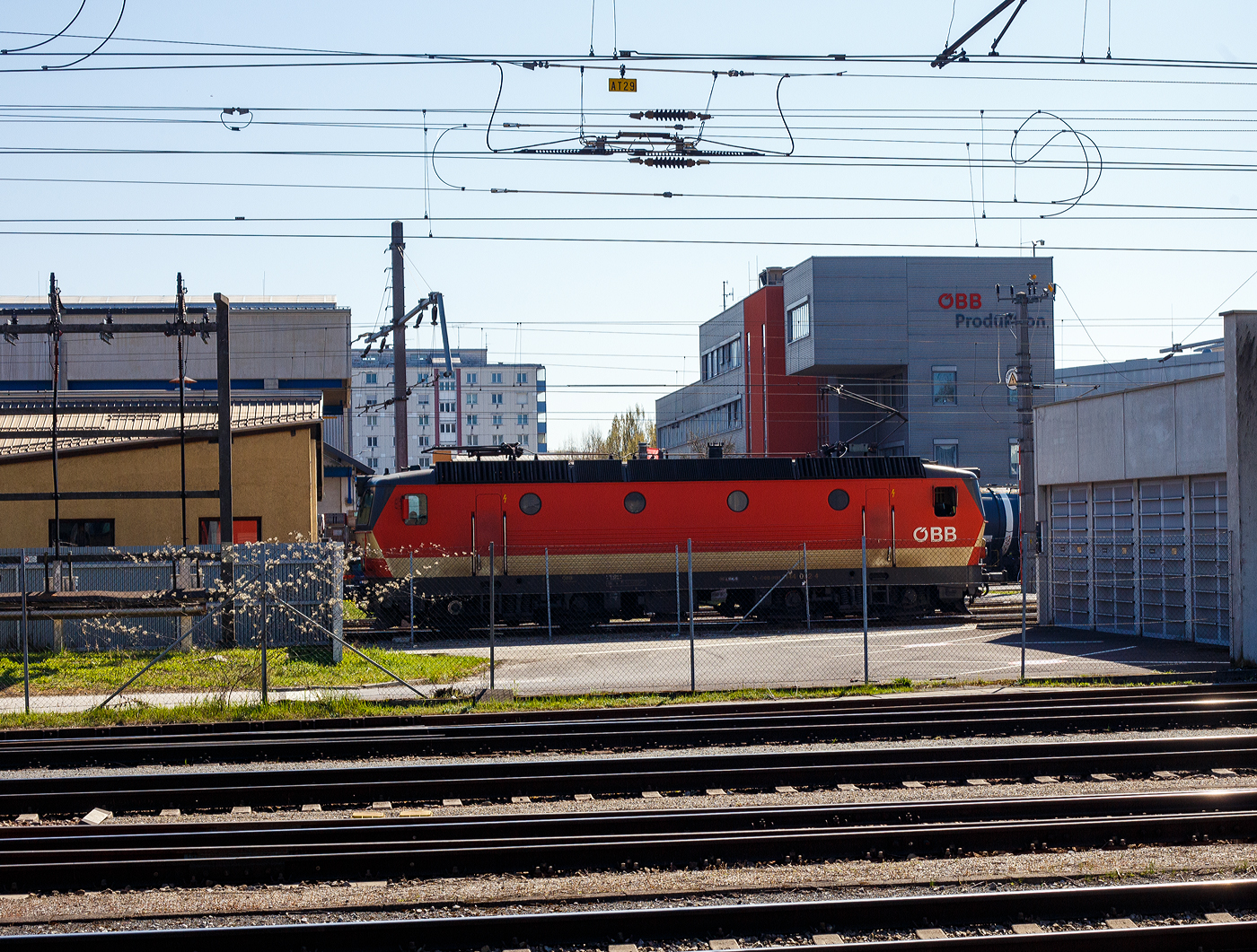 Alpenstaubsauger“ seit 50 Jahren im Dienst
Der „Alpenstaubsauger“ ÖBB 1144 092-4 (A-ÖBB 91 81 1144 092-4) der ÖBB-Produktion GmbH, ex ÖBB 1044 092-3, ex ÖBB 1044.92, rangiert am 04 April 2025, gegenüber dem Hauptbahnhof, im Bahnbetriebswerk Linz/Werk Linz der ÖBB Technische Services GmbH (ehemals ÖBB-Hauptwerkstatt Linz).

Die ÖBB-Produktion GmbH ist heute für die Traktion und Fahrzeugservice der Österreichischen Bundesbahnen im ÖBB-Konzern zuständig. Für die Wartung, Instandhaltung und Modernisierung ist wiederum die ÖBB Technische Services GmbH / ÖBB Train Tech zuständig.

Seit 50 Jahren sind die Lokomotiven der Reihe 1044/1144 unterwegs. Über Jahrzehnte prägten sie das Bild der Bahn. Ihr Lüftergeräusch brachte der Lok mit den Bullaugen den Spitznamen „Alpenstaubsauger“ ein. Sie noch regelmäßig unterwegs, allerdings werden sie immer mehr von moderneren Loks verdrängt.

Im Güterverkehr ist die Lok, die nun als 1144 bezeichnet unterwegs, u.a. in Tirol noch täglich zu sehen, vor allem auf der Strecke von Kufstein bis zum Arlberg. Auch vor Wendezügen versieht sie noch Dienst, diese nicht klimatisierten Züge werden aber zunehmend von Triebwagengarnituren abgelöst. Auch wenn die ehemals stärkste vierachsige Lokomotive der Welt etwa 1.000 Kilowatt weniger Leistung als etwa die modernen Taurus- oder Vectron-Loks hat, heißt das nicht, dass sie sich völlig geschlagen geben muss.

Lok kann ihre Leistung gut auf die Schiene bringen:
Bei einer Lokomotive geht es vor allem darum, ihre Leistung auch auf die Schiene zu bringen und gerade bei widrigen Wetterverhältnissen kann die alte Lok ihre Vorzüge ausspielen, wenn sie etwa am nassen Gleis ein kontrolliertes Durchrutschen der Räder zulässt, das deutlich hörbar ist und auch unter der Bezeichnung „Makroschlupf“ bekannt ist. Das ist aber nur ein Aspekt der technischen Meisterleistung, die hinter dieser Lok steckt.

Entwickelt wurde die Lok von österreichischen Firmen, es wurde aber auch teilweise die Technik einer schwedischen Lok (der Rc2) übernommen, die in Österreich als Reihe 1043 im Dienst stand und bereits eine stufenlose Steuerung der Zugkraft aufwies. Die Versuche mit dieser Lok waren sehr positiv ausgefallen. Diese sogenannte „Thyristorsteuerung“ wurde auch bei der 1044 übernommen, allerdings war die 1044 für höhere Geschwindigkeiten und deutlich mehr Leistung ausgelegt. Damit konnte mit dieser Lok leistungsmäßig die Grenze einer Stufensteuerung überwunden werden.

Die Thyristoren werden mit Öl gekühlt, „diese möchten sehr gut gekühlt werden, weil da einfach viel Leistung erzeugt wird“. Aufgrund dieser Luftdurchsatzmenge ist dann das Heulen entstanden, das der Lok ihren Spitznamen „Alpenstaubsauger“ einbrachte.

Ab 1978 in Serie gefertigt:
Zuerst rief man die Baureihe 1044 mit zwei Prototypen ins Leben. Der erste Prototyp, die 1044.01, war ab 1974 im Einsatz. Ab 1978 wurden die Serienloks in Dienst gestellt. Die 1044 war eine klassische Universallokomotive, die für alle Züge eingesetzt werden konnte. Von Kinderkrankheiten blieb auch diese Reihe nicht verschont, Radreifenbrüche und vor allem Ausfälle durch Flugschnee machten Änderungen bei der Konstruktion notwendig.

Aus der 1044 wurde die 1144:
Letztlich bewährten sich die Lokomotiven aber sehr gut und sie wurden für Jahrzehnte zum Paradepferd der ÖBB. Die Lokomotiven mit einer Leistung von bis zu 5.400 Kilowatt waren für 160 km/h zugelassen. Mit dem Umbau zur Tauglichkeit für Wendezugbetrieb mit Steuerwagen wurde aus der 1044 die 1144. Zuletzt im Jahr 1995 wurden nochmals 36 Stück der Lokomotive bestellt, ehe im Jahr 2000 mit der „Taurus“ ein Nachfolger den Dienst antrat.

Ein einheitliches Erscheinungsbild haben die Loks bis heute nicht. Sie sind in verschiedenen Lackierungen unterwegs und ein Blick auf die Lüftungsgitter auf der Dachkante verrät eine große Vielfalt, hier gibt es niedrige Gitter, hohe Gitter, gemischte Varianten, Gitter mit Schalldämpfern sowie Gitter ohne Schalldämpfung. Die erste Prototyplokomotive (1044.01) wurde zu einer Schnellfahrlokomotive umgebaut, die für 220 km/h zugelassen ist und die Bezeichnung 1044.501 erhielt. Insgesamt wurden 217 Stück der 84 Tonnen schweren und 16,1 Meter langen Lok gebaut.

Die Bremsenergie wird in Wärme statt Strom umgewandelt
Seit dem Jahr 2018 werden immer wieder Maschinen der Reihe 1144 ausgemustert. Ein Nachteil gegenüber modernen Maschinen ist, dass sie die beim elektrischen Bremsen gewonnene Energie in Wärme umwandelt und nicht als Strom ins Netz rückspeisen kann.

Mittlerweile veraltete Steuerungstechnik
Die Thyristortechnik ist inzwischen „veraltet“. So erzeugt diese Technik auch eine gewisse „Blindleistung“, welche das Stromnetz geschwächt. Das ist kein großes Problem, hat es aber etwas herausfordernder gemacht. Eine Prognose, wie lange die 1144 noch im regulären Einsatz steht ist noch unklar. Das entscheide der Fahrzeugeigentümer. Aber mit der Möglichkeit, Strom in die Fahrleitung zurückzuspeisen, erspart man sich schon sehr viel Geld. Somit haben modernerer Loks eine höhere Wirtschaftlichkeit.
