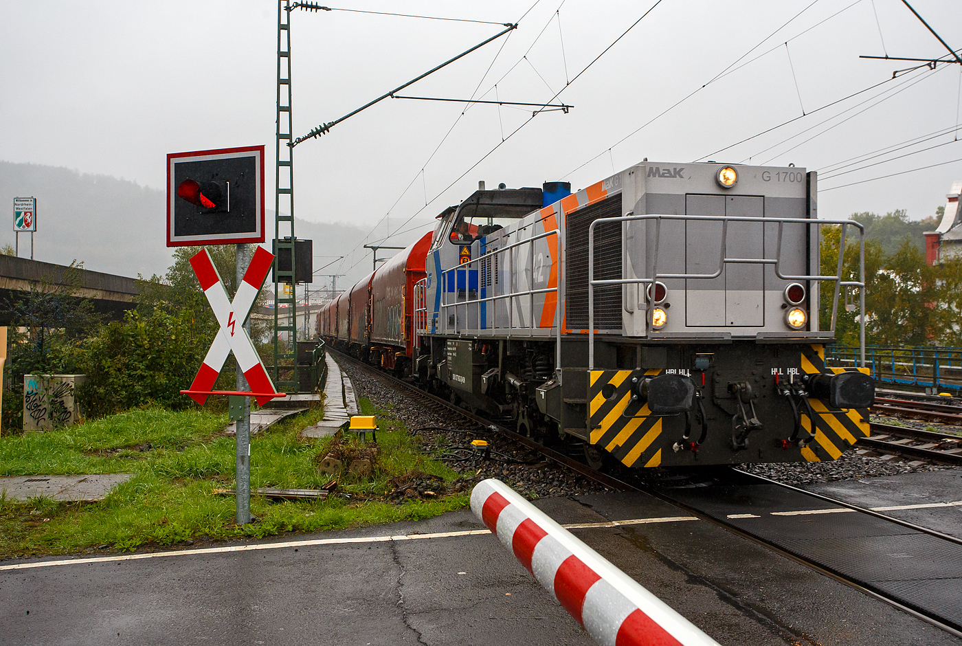 Auch bei Regen fahren Züge, so ging ich auch nochmal an die Strecke. Die KSW 42 bzw. 277 902-3 (92 80 1277 902-3 D-KSW) der KSW (Kreisbahn Siegen-Wittgenstein), fährt am 06 Oktober 2025, mit einem Coilzug durch Niederschelden/Niederschelderhütte in Richtung Betzdorf/Sieg. Man kann es an dem Schild an der B62 oben links erkennen, der Zug überquert die Sieg und passiert somit die Landesgrenze zwischen NRW und Rheinland Pfalz.

In Betzdorf setzt die Lok dann um und bringt dann den Coilzug, über die KBS 462 „Hellertalbahn“, nach Herdorf auf den KSW Rangierbahnhof Herdorf (Freien Grunder Eisenbahn KSW NE447 / DB-Nr. 9275). 