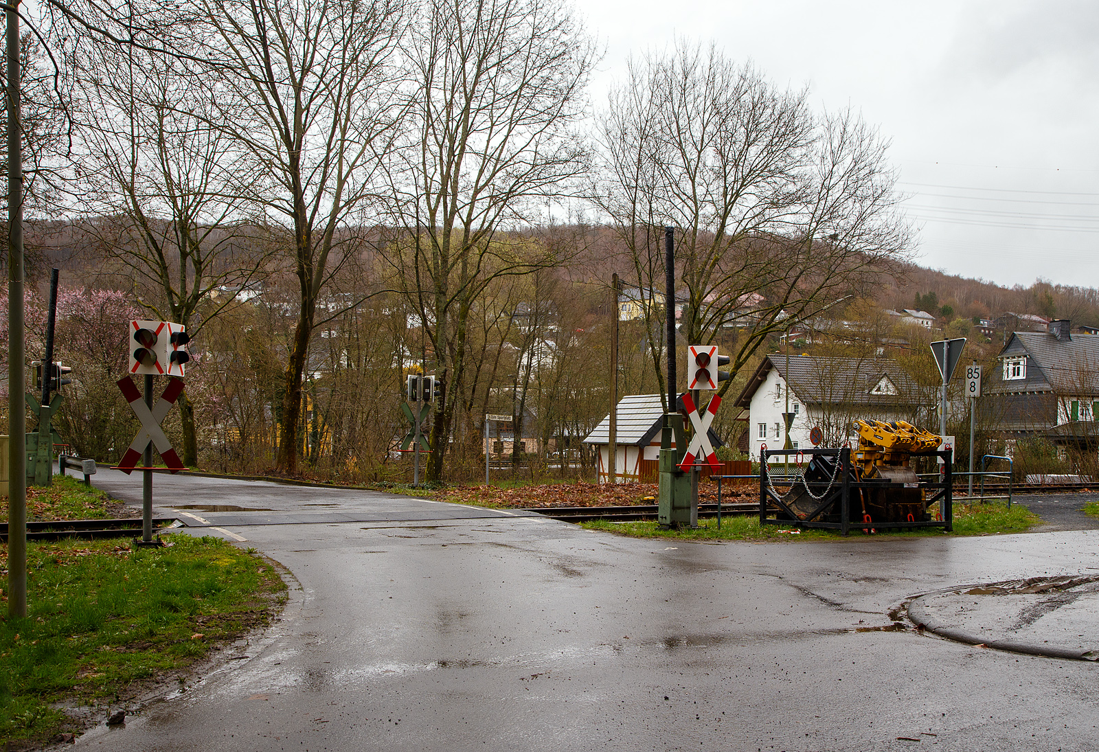 Bahnübergang (BÜ) bei km 85,8 an der Hellertalbahn KBS 462 beim Hp Grünebach Ort am 01.04.2023. Da der Streckenabschnitt zwischen Betzdorf (Sieg) und Herdorf Hp. Königstollen, ist wegen dem Felsstutz am 23.12.2022, seitdem bis voraussichtlich zum kleinen Fahrplanwechsel am 09. Juni 2023 gesperrt. So sind hier die Schranke mit schwarzer Folie umwickelt und die Lichtzeichen verdeckt und durchgeixt. 

Dies heißt aber nicht dass Schienenfahrzeuge keinen Vorrang haben und man als Verkehrsteilnehmer nicht auf Schienenverkehr achten muss, denn die Andreaskreuze sind nicht abgehangen und behalten die Gültigkeit. Vielmehr ist der Grund hier das bei kreuzenden ettl. Schienenverkehr sich die Schranken nicht schließen und kein Rotlicht gezeigt wird. Die Sicherungseinrichtungen können demontiert sein und für z.B. die Hangsicherungsarbeiten beim Hp. Königstollen kann Zugverkehr stattfinden.
