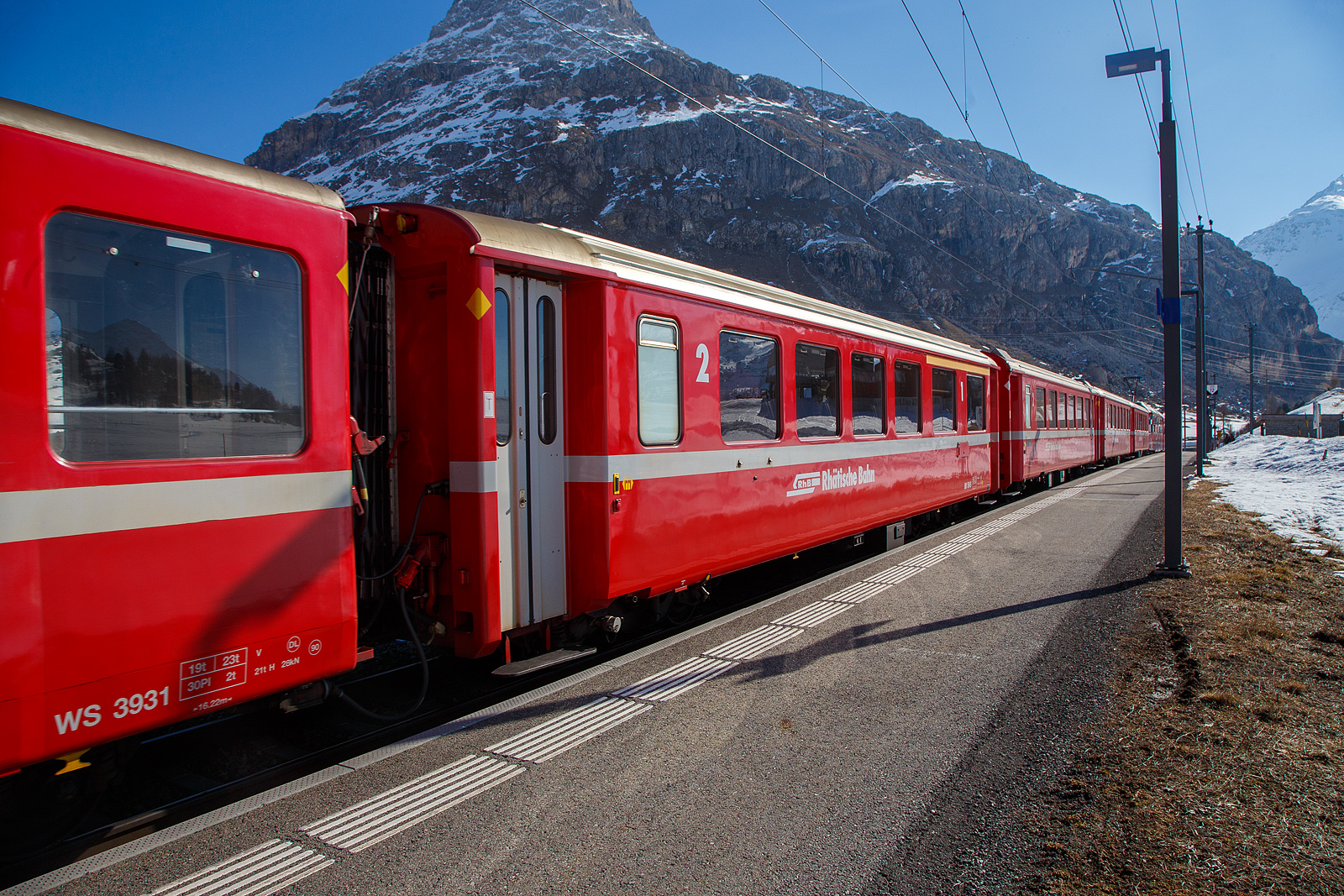Berninabahn Personenwagen RhB AB 1545 (Baujahr 1968) ein verk�rzter 1./2.Klasse Einheitswagen I (EW I) mit Aluminiumwagenkasten am 22.03.2023 in der Station Bernina Diavolezza (2.082 m �. M.) im Zugverbund.

Mit mehr als 100 Fahrzeugen bilden die als Einheitswagen I bezeichneten Personenwagen bis heute die gr��te Serie im Rollmaterialbestand der RhB. Das Fahrzeugkonzept wurde Anfang der sechziger Jahre in enger Zusammenarbeit zwischen Industrie und RhB entwickelt. Als Neuheit galten damals die Einstiegsbereiche mit WC und Stauraum f�r sperriges Gep�ck an den Wagen�berg�ngen. Folglich weicht das Konzept deutlich von den Mitteleinstiegswagen aus den vierziger Jahren ab.

Die ersten von FFA und SIG gebauten Einheitswagen I wurden Ende 1963 in Betrieb genommen. In einem Zeitraum von etwa zehn Jahren wuchs der Bestand an EW I kontinuierlich. Neben den 18,42 m langen Wagen, die haupts�chlich auf dem Stammnetz eingesetzt werden, kamen auch Sonderbauformen mit Aluminiumwagenkasten hinzu. Zu diesen z�hlen beispielsweise diese auf 14,91 m verk�rzten Fahrzeuge f�r den Einsatz auf der Berninabahn. Um auch die dort engen 50 m Radien befahren zu k�nnen, wurden die Wagen AB 1541-1546 bzw. B 2307-2314 sowie B 2451-2460 deutlich l�ngenverk�rzt ausgef�hrt. Die Fahrzeuge werden heute noch in vielen Regionalz�gen auf der Berninalinie eingesetzt, sie laufen aber auch auf dem Stammnetz und haben zudem eine Zulassung f�r die benachbarten MGB (ex FO/BVZ). 

TECHNISCHE DATEN:
Baujahr und Hersteller: 1968 / Flug- und Fahrzeugwerke Altenrhein AG (FFA)
Spurweite: 1.000 mm
Anzahl der Achsen: 4
L�nge �ber Puffer: 14.910 mm
Drehgestellart: SWP 68
Sitzpl�tze: 12 (1.Klasse) / 30 (2.Klasse)
Eigengewicht: 14,0 t
Max. Gesamtgewicht: 17 t
zul�ssige Geschwindigkeit: 90 km/h
Lauff�hig: StN (Stammnetz) / BB (Berniabahn) / MGB (Matterhorn Gotthard Bahn)
