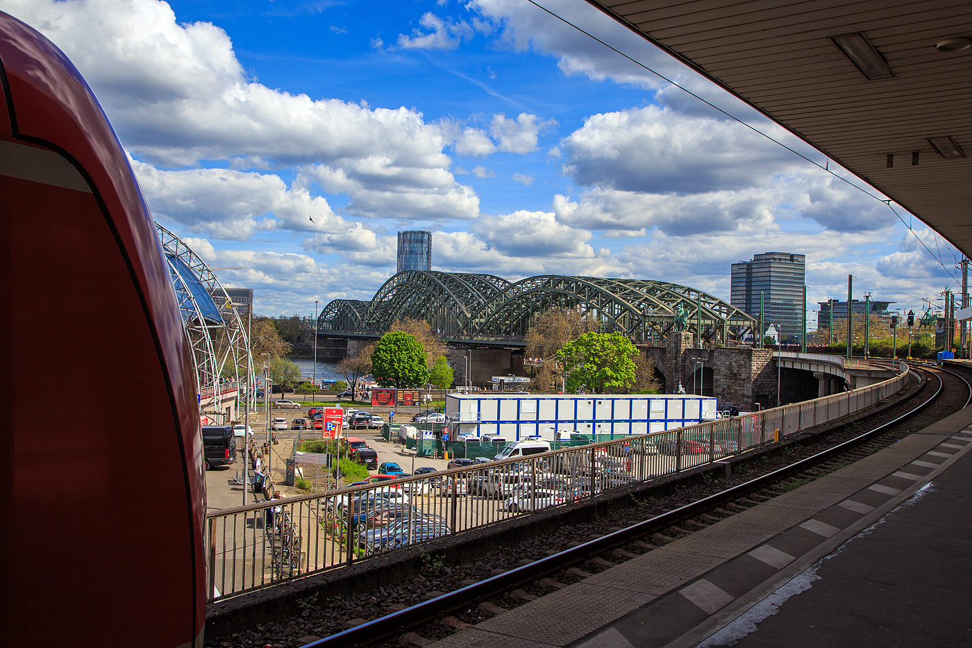 Blick auf die Hohenzollernbrücke in Köln vom Bahnsteig 11 des Hauptbahnhofes am 30.04.2023.

Die Hohenzollernbrücke wurde von 1907 bis 1911 gebaut. Sie ersetzte die Dombrücke, die den Anforderungen des stetig zunehmenden Eisenbahnverkehrs nicht länger gewachsen war. Das Besondere am Bau der neuen Brücke war, dass sie unter laufendem Betrieb der Dombrücke errichtet wurde und diese nach und nach ersetzte. Sie bestand nach ihrer Fertigstellung aus drei nebeneinander liegenden Fachwerkbogenbrücken mit jeweils drei Bögen.

Die Hohenzollernbrücke ist die einzige Brücke in Köln, die nicht durch Bomben zerstört wurde. Vielmehr übernahm es die Wehrmacht am 6. März 1945 selbst, den herannahenden Alliierten durch Sprengung der Brücke eine Rheinüberquerung zu erschweren. Nach dem Krieg wurde bis 1948 zunächst eine der (zweigleisigen) Bahnbrücken wieder aufgebaut. Die Straßenbrücke wurde aus verkehrstechnischen Gründen nicht wiederhergestellt. In den Jahren 1956 bis 1959 und von 1986 bis 1987 wurde jeweils ein weiterer Fachwerkbogen hinzugefügt, so dass die Bahn heute über sechs Gleise auf der Hohenzollernbrücke verfügt. Die zwei nördlichen Gleise sind der S-Bahn vorbehalten. Bei der Hohenzollernbrücke gibt es zu beiden Seiten Geh- und Radwege, die von der Stadt Köln unterhalten und gepflegt werden, während sich die Brücke selbst, wie auch die Südbrücke, im Eigentum der Deutschen Bahn AG befindet.

Mit etwa 1220 Zugfahrten pro Tag ist sie eine der meistbefahrenen Eisenbahnbrücken in Deutschland.  Das Bauwerk gilt, zusammen mit dem Kölner Hauptbahnhof, als zentraler Engpass im Schienenverkehr in der Region Köln.

Technische Daten:
Typ: sechsgleisige Eisenbahnbrücke mit Geh- und Radwegen auf beiden Seiten
Bauart: drei nebeneinander liegende Fachwerkbögenbrücken
Baujahre: je eine Brücke 1946 bis 1948, 1956 bis 1959 und 1986 bis 1987
Spannweiten: 111,88 Meter - 167,75 Meter - 122,56 Meter, insgesamt 409,19 Meter
Gesamtbreite: 26,20 Meter
