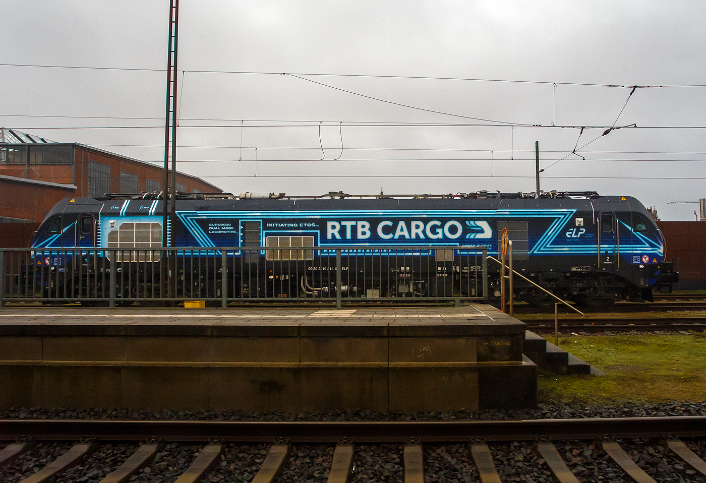Blick aus dem Zug heraus...
Die an die RTB CARGO GmbH (Düren) vermietete Stadler EURO 9000 der ELP - European Loc Pool AG (Frauenfeld/CH) 2019 311-0 (90 80 2019 311-0 D-ELP) steht am 14 Februar 2024 beim Bahnhof Lingen (Ems)

Die Stadler EURO 9000 eine Co'Co'- DualModeLok wurde 2023 von Stadler Rail Valencia S.A.U. in Albuixech (Spanien) unter der Fabriknummer  4073  gebaut und an die ELP - European Loc Pool AG in Frauenfeld (CH) ausgeliefert. Seit 26.01.2024 ist sie an die RTB CARGO GmbH (Düren) vermietet. 

Seit Mai 2019 hat der European Loc Pool (ELP) dreißig elektrische Co’Co’-Lokomotiven des Typs EURO 9000 bei Stadler bestellt, um sie an Bahnbetreiber aus verschiedenen Ländern zu vermieten. Dieser Auftrag ist Teil des Rahmenvertrags zwischen Stadler und ELP über insgesamt 100 Lokomotiven. Seit 2023 sind die ersten Loks dieses Typs zugelassen und ausgeliefert. Die Euro9000 Plattform ist die konsequente Weiterentwicklung der bekannten Stadler Lokomotiv-Familie EuroDual und Euro4000.

Die leistungsstarken Mehrsystem-Zweikraftlokomotiven mit dieselelektrischem und elektrischem Antrieb für den Streckendienst, ermöglichen den Betrieb auf elektrifizierten Gleich- und Wechselstrom-Strecken. Sie sind aber auch mit zwei Dieselmotoren für den Betrieb auf nicht elektrifizierten Strecken ausgestattet. Die TSI-konformen Lokomotiven sind für den Betrieb auf den wichtigsten europäischen Eisenbahnkorridoren einschließlich der folgenden Länder vorgesehen: Deutschland, Österreich, Schweiz, Italien, Belgien und Niederlande. Alle haben die entsprechenden Länderpakete, ETCS und Funkfernsteuerung als Standardausrüstung. 

Die Hochleistungslokomotiven (duale Multisystem-Lokomotiven) verfügen über zwei komfortable Fahrerkabinen, eine leichte Ganzschalenstruktur, ein Wechselstrom-Antriebssystem und einen hohen Grad an Redundanz der Hauptantriebskomponenten. Die EURO9000 ist auf dem neuesten Stand der Technik. Mit einem Leistungsbereich von bis zu 9 MW und einer hervorragenden Zugkraft von bis zu 500 kN wird die EURO9000 in vielen Fällen den Betrieb mit nur einer Lokomotive ermöglichen, wo heute zwei Lokomotiven erforderlich sind. Die neueste Drehgestell-Technologie führt zudem zu einer geringeren Abnutzung der Infrastruktur und zu geringeren
Netznutzungsgebühren.

Die Euro9000, die Lokomotive der „nächsten Generation“, steht für Spitzenleistung in der europäischen Schienengüterverkehrsbranche. Mit einer Zugkraft von 500 kN und einer Leistungsfähigkeit von bis zu 1,9 MW im Dieselbetrieb und 9 MW im Elektrobetrieb ermöglicht sie eine bis zu 50% höhere Beladungskapazität. Eine ihrer bemerkenswertesten Eigenschaften ist die ‘Boost’-Fähigkeit auf 3-kV-DC-Strecken (Gleichstom), die es der Euro9000 ermöglicht, ihre elektrische Leistung durch die Hinzunahme der Dieselkraft zu steigern und so eine beeindruckende kombinierte Leistung von 7,7 MW auf den Rädern zu erreichen.

TECHNISCHE DATEN:
Spurweite: 1.435 mm (Normalspur)
Achsanordnung: Co’Co’ 
Länge über Puffer: 23.020 mm
Drehzapfenabstand: 14.000 mm
Breite: 2.900 mm
Höhe: 4.290 mm
Achsabstand im Drehgestell: 3.600 mm (2 x 1.800 mm)
Treibdurchmesser: 1.067 mm (neu)
Eigengewicht: 120 t
Achslast: 20 t
Höchstgeschwindigkeit: 120 km/h
Elektrische Leistung am Rad: bis zu 9.000 kW
Leistung bei Dieselantrieb: 1.900 kW (2.582 PS)
Anfahrzugkraft: 500 kN
Dauerzugkraft: 430 kN

Dieselmotor (2 Stück verbaut, Daten eines Motors):
Motorbauart: Caterpillar  V-12-Viertakt-Dieselmotor mit Abgasturbolader und Ladeluftkühlung (TA), sowie  Direkteinspritzung vom Typ CAT C32 
Motorleistung: 950 kW (1.291 PS)
Motornenndrehzahl: 1.800 U/min
Hubraum: 32,1 l (Bohrung Ø 145 mm / Hub 162 mm)
Verdichtungsverhältnis: 16,5:1
Motorgewicht (trocken): ca. 13.000 kg
Motorabmessung: 1.917 x 1.479 x 1.319 mm (l x b x h)
Abgasnorm: Stufe V

Anzahl der Fahrmotoren: 6
Antrieb: elektrisch (AC/AC) oder dieselelektrisch
Speisespannung: 25 kV 50 Hz und 15 kV 16.7 Hz
Tankinhalt Diesel: 1.800 l
Bremssystem Mechanisch: Pneumatisch 
Bremssystem Dynamisch: Regenerativ/Rheostatisch
Primär Federung: Schraubenfedern
Sekundär Federung: Gummi-Metall Vertikal- und Horizontaldämpfer
Zugbeeinflussung: PZB, ETCS

Quellen: ELP, Stadler Rail und CAT
