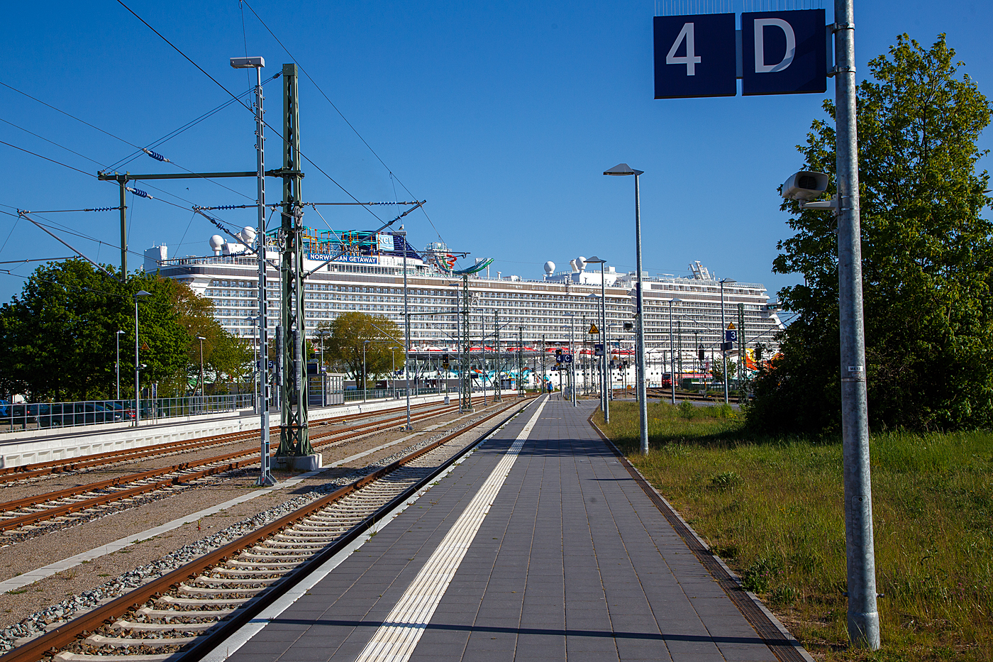 Da braucht es schon einige Züge, wenn man die ganzen Passagiere in Züge packen will. Der Bahnhof Warnemünde am 15 Mai 2022, hinten im Warnemünde Cruise Center liegt am Warnemünde Passagierkai, Pier 8, das gewaltige Kreuzfahrtschiff NORWEGIAN GETAWAY der US-amerikanischen Reederei Norwegian Cruise Line Corporation Ltd. (NCL). Da sieht der dreiteilige Bombardier Talent 2 (BR 442/443) der S-Bahn Rostock, der gerade kommt, wie ein größeres Rettungsboot des Schiffes aus.

Wenn man bedenkt dass das Warnemünde Cruise Center für einen Passagierwechsel von bis zu 2.500 Personen am Tag ausgelegt ist, würde es bei diesem Schiff  mit bis zu 4.000 Passagier alleine 1 1/2 Tage brauchen um die kompletten Passagier zu wechseln. Schlimmer wäre aber solch ein Schiff kommt mal in Seenot, wie lange bracht es da um die fast 6.000 Menschen (Passagiere und Besatzungen) sicher von Bord zu bekommen. Da machen wir doch lieber Schienen-Kreuzfahrten. 

TECHNISCHE DATEN der Norwegian Getaway:
Flagge: Bahamas
Bauwerft: Meyer Werft GmbH Papenburg, Deutschland (Baunummer S.692) 
Baureihe: Breakaway-Klasse
Kiellegung / Stapellauf / Übernahme: 30.10,2012 / 02.11. 2013 / 10.01.2014	
Vermessung: 145.655 BRZ
Länge: 324 m
Breite auf Spanten: 39,7 m (über alles 52 m)
Anzahl der Decks: 18
Anzahl der Passagierkabinen: 2.015
Passagiere: 3.963
Besatzung: ca. 1646
Energieversorgung:4 MAN-Dieselgeneratoren
Propeller:	2 × Azipod
Maschinenleistung gesamt: 67.200 kW (84.840 PS)
Antriebsleistung (Dieselelektrischer Antrieb): 42. 000 kW (42 MW)
Max. Geschwindigkeit:  21,5 kn (40 km/h)
Anzahl der Restaurants: 21
Anzahl der Pools: 3

Der Bahnhof Warnemünde liegt im gleichnamigen Ostseebad, einem Ortsteil der Hansestadt Rostock. Das Empfangsgebäude und einige weitere Anlagen des Bahnhofs stehen unter Denkmalschutz. Der Bahnhof ist Endpunkt der Linien S1, S2 und S3 der S-Bahn Rostock. Neben dem Rostocker Hauptbahnhof ist er der zweite Fernverkehrsbahnhof Rostocks mit Verbindungen nach Dresden, Leipzig oder Wien. Bis 1995 war er Ausgangspunkt der Fähren nach Gedser in Dänemark. Es sind es nur noch wenige Meter zu Fuß bis zum 2005 eröffneten Warnemünder Cruise Center, ca. 5 Minuten auch mit Gepäck.

Quellen: Meyer Werft, NCL, Rostock PORT/ Rostock.de, Wikipedia
