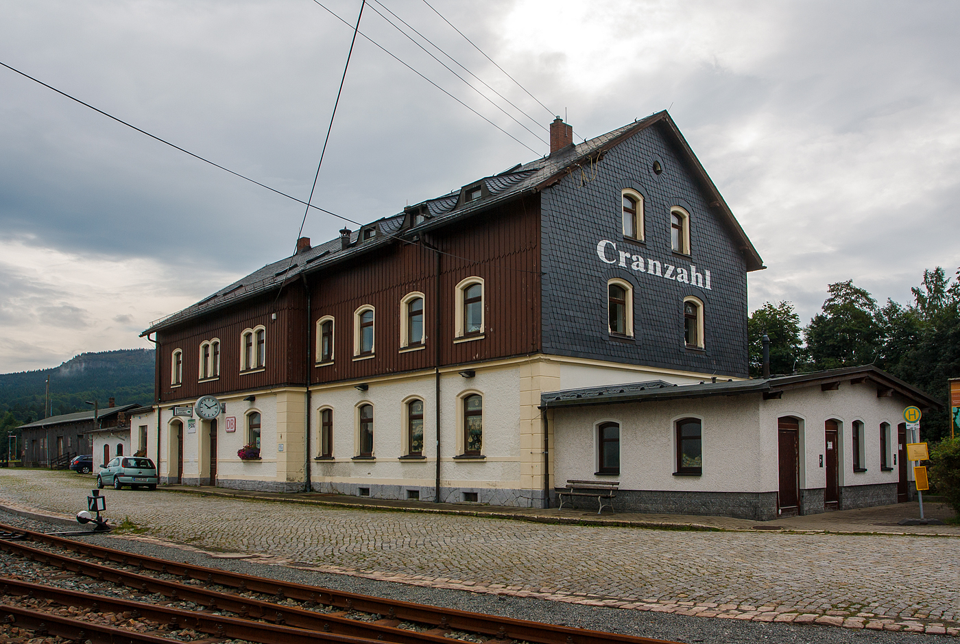 Das Empfangsgeb�ude des Bahnhof Cranzahl am 26 August 2013.

Der Bahnhof Cranzahl ist eine Betriebsstelle der Bahnstrecke Vejprty (Weipert) - Annaberg-Buchholz unt Bf (KBS 517) und der hier anschlie�enden Schmalspurbahn Cranzahl–Kurort Oberwiesenthal (SDG Fichtelbergbahn / KBS 518) auf dem Gebiet des Ortsteiles Cranzahl der Gemeinde Sehmatal im s�chsischen Erzgebirgskreis.

Cranzahl erhielt an der am 3. August 1872 er�ffneten Bahnstrecke Weipert–Annaberg einen Bahnanschluss. 1880 wurde der erste Teil des heutigen Empfangsgeb�udes errichtet. Mit dem Bau der Schmalspurbahn (am 19. Juli 1897 er�ffnet) wurde auch der Bahnhof erweitert. Das Empfangsgeb�ude wurde ebenfalls umgebaut und erhielt seine heutige Form. An Hochbauten wurde ein einst�ndiges Heizhaus, eine Umladehalle und eine Betriebsmittel�berladerampe neu errichtet.

Bereits bei der Projektierung war eine Rollbockgrube eingeplant, die 1899 gebaut wurde. 1906 wurde diese durch eine Rollwagengrube ersetzt. Durch den unerwartet hohen Wintersportausflugsverkehr stellte der Bahnhof ein Betriebshindernis dar. Bereits um 1900 wurde f�r die Schmalspurbahn ein zweites Bahnsteiggleis gebaut, aber auch dieses konnte das Problem nicht l�sen. Ab 1912 wurde daraufhin der Bahnhof grundlegend erweitert. Es wurde s�dlich der Normalspuranlagen ein neuer Bahnhofsteil f�r den Personenverkehr der Schmalspurbahn gebaut. Dazu musste ausreichend Bauplatz in den Berghang gesprengt werden. Seit dem Abschluss der Umbauarbeiten m�ssen Personenz�ge nicht mehr die Normalspurstrecke �berqueren, auch sind Schmalspurzugkreuzungen in Cranzahl m�glich. Die G�teranlagen verblieben an der bisherigen Stelle. Seitdem haben sich die Anlagen des Bahnhofs kaum ver�ndert. Das haupts�chlich als Werkstatt genutzte Heizhaus erhielt in den 1920er Jahren einen Anbau mit einer Werkstatt.

Cranzahl bekam in den Sommermonaten des Jahres 1969 ein Eilzugpaar von Berlin, das �ber Zwickau fuhr, der in Annaberg-Buchholz S�d „Kopf machte“. Cranzahl erhielt im Jahre 1971 ein t�gliches Eilzugpaar von Leipzig kommend und wieder zur�ck, dieses verkehrte noch bis zum 1. Juli 1991. Der Eilzug hielt aber nie in Annaberg-Buchholz. Im Jahre 1991 war das Ende der Eilz�ge nach Cranzahl eingeleitet.

Obwohl alle Lokomotiven der Schmalspurbahn immer in Oberwiesenthal stationiert sind, wurden die Dampflokomotiven lange Zeit in Cranzahl bekohlt. Der daf�r vorhandene Kran wurde in den 1980er Jahren durch ein F�rderband ersetzt. Seit Herbst 2023 erfolgt die Bekohlung am Bahnhof Oberwiesenthal. Grund daf�r ist die Anlieferung der Kohle auf der Stra�e, welche bislang bis Cranzahl per Schiene erfolgte.

Die Weichen und Signale des Bahnhofs Cranzahl werden �ber ein mechanisches Stellwerk der Bauart J�del 11000 gestellt. Die Ausfahrsignale sind als Formsignale, die Einfahrsignale als Lichtsignale nach dem Hl-Signalsystem ausgef�hrt, die �ber Hebel gestellt werden. 

Bis 2034 soll der Bahnhof Cranzahl elektrifiziert werden. Der Grund hierf�r ist der Einsatz von Akkutriebz�gen, welche die starke Steigung von Annaberg-Buchholz S�d nach Cranzahl nicht schaffen w�rden.
