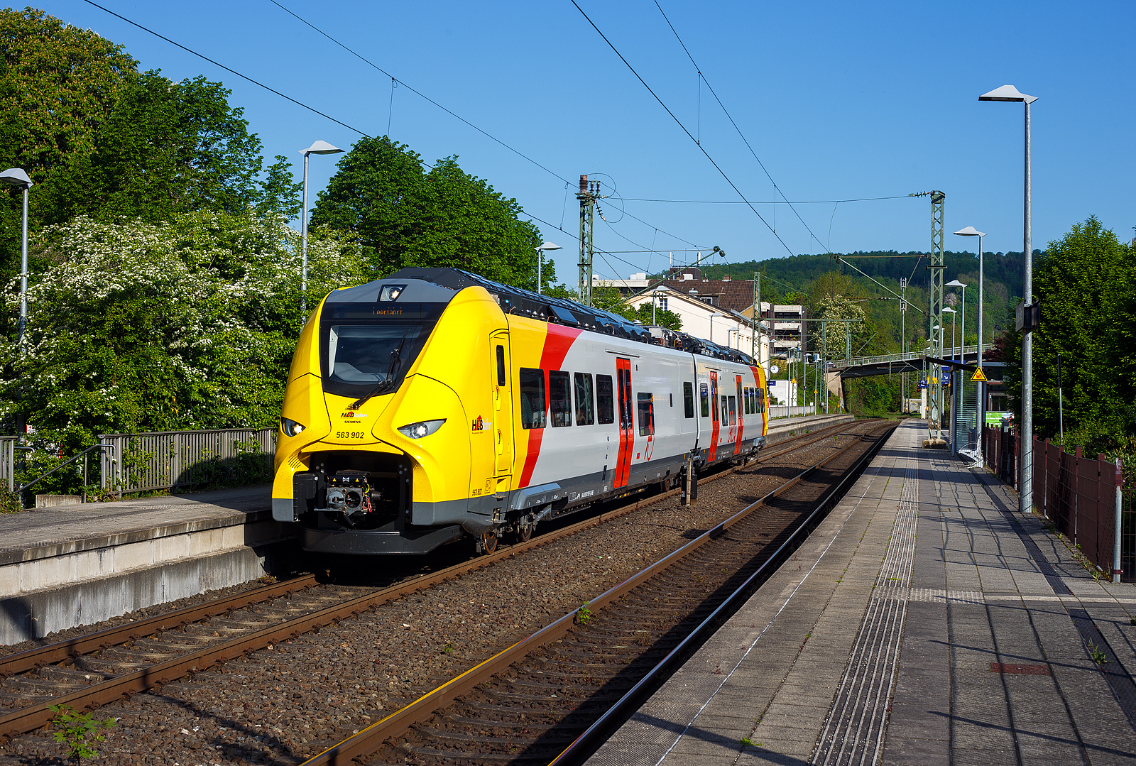 Das ist der neue Klimaschutz am Westerwald....
Einer der drei neuen zweiteiligen Hybridtriebz�ge (E/Akku) der BR 563 vom Typ SIEMENS Mireo Plus B der HLB (Hessische Landesbahn GmbH). Der HLB 563 802 / 563 902 (94 80 0563 802-8 D-HEB / 94 80 0563 902-6 D-HEB) f�hrt am 02 Mai 2025 auf Leerfahrt durch den Bahnhof Kirchen/Sieg in Richtung Betzdorf, hier hat er kurz Hp 0. Der Triebzug f�hrt hier sogar im Batteriemodus, denn es kein Stromabnehmer angehoben.  

Der zweiteilige SIEMENS Mireo Plus B wurden 2024/25 von SIEMENS in Krefeld gebaut und im April 2025 an die HLB ausgeliefert.

Auszug aus der Pressemitteilung der HLB:
Alternative Antriebe im Norden von Rheinland-Pfalz: Durchbruch beim Pilotprojekt mit Batteriez�gen im Westerwald / Zuschlag an Siemens Mobility f�r Mireo Plus B Fahrzeuge

Als Aufgabentr�ger f�r den Nahverkehr auf der Schiene im Norden von Rheinland-Pfalz setzt sich der SPNV-Nord gemeinsam mit seinen Projektpartnern von Bund, Land und Eisenbahnverkehrsunternehmen (EVU) f�r den Einsatz von alternativen Antrieben als Abkehr vom Dieselbetrieb ein.

Dabei konnte bereits im letzten Jahr f�r die Beschaffung der Fahrzeuge eine Unterst�tzung aus dem F�rderprogramm des Bundesministeriums f�r Digitales und Verkehr (BMDV) f�r alternative Antriebe gewonnen werden.

Als Besonderheit sollen im SPNV-Nord erstmalig die beiden Antriebstechnologien f�r die Dekarbonisierung des Schienenverkehrs, Wasserstoff und Batterieelektrik, nebeneinander im mehrj�hrigen Fahrgastbetrieb zum Einsatz kommen mit einer vollst�ndigen R�ckfallebene mit Dieselfahrzeugen.

Das betrifft auch den Pilotbetrieb mit drei batterie-elektrischen Fahrzeugen im Westerwald, der zum Fahrplanwechsel im Dezember 2025 geplant ist. Dieser sieht einen Fahrzeugeinsatz auf der RB 90 Limburg – Au – Siegen (Oberwesterwaldbahn und Siegstrecke) und auf der RB 29 Limburg – Siershahn (Unterwesterwaldbahn) durch die Hessische Landesbahn (HLB) vor. Bei diesem Pilotprojekt wurde j�ngst ein wichtiger Durchbruch erzielt:

Als Ergebnis der von der HLB daf�r durchgef�hrten Fahrzeugausschreibung hat Siemens Mobility jetzt den Zuschlag f�r drei zweiteilige Mireo Plus B Batteriez�ge erhalten. Das Fahrzeug mit seiner hohen Antriebsleistung ist f�r den anspruchsvollen Einsatz im Westerwald bestens geeignet. Der geplante Einsatz der drei Batteriez�ge auf den Linien RB 90 und RB 29 umfasst eine Jahresfahrleistung von fast 400.000 Zug-km und ersetzt drei Dieselfahrzeuge. Da die HLB emissionsfreien Bahnstrom bezieht, werden j�hrlich fast 1.150 Tonnen CO2 eingespart. Der Betrieb der Batteriefahrzeuge erfordert keine neue Infrastruktur, denn die Wendezeiten in Limburg von �ber 20 Minuten auf der RB 29 werden f�r die Aufladung der Fahrzeuge ausreichend sein. Bei den auf der RB 90 verkehrenden Batteriefahrzeugen erfolgt dies im elektrifizierten Abschnitt zwischen Au und Siegen. Die Oberwesterwaldbahn (Limburg – Au) ist mit der L�nge von rund 75 km und der zu �berwindende H�he von ca. 350 m derzeit in Deutschland die anspruchsvollste Strecke f�r den vorgesehenen Einsatz von Batteriez�gen.

Die Ausschreibung der Batteriefahrzeuge war so ausgestaltet, dass die Hersteller die M�glichkeit hatten, die Fahrzeuge in laufende Bestellungen zu integrieren, so dass eine schnelle Lieferzeit in Aussicht gestellt wurde.

Siemens Mobility baut f�r den Einsatz im Westerwald drei zweiteilige Mireo Plus B Batteriez�ge, die durch jeweils drei T�ren pro Seite einen schnellen Ein- und Ausstieg erm�glichen. Die Z�ge verf�gen f�r den Betrieb unter Oberleitung und zum Aufladen der Batterien �ber einen Stromabnehmer und verkehren auf den nicht-elektrifizierten Strecken im Batteriebetrieb. Die ger�umigen Fahrzeuge bieten den Fahrg�sten 126 Sitzpl�tze und 156 Stehpl�tze und sind mit einer speziellen Einstiegshilfe ausgestattet, die mobilit�tseingeschr�nkten Menschen das Bahnfahren erleichtert.

Die neuen Batteriez�ge werden auf der Oberwesterwaldbahn Limburg – Altenkirchen - Au - Siegen, und auf der Unterwesterwaldbahn zwischen Limburg – Montabaur – Siershahn unterwegs sein. Die Strecke der OWB betr�gt ca. 115 km, davon sind ca. 75 km ohne Fahrdraht. Es ist vorgesehen die Z�ge in Limburg und auf dem Teilabschnitt Au – Siegen nachzuladen. Auf der UWB betr�gt die nicht elektrifizierte Strecke ca. 35 km. Damit ist ein Zugbetrieb hin und zur�ck ohne Nachladen m�glich. Insgesamt werden die Z�ge �ber 50 Bahnh�fe anfahren.

Technik und Fahrzeugaufbau:
Die Triebz�ge werden nur mit elektrischem Antrieb angeboten. Die Fahrzeugplattform ist mit Jakobs-Drehgestellen und Einzeldrehgestellen, �hnlich wie bei den ICE 4 mit innengelagerten Rads�tzen lieferbar. Die Wagenk�sten werden in Aluminium-Integralbauweise hergestellt. Bei diesem zweiteiligen Triebzug ruht je ein Wagenkasten auf einen Triebdrehgestell SF 7500 als Enddrehgestell, sowie auf der H�lfte des mittigen Jakobs-Laufdrehgestell SF 7500. 

Die Triebz�ge werden im Siemens-Werk Krefeld gefertigt. Im M�rz 2020 erhielt Siemens Mobility den ersten Auftrag f�r eine zweiteilige Variante des Mireo Plus B die ihren Fahrstrom sowohl aus einer Batterie als auch aus der Fahrleitung erh�lt. Die Batterie kann im Stand und w�hrend der Fahrt aus der Fahrleitung geladen werden. Die Reichweite eines Mireo Plus B im Batteriebetrieb wird mit 80 bis 120 Kilometern angegeben.

Zum Einsatz kommen Lithiumtitanat-Akkumulatoren (LTO) von Toshiba, die unter den Wagenb�den verbaut sind. Diese haben eine hohe Zyklenfestigkeit auch bei hohen Ladestr�men, wie sie beim Bremsen und Anfahren auftreten – bei einer Laderate von 10C garantiert der Hersteller seit 2019 mindestens 15.000 Ladezyklen und seit 2022 mindestens 40.000 Ladezyklen.

Unterwesterwaldbahn/Oberwesterwaldbahn:
Am 7. Februar 2023 gab Siemens Mobility bekannt, dass die Hessische Landesbahn (HLB) f�r den Einsatz auf den Regionalbahn Linien RB 29 (Limburg (Lahn)–Montabaur–Siershahn) und RB 90 (Limburg/Lahn–Au/Sieg– Siegen) auf der Unterwesterwaldbahn bzw. Oberwesterwaldbahn drei Mireo Plus B bestellt habe. Der Einsatz ist ab Sommer 2025 geplant und soll im Rahmen eines Pilotbetriebes die Eignung von Triebz�gen mit alternativen Antrieben auf den topografisch anspruchsvollen Strecken demonstrieren. Der Betrieb soll nach Angaben der HLB j�hrlich fast 1.150 Tonnen Kohlenstoffdioxid einsparen.

TECHNISCHE DATEN:
Spurweite: 1.435 mm (Normalspur)
Achsfolge: Bo’-2’-Bo’
Fahrzeugl�nge �ber Kupplung: 46.560 mm
Drehzapfenanstand: 2 x 17.930 mm
Achsabstand im Triebdrehgestell (Enddrehgestell): 2.300 mm
Achsabstand im Jakobs-Laufdrehgestell: 2.600 mm
Drehgestellplattform: SF 7500 mit innengelagerten Rads�tzen
Raddurchmesser: 880 mm (neu) / 810 mm (abgenutzt)
Anzahl der T�ren je Seite: 3
Eigengewicht im betriebsbereiten Zustand: 92.891 kg
Installierte Leistung: 1.700 kW
Leistungs�bertragung: elektrisch
Motoren: 2 Drehstrom-Asynchronmotoren
H�chstgeschwindigkeit: 140 km/h 
Kupplung: Mittelpufferkupplung Schaku Typ 10
Sitzpl�tze: 126
Bremse: FT C-el-pn-R-A-E-Mg (D)
kleinster befahrbarer Gleisbogen: R 150 m (Normal) / R 100 m (Werkstatt)
Zulassungen: Deutschland (D)

Ein kleiner Nachteil gegen�ber den LINT-Dieseltriebz�gen ist mir aufgefallen, die Gesamt-Fensterfl�che ist geringer. Ich bin aber sehr gespannt auf den Betriebseinsatz und wie es l�uft.
