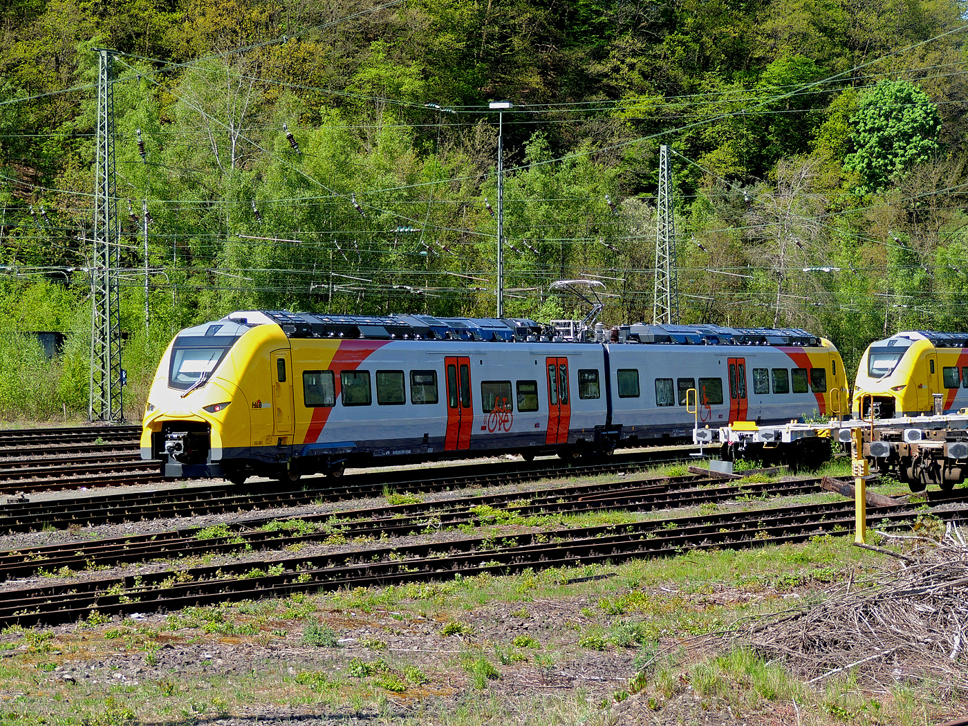 Das ist der neue Klimaschutz am Westerwald....
Zwei der drei neuen zweiteiligen Hybridtriebzüge (E/Akku) der BR 563 vom Typ SIEMENS Mireo Plus B der HLB (Hessische Landesbahn GmbH) sind am 30 April 2025 in Betzdorf/Sieg abgestellt. Links der 563 801/563 901 (94 80 0563 801-0 D-HEB / 94 80 0563 901-8 D-HEB) und rechts daneben der 563 803/563 903 (94 80 0563 803-6 D-HEB / 94 80 0563 903-4 D-HEB)

Die beiden zweiteiligen SIEMENS Mireo Plus B wurden 2024 von SIEMENS in Krefeld gebaut. 

Auszug aus der Pressemitteilung der HLB:
Alternative Antriebe im Norden von Rheinland-Pfalz: Durchbruch beim Pilotprojekt mit Batteriezügen im Westerwald / Zuschlag an Siemens Mobility für Mireo Plus B Fahrzeuge

Als Aufgabenträger für den Nahverkehr auf der Schiene im Norden von Rheinland-Pfalz setzt sich der SPNV-Nord gemeinsam mit seinen Projektpartnern von Bund, Land und Eisenbahnverkehrsunternehmen (EVU) für den Einsatz von alternativen Antrieben als Abkehr vom Dieselbetrieb ein.

Dabei konnte bereits im letzten Jahr für die Beschaffung der Fahrzeuge eine Unterstützung aus dem Förderprogramm des Bundesministeriums für Digitales und Verkehr (BMDV) für alternative Antriebe gewonnen werden.

Als Besonderheit sollen im SPNV-Nord erstmalig die beiden Antriebstechnologien für die Dekarbonisierung des Schienenverkehrs, Wasserstoff und Batterieelektrik, nebeneinander im mehrjährigen Fahrgastbetrieb zum Einsatz kommen mit einer vollständigen Rückfallebene mit Dieselfahrzeugen.

Das betrifft auch den Pilotbetrieb mit drei batterie-elektrischen Fahrzeugen im Westerwald, der zum Fahrplanwechsel im Dezember 2025 geplant ist. Dieser sieht einen Fahrzeugeinsatz auf der RB 90 Limburg – Au – Siegen (Oberwesterwaldbahn und Siegstrecke) und auf der RB 29 Limburg – Siershahn (Unterwesterwaldbahn) durch die Hessische Landesbahn (HLB) vor. Bei diesem Pilotprojekt wurde jüngst ein wichtiger Durchbruch erzielt:

Als Ergebnis der von der HLB dafür durchgeführten Fahrzeugausschreibung hat Siemens Mobility jetzt den Zuschlag für drei zweiteilige Mireo Plus B Batteriezüge erhalten. Das Fahrzeug mit seiner hohen Antriebsleistung ist für den anspruchsvollen Einsatz im Westerwald bestens geeignet. Der geplante Einsatz der drei Batteriezüge auf den Linien RB 90 und RB 29 umfasst eine Jahresfahrleistung von fast 400.000 Zug-km und ersetzt drei Dieselfahrzeuge. Da die HLB emissionsfreien Bahnstrom bezieht, werden jährlich fast 1.150 Tonnen CO2 eingespart. Der Betrieb der Batteriefahrzeuge erfordert keine neue Infrastruktur, denn die Wendezeiten in Limburg von über 20 Minuten auf der RB 29 werden für die Aufladung der Fahrzeuge ausreichend sein. Bei den auf der RB 90 verkehrenden Batteriefahrzeugen erfolgt dies im elektrifizierten Abschnitt zwischen Au und Siegen. Die Oberwesterwaldbahn (Limburg – Au) ist mit der Länge von rund 75 km und der zu überwindende Höhe von ca. 350 m derzeit in Deutschland die anspruchsvollste Strecke für den vorgesehenen Einsatz von Batteriezügen.

Die Ausschreibung der Batteriefahrzeuge war so ausgestaltet, dass die Hersteller die Möglichkeit hatten, die Fahrzeuge in laufende Bestellungen zu integrieren, so dass eine schnelle Lieferzeit in Aussicht gestellt wurde.

Siemens Mobility baut für den Einsatz im Westerwald drei zweiteilige Mireo Plus B Batteriezüge, die durch jeweils drei Türen pro Seite einen schnellen Ein- und Ausstieg ermöglichen. Die Züge verfügen für den Betrieb unter Oberleitung und zum Aufladen der Batterien über einen Stromabnehmer und verkehren auf den nicht-elektrifizierten Strecken im Batteriebetrieb. Die geräumigen Fahrzeuge bieten den Fahrgästen 126 Sitzplätze und 156 Stehplätze und sind mit einer speziellen Einstiegshilfe ausgestattet, die mobilitätseingeschränkten Menschen das Bahnfahren erleichtert.

Die neuen Batteriezüge werden auf der Oberwesterwaldbahn Limburg – Altenkirchen - Au - Siegen, und auf der Unterwesterwaldbahn zwischen Limburg – Montabaur – Siershahn unterwegs sein. Die Strecke der OWB beträgt ca. 115 km, davon sind ca. 75 km ohne Fahrdraht. Es ist vorgesehen die Züge in Limburg und auf dem Teilabschnitt Au – Siegen nachzuladen. Auf der UWB beträgt die nicht elektrifizierte Strecke ca. 35 km. Damit ist ein Zugbetrieb hin und zurück ohne Nachladen möglich. Insgesamt werden die Züge über 50 Bahnhöfe anfahren.

TECHNISCHE DATEN:
Spurweite: 1.435 mm
Achsfolge: Bo’-2’-Bo’
Fahrzeuglänge über Kupplung: 46.560 mm
Drehzapfenanstand: 2 x 17.930 mm
Anzahl der Türen je Seite: 3
Installierte Leistung: 1.700 kW
Leistungsübertragung: elektrisch
Motoren: 2 Drehstrom-Asynchronmotoren
Höchstgeschwindigkeit: 140 km/h 
Kupplung: Mittelpufferkupplung Schaku Typ 10
kleinster befahrbarer Gleisbogen: R 150 m (Normal) / R 100 m (Werkstatt)

Ein kleiner Nachteil gegenüber den LINT-Dieseltriebzügen ist mir aufgefallen, die Gesamt-Fensterfläche ist geringer. Ich bin aber sehr gespannt auf den Betriebseinsatz und wie es läuft.
