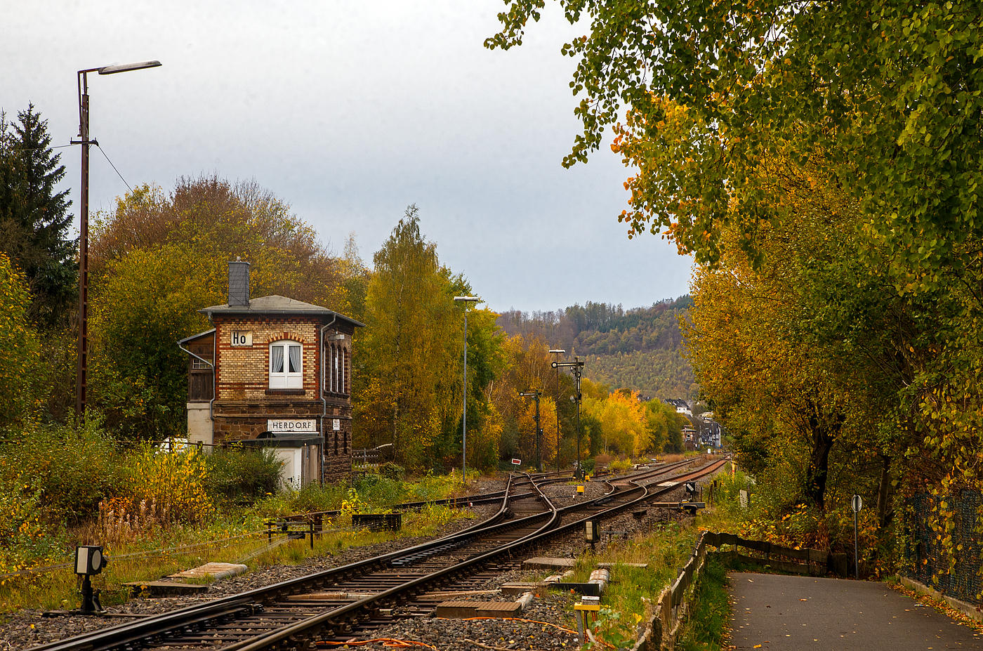 Das1901 gebaute mechanische Weichenwärter Stellwerk Herdorf Ost (Ho), an der Bahnstrecke Betzdorf - Haiger (KBS 462 „Hellertalbahn“), hier am 03.11.2022. 

Ja, in Herdorf gibt es immer noch den Luxus von zwei in Betrieb befindlichen Stellwerken, hier links das Weichenwärter Stellwerk Herdorf Ost (Ho) und weiter hinten das ca. 600 m entfernte Stellwerk Herdorf Fahrdienstleiter (Hf). Dazwischen der eigentliche Bereich vom Bahnhof Herdorf (Empfangsgebäude ist rechts von den Gleisen nicht im Bild). Neben meinem Standort, befindet sich die Weiche zur Anschlussstelle KSW (ex Freien Grunder Eisenbahn), so ist diese hier in meinem Rücken.

Da die Stellwerkstechnik in Herdorf noch rein mechanisch ist, werden beide noch benötigt, bzw. ein Umbau auf ein Stellwerk ist wohl zu aufwendig.