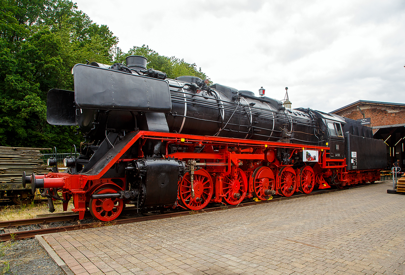 Der „Jumbo“ bzw. die schwere kohlegefeuerte Dreizylinder-G�terzug-Dampflokomotive 44 508, ex DB 044 508-0, am 02.07.2023 ausgestellt beim Lokschuppen vom Erlebnisbahnhof Westerwald der Westerw�lder Eisenbahnfreunde 44 508 e. V. hier war Lokschuppen-/Sommerfest.

Seit der meiner letzten Ablichtung am 05.05.2018 von ihr, siehe http://hellertal.startbilder.de/bild/deutschland~museen-und-ausstellungen~westerwaelder-eisenbahnfreunde-wef-44-508-e-v/610219/man-sieht-es-sehr-deutlich-der.html , hat sich aber viel getan, die Treib- und Kuppelstangen fehlen aber noch. 

Die Lok ist Eigentum vom DB-Museum und eine Leihgabe an die Eisenbahnfreunde, die nach ihr ihren Verein genannt haben. Wie man sieht, gibt es noch viel zu tun bis sie wieder im alten Glanz erstrahlt.

Die Dampflokomotive 44 508 wurde im Jahr 1941 von der Lokomotivfabrik Krauss-Maffei in M�nchen unter der Fabriknummer 16113 gebaut und an die DR geliefert. Nach dem Krieg blieb sie im Westen und wurde so 1949 als 44 508 in den Bestand der Deutsche Bundesbahn aufgenommen, mit der Einf�hrung des EDV-Nummernschemas wurde sie zum 01.01.1968 in 044 508-0 umgezeichnet. Seit Mitte der 1950er Jahre ist sie gekuppelt mit dem 2'2'T34 Tender der ex �BB 44 1561 (Borsig Lokomotiv-Werke GmbH, Hennigsdorf-Berlin, Baujahr 1940, Fabriknummer 15400). Bis zu ihrer Au�erdienststellung im Mai 1977, im BW Gelsenkirchen-Bismarck legte sie eine Strecke von �ber 1.9 Millionen Kilometern zur�ck.

Die Maschine verf�gt �ber ein Drei-Zylinder-Triebwerk, f�nf Antriebsachsen und einen Schlepptender, in dem sie 10 Tonnen Kohle und 34 Kubikmeter Wasser mitf�hren kann. Sie erreicht eine maximale Leistung von 1.910 PS bei einem Dienstgewicht von 160 Tonnen. 

Die 44 508 wurde im Mai 1977 beim Bahnbetriebswerk Gelsenkirchen-Bismarck au�er Dienst gestellt. Die 44 508 ist eine der letzten erhaltenen Dampflokomotiven ihrer Bauart. Sie wurde im Jahr 1987 durch eine Freizeitgruppe des Bahn-Sozialwerkes (BSW) �bernommen. Damit begann die museale Aufarbeitung der Lok, die im Jahre 2002 jedoch unterbrochen wurde, als das Domizil in Siershahn ger�umt werden musste. Der Verein Westerw�lder Eisenbahnfreunde �bernahm diese Dampflokomotive als Leihgabe des DB Museums, auch wenn sie nie im Westerwald eingesetzt war. 

Um das hohe ehrenamtliche Engagement und die damit verbundene immense Zahl von bereits geleisteten Arbeitsstunden zu w�rdigen, soll sie im Erlebnisbahnhof Westerwald weiterhin �u�erlich aufgearbeitet werden und einen Ehrenplatz im Museum erhalten.

Die Lokomotiven der Baureihe 44 der Deutschen Reichsbahn waren schwere, f�nffach gekuppelte G�terzug-Einheitsdampflokomotiven der Gattung G 56.20 mit Drillingstriebwerk. Sie waren vorgesehen f�r die Bef�rderung von G�terz�gen bis 1.200 t auf Mittelgebirgsstrecken und 600 t �ber Steilrampen.

Im Jahr 1926 wurden 10 Prototypen gebaut, denen 1932 zwei weitere folgten. Die Serienfertigung der Baureihe 44 begann erst 1937, nachdem ihr Weiterbau anstelle der Zwei-Zylinder�Lokomotiven der Baureihe 43, die parallel zur 44 entwickelt und gebaut worden war, beschlossen wurde. Die Baureihe 44 wurde dagegen als Drei-Zylinder-Lokomotiven ausgebildet, wobei der dritte Zylinder im Rahmen unter der Rauchkammer angeordnet ist. Die gro�en Leistungsreserven und ihre ausgezeichnete Laufruhe wogen den Nachteil der schwierigen Unterhaltung des im Rahmen schlecht zug�nglichen dritten Triebwerkes mehr als auf. So verwundert es nicht, dass die letzte Dampflokomotive, die bei der Deutschen Bundesbahn in Betrieb war, der Baureihe 44 angeh�rte. Es handelt sich um 44 903 �l, die am 26.10.1977 in Emden au�er Dienst gestellt wurde.

TECHNISCHE DATEN:
Gebaute St�ckzahl: 1989
Bauart  1'E h3
Gattung:  G 56.20
Spurweite:  1435 mm (Normalspur)
L�nge �ber Puffer:  22.620 mm
H�he:  4.550 mm
Fester Radstand:  3.400 mm
Gesamtradstand:  9.650 mm
Dienstgewicht:  169,8 t (mit Tender)
Radsatzfahrmasse:  19,8 t
H�chstgeschwindigkeit: 80 km/h (r�ckw�rts nur 50 km/h)
Leistung:  1.910 PS (1.405 kW) bei Lok mit �lfeuerung 2.100 PS
Treibraddurchmesser:  1.400 mm
Laufraddurchmesser vorn:  8.50 mm
Zylinderanzahl:  3
Zylinderdurchmesser:  550 mm
Kolbenhub:  660 mm
Kessel�berdruck:  16 bar
Rostfl�che:  4,55 m�
�berhitzerfl�che:  100,00 m�
Verdampfungsheizfl�che:  237,67 m�
Bremse:  selbstt�tig wirkende Einkammer-Druckluftbremse Bauart Knorr
Steuerung:  Bauart Heusinger
Tender: 2´2´T34
Kohlenvorrat:  10 t
Wasservorrat: 34 m�