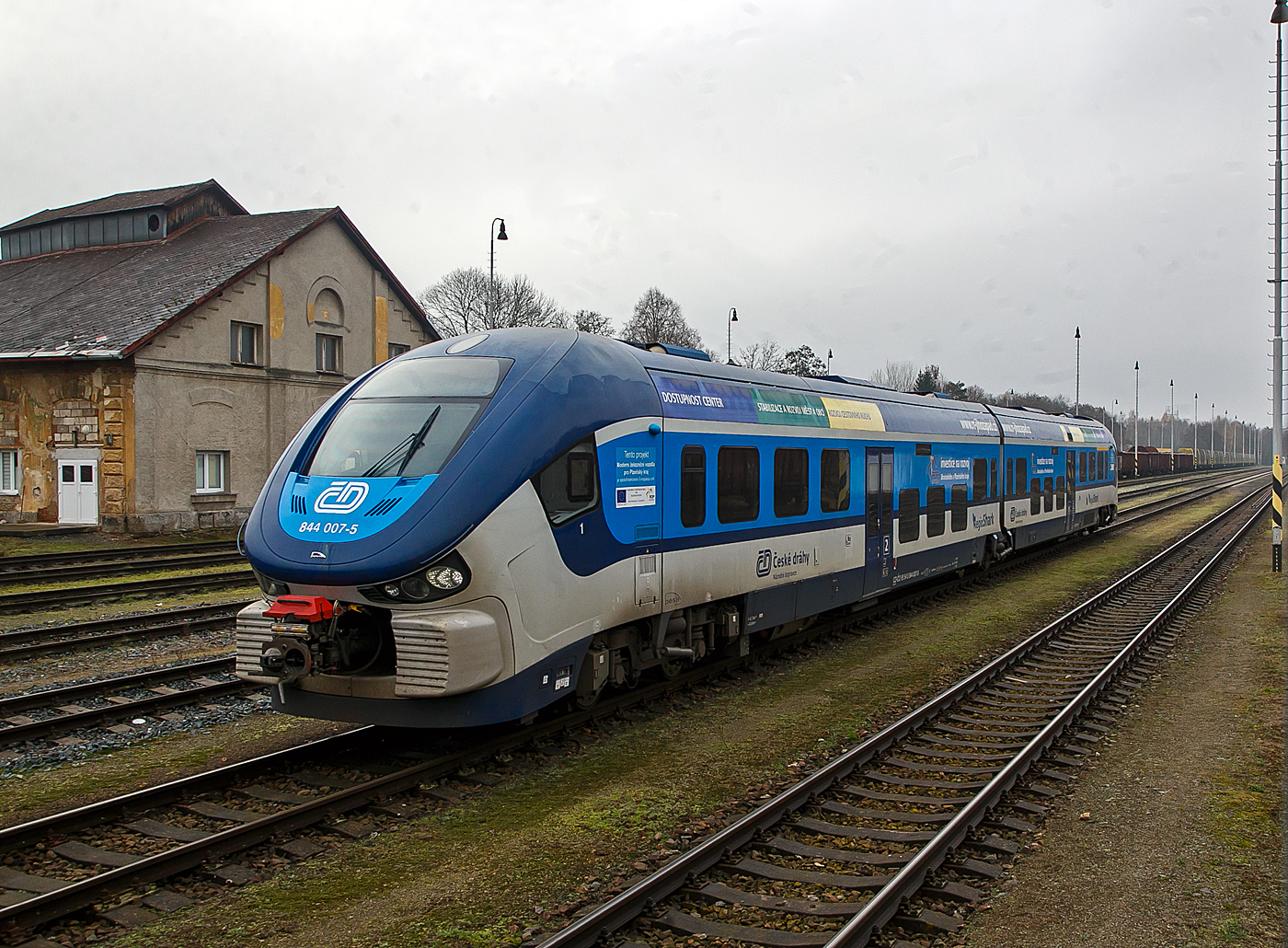 Der „RegioShark“  ČD 844 007-5 (CZ- ČD 95 54 5 844 007-5), ein Dieseltriebzug vom Typ PESA LINK II (Projektname DMU 120), steht am 22.11.2022 beim Bahnhof Doma�lice (Taus).

Die Fahrzeuge setzen sich aus zwei weitgehend identischen H�lften zusammen, die �ber ein nicht angetriebenes Jakobsdrehgestell verbunden sind. Angetrieben werden die beiden �u�eren Drehgestelle �ber zwei MTU-Powerpacks, vom Typ MTU 6H 1800 R85 mit je 390 kW Leistung, die unter dem Wagenfu�boden angeordnet sind. Die Leistungs�bertragung erfolgt jeweils mittels hydromechanischen Getriebe auf jeweils beide Achsen der Triebdrehgestelle. Bei Strecken mit Steigung h�rt man im Innenraum sehr stark wie die Motoren arbeiten m�ssen, ansonsten sind die Fahrzeuge aber sehr Laufruhig.

Zwischen den Drehgestellen ist der Fahrgastraum niederflurig ausgef�hrt, sodass an Bahnsteigen mit einer H�he von 550 Millimetern �ber Schienenoberkante ein barrierefreier Einstieg gew�hrleistet ist. Der Fahrgastraum ist klimatisiert. 

TECHNISCHE DATEN:
Anzahl: 31 Hersteller:  PESA, Bydgoszcz, Polen
Spurweite:  1.435 mm (Normalspur)
Achsformel: B'2'B'
L�nge �ber Kupplung:  43.730 mm
Achsstand im Drehgestell:  2.100 mm
H�he:  4.185 mm
Breite: 2.900 mm
Dienstgewicht: 84,4 t
H�chstgeschwindigkeit: 120 km/h
Motoren: 2 St�ck MTU Unterflur-Powerpack  6H 1800 R85L
Installierte Leistung: 2 x 390 kW
Leistungs�bertragung: hydromechanisch (Voith-Diwa-Getriebe)  
Kupplungstyp: Scharfenberg
Sitzpl�tze: 120
