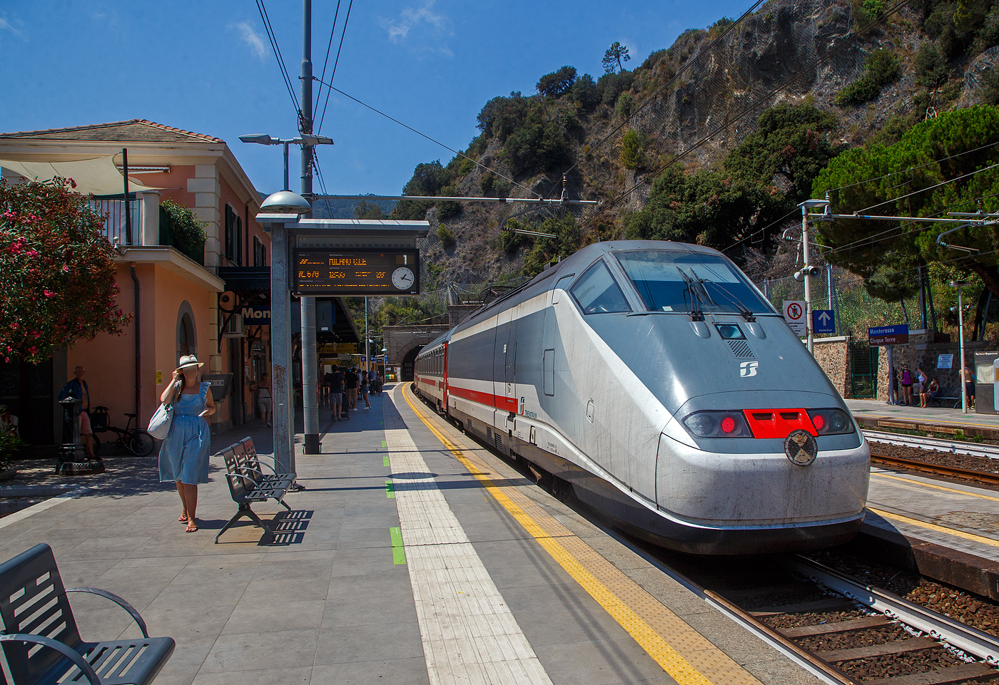Der Bahnhof Monterosso Cinque Terre (komplette Bezeichnung der Gemeide Monterosso al Mare) an der Italienischen Riviera. Von den den Cinque Terre Bahnh�fen hat Monterosso die l�ngsten Bahnsteige unter freiem Himmel, so halten hier auch Intercity-Z�ge. 

Das Fischerdorf Monterosso al Mare ist das n�rdlichste Dorf und mit rund 1700 Einwohnern der gr��te Ort der Cinque Terre an der Italienischen Riviera. Monterosso erstreckt sich �ber rund 1,5 Kilometer und ist zweigeteilt, die kleine Altstadt ist vom neueren Viertel Fegina durch einen ins Meer ragenden Felsen getrennt, auf dem sich der markante Wachtturm Torre Aurora aus dem 16. Jahrhundert erhebt. Durch den Felsen f�hrt ein rund 100 m langer Fu�g�ngertunnel.

Hier verl�sst am 22.07.2022 gerade, im Sandwich zweier E.414 (ehemalige Triebk�pfe E.404 A der ersten ETR 500 – Monotensione), der Trenitalia InterCity IC 670 (Livorno – Pisa - La Spezia - Monterosso - Genova - Milano Centrale), den Cinque Terre Bahnhof Monterosso.