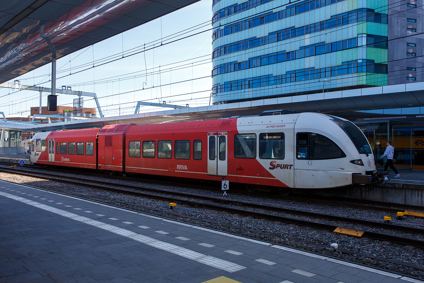 Der diesel-elektrische Stadler GTW 2/6 - Spurt 10.264 „Alfred Mozer“ der Arriva Nederland steht am 29 April 2025 im Bahnhof Arnhem Central (Arnheim Hbf), als Stoptrein RS33 nach Tiel, zur Abfahrt bereit. 

Der dieselelektrische Triebzug vom Typ Stadler GTW 2/6 der 4. Generation wurde 2012 von Stadler Rail im Werk Bussnang (Schweiz) gebaut.

GTW ist eine Leichtbau-Fahrzeugfamilie, die sich nicht nur �u�erlich in unterschiedlichen Stirnfronten von eckig bis stromlinienf�rmig (wie hier bei der 4. Generation) unterscheidet und in verschiedenen Zusammenstellungen und Antriebsvarianten lieferbar ist, sondern auch in verschiedenen Spurweiten sowie als Zahnradbahnfahrzeug, wobei die Normalspurversionen UIC-konforme Vollbahnfahrzeuge sind. Das Grundkonzept des GTW ist eher unkonventionell: Ein mittiges Antriebsmodul, auch Antriebscontainer genannt, sorgt mit seinen beiden angetriebenen Achsen f�r den Antrieb des Triebzugs. Zwei leicht gebaute Endmodule mit je einem Drehgestell und Niederflureinstieg st�tzen sich auf das Antriebsmodul ab, was ein g�nstiges Traktionsgewicht bewirkt.

Das Konzept der GTW ergibt eine sehr gute Raumausnutzung der Endmodule. Au�er �ber den Drehgestellen und an den aufgest�tzten Enden sind die GTW niederflurig ausgef�hrt (�ber 65 % Niederfluranteil). Durch Einf�gen eines Mittelwagens, ebenfalls mit nur einem Drehgestell, kann ein GTW 2/6 zum GTW 2/8 ausgebaut werden. Statt des Mittelwagens kann aber auch ein weiteres Antriebsmodul eingef�gt werden. Beim GTW 4/8 wurde zwischen den zwei benachbarten Modulen ein laufwerkloses Mittelteil eingeh�ngt. Wenn zwei GTW 2/6 miteinander verbunden werden und zwei F�hrerst�nde wegfallen, entsteht ein GTW 4/12. F�r betriebliche Flexibilit�t k�nnen bis zu vier GTW gleicher Bauart gekuppelt und �ber die Vielfachsteuerung gemeinsam gesteuert oder ein antriebsloser, einem Endwagen �hnelnder Steuerwagen mit der Achsformel 2’2’ mitgef�hrt werden.

Fahrzeuge der Arriva Nederland:
Die Arriva Nederland besitzt 96 GTW 2/6 bzw. 2/8 die zwischen 2006 und 2016 von Stadler in Bussnang (Schweiz), als diesel-elektrische bzw. elektrische (DC) Fahrzeuge gebaut, wurden. Bei den ab 2012 gebauten diesel-elektrischen GTW wurde zur Vergr��erung der Beinfreiheit die Raumaufteilung im Niederflurbereich angepasst. Grunds�tzlich entsprechen die Fahrzeuge den bereits seit 2006 an Arriva gelieferten Fahrzeugen. Sie verf�gen jedoch �ber einen neu entwickelten Antrieb mit Deutz- statt MAN-Motoren.

2005 bestellte Arriva f�r die Bedienung der niederl�ndischen Provinzen Friesland und Groningen 22 Diesel-GTW 2/6 und 29 Diesel-GTW 2/8, davon sind 8 f�r den Einsatz nach Deutschland ausger�stet. Die Z�ge mussten in nur 29 Monaten gebaut und geliefert werden. Weil damals in den Niederlanden die versch�rften Crashnormen bereits in Kraft waren, mussten die Endwagenk�sten mit F�hrerkabine neu entwickelt werden. Zus�tzlich zur Druckfestigkeit von 1.500 kN wurde der Wagenkasten auf eine Versagenslast von 3.000 kN und das Energieabsorptionsverm�gen bei einer Kollision von rund 900 kJ auf 2100 kJ erh�ht. Die Frontstruktur und die Seitenw�nde der Wagenk�sten wurden mit den Flirt-Wagenk�sten vereinheitlicht, wobei seither eine integrale, komplette geschwei�te Bauweise mit Aluminium-Strangpressprofilen zur Anwendung kommt. Damit wird eine h�here Stabilit�t der Rohbaustruktur erreicht. Zur Vereinfachung der Zulassungen sind die meisten sicherheitsrelevanten Funktionen in Relais-Technik realisiert.

2007/08 erhielt auch Veolia Transport Niederlande zwei- und dreiteilige Diesel-GTW, die weitgehend denen von Arriva entsprechen. Nach den Lieferungen der Diesel-GTW an Arriva und Veolia gewannen beide Unternehmen auch Ausschreibungen f�r mit 1.500 Volt Gleichspannung elektrifizierte Strecken. Die daf�r gelieferten GTW sind mit Stromrichtern ausgestattet, die auf Basis der 3-kV-Flirt-Stromrichter entwickelt wurden. Die elektrischen und dieselbetriebenen Z�ge von Veolia verkehren in gemischter Mehrfachtraktion. Dazu sind alle Z�ge mit Schaltern sowohl f�r den Dieselmotorstart als auch f�r Hauptschalter und Stromabnehmer ausgestattet.
Antrieb mit Dieselmotoren (diesel-elektrisch):
Die GTW mit Dieselantrieb der ersten Generation wurden mit einem Zw�lfzylinder-V-Motor des Typs 83-TD13 von MTU Friedrichshafen mit 550 kW Nennleistung ausgestattet. Wegen der Breite des Zw�lfzylindermotors musste der Durchgang durch das Antriebsmodul asymmetrisch angeordnet werden. 

Bei der zweiten Generation wurden zwei schnelllaufende, wassergek�hlte Sechszylinder-Lkw-Reihenmotoren mit je 390 kW Nennleistung von MAN eingebaut, die die strengen Euro-3-Abgasvorschriften im Stra�enverkehr erf�llen. Die Beschaffung von in gro�en Mengen produzierten Lkw-Motoren ist zudem kosteng�nstiger als von speziellen Dieselmotoren f�r Schienenfahrzeuge. Die beiden nun v�llig getrennten Antriebsaggregate bieten eine gr��ere Leistung als der MTU-Motor und den Vorteil der Redundanz, so dass bei St�rungen mit einem Aggregat weitergefahren werden kann. Die beiden Dieselmotoren sind auf beiden Seiten des Antriebmoduls angeordnet und erlauben einen symmetrischen Durchgang von einem Fahrgastraum zum anderen.

Die 2012 f�r Arriva Gelderland beschafften Fahrzeuge (wie diese hier) erhielten je zwei neuentwickelte Deutz-Dieselmotoren vom TCD 16.0 V8. Der wassergek�hlter 8-Zylinder Motor in V-Ausf�hrung (90�) mit Common Rail Einspritzsystem, Turboaufladung und Ladeluftk�hlung mit einer Leistung von 520 kW erf�llt die Abgasnormen EU Stufe V / US Tier 4. Bei einer Drehzahl von 1.400 U/min erbringt der Motor ein maximales Drehmoment von 2.890 Nm.
Weitere Motordaten:
Hubraum: 15.9 l (Bohrung � 123 mm x 140 mm Hub)
Leistung: 520 kW (697 PS) bei 2.100 U/min
Max. Drehmoment: 2.890 Nm bei 1.400 U/min
Leerlaufdrehzahl: min. 600 U/min
L�nge x Breite x H�he: 1.150 x 945 x 1.170 mm
Gewicht (trocken): 1.260 kg

Die redundante Antriebsausr�stung besteht aus 2 Antriebsstr�ngen mit je 1 Dieselmotor, Asynchrongenerator, IGBT-Stromrichter und Asynchronfahrmotor

TECHNISHE DATEN der GTW 2/6:
Spurweite: 1.435 mm (Normalspur)
Antriebsart: dieselelektrisch
Achsfolge: 2'Bo'2'
Inbetriebsetzung: 2006-2016
L�nge �ber Kupplung 40.890 mm
Fahrzeugbreite 2.950 mm
Fahrzeugh�he 4.035 mm
Fu�bodenh�he: Niederflur 830mm / Hochflur 996 mm
T�ren je Seite: 2 je 1.300 mm breit
Dienstgewicht (tara): ca. 68 t
Achsabstand im Drehgestell: 2.100 mm
Triebraddurchmesser: 860 mm (neu)
Laufraddurchmesser: 750 mm (neu)
Max. Leistung am Rad: 600 kW 
Anfahrzugkraft: 80 kN
H�chstgeschwindigkeit: 140 km/h
Sitzpl�tze in der 2. Kl.:  92 (Sommer Layout) /100 (Winter Layout)
Sitzpl�tze in der 1. Kl.:  8
Klappsitze: 18 (Sommer Layout) / 11 (Winter Layout)
Sommer Layout bedeutet das mehr Platz f�r Fahrr�der vorhanden ist.

Abweichende TECHNISHE DATEN der GTW 2/8:
Achsfolge: 2’2’Bo’2’
L�nge �ber Kupplung 55.937 mm
T�ren je Seite: 3 je 1.300 mm breit
Dienstgewicht (tara): ca. 87 t
Sitzpl�tze in der 2. Kl.: 148 (Sommer Layout) /156 (Winter Layout)
Sitzpl�tze in der 1. Kl. 16
Klappsitze: 21 (Sommer Layout) / 14 (Winter Layout)
