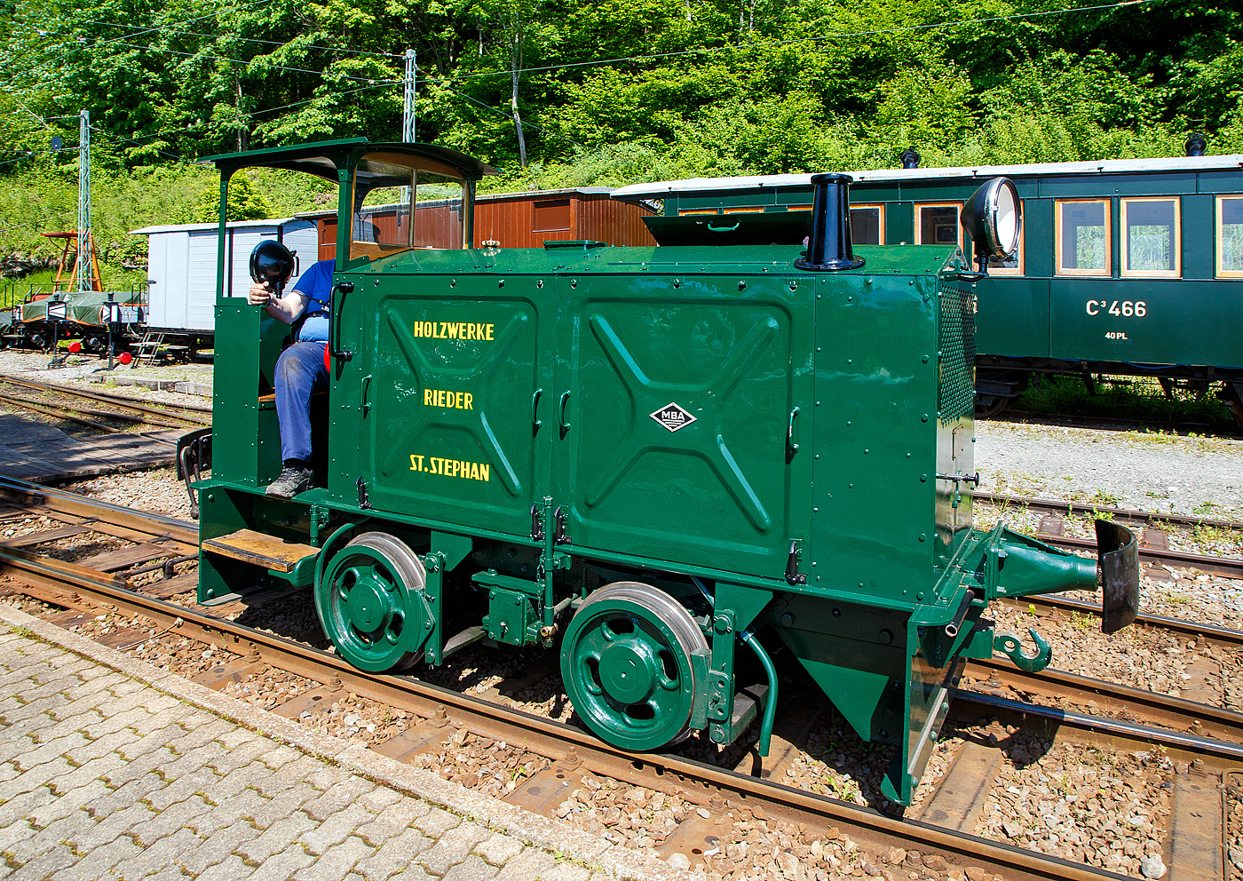 Der doch recht kleine ex MOB Schienentraktor Tm 2/2 Nr. 1, ex Holzwerk Rieder, der Museumsbahn Blonay-Chamby hat am 27 Mai 2023 im Museumsareal in Chaulin die Rangierarbeit erledigt nun geht es wieder zur�ck in die Bereitstellung.

Die kleine Diesellok, vom Typ O&K RL 2a wurde 1931 von Orenstein & Koppel im Werk Babelsberg unter der Fabriknummer 20200 gebaut und an die Grande Dixence SA f�r die Baustelle der ersten Dixence-Staumauer  geliefert, wo sie bis 1940 im Einsatz war. Im 1941 wurde sie dann von der Firma Mauerhofer & Zubner, f�r den Einsatz von Bauz�gen beim Fahrleitungsumbau bei der MOB �bernommen. 1950 wurde die kleine Lok an das Holzwerk Rieder in St. Stephan verkauft, diese Farbgebung tr�gt sie auch aktuell bei der BC. Die Lok tr�gt Fabrikschilder der MBA, wobei die Umbenennung der O&K in Maschinenbau und Bahnbedarf Aktiengesellschaft, vormals Orenstein & Koppel (MBA) erst im Februar 1940 erfolgte.

Die MOB (Montreux-Berner Oberland-Bahn / Montreux Oberland Bernois) kaufte die Lok dann 1979 wieder zur�ck und bezeichnete sie als Tm 2/2 1. Bei der MOB wurde sie f�r Rangierarbeiten, von Zementwagen auf Rollb�cken in St. Stephan eingesetzt. Die Lok wurde 1995 von der MOB ausrangiert verbleib aber erst noch im Depot Montbovon. 2006 ging sie dann an die Museumsbahn Blonay-Chamby.

Die Lok hat einen 2-Zylinder-Orenstein & Koppel-Dieselmotor mit 22 PS (16 kW) Leistung, die Leistungs�bertragung erfolgt �ber ein Zweigang-Konuskupplungs-Wendegetriebe mit stufenloser Geschwindigkeit Regulierung, �ber zwei Rollenketten auf die vordere Achse und von dieser �ber eine Rollenkette auf die hintere Achse. Das Zweigang-Konuskupplungsgetriebe erm�glicht zwei verschiedene Geschwindigkeitsstufen f�r beide Fahrtrichtungen. Dabei laufen immer beide G�nge im Eingriff, jeweils einer wird eingekuppelt. Eine einfache Wendeschaltung im Getriebe erm�glicht den Fahrtrichtungswechsel bei Stillstand der Lokomotive. Die einfache Bauart des Getriebes hat sich schon bei den Benzinloks bew�hrt und wurde bei fast allen O&K-Loks der unteren Leistungsklassen angewendet.

TECHNISCHE DATEN:
Spurweite: 1.000 mm (Meterspur)
Achsfolge: B
L�nge �ber Puffer: 4.490 mm
Kastenl�nge: 3.450 mm
H�he: 2.270 mm
Breite: 1.240 mm
Achsabstand: 1.170 mm
Raddurchmesser : 550 mm
Eigengewicht: 7.000 kg
Leistung: 16 kW (22 PS)
H�chstgeschwindigkeit: 7 km/h
Achslager: Gleitlager

Die O&K Typenbezeichnung  RL  stand f�r  Roh�l  (= Diesel).

Anfang des 20. Jahrhunderts war es noch �blich bei und auf Gro�baustellen Feld- oder Schmalspurbahnen zu bauen und zu betreiben. Heute durch Entwicklung von moderner und oft sehr schweren Baumaschinen und Muldenkipper eigentlich undenkbar.