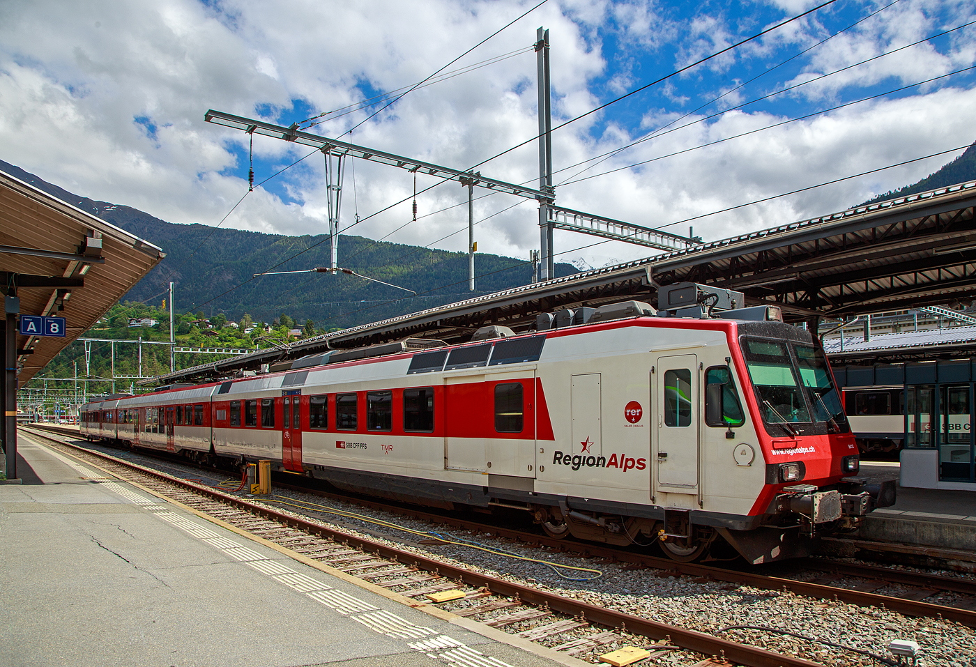 Der dreiteilige NPZ Domino RA12 der RegionAlps (ex SBB RBDe 4/4) hat am 25.05.2023 als Regio (St-Gingolph–St-Maurice –Martigny–Sion–Brig), Steuerwagen voraus, seinen Zielbahnhof Brig erreicht.

Der NPZ Domino besteht aus:
1./2. Klasse Steuerwagen ABt NPZ DO RA 50 85 39-43 948-1 CH-RA
Modernen 2.Klasse INOVA-Zwischenwagen mit Niederfluranteil B NPZ DO RA 50 85 29-43 407-0 CH-RA
und dem 
Triebwagen RBDe 560 DO RA 94 85 7 560 412-9 CH-RA, ex SBB RBDe 560 010-1 (Umbau 2009), hier rechts im Vordergrund.

Die Regionalps (RA) ist ein Eisenbahnverkehrsunternehmen im Kanton Wallis, mit Sitz in Martigny hat. Eigentümer derim Jahr 2003 gegründete Gesellschaft  sind die Schweizerischen Bundesbahnen (SBB) mit 70 %, die Transports de Martigny et Régions (TMR) mit 18 % und der Kanton Wallis mit 12 %. Die RA betreibt den Regionalverkehr vor allem im Rhonetal zwischen dem Ostufer des Genfersees und Brig. Inzwischen gehören Regionalps 16 dreiteilige NPZ Domino (Trieb-, Zwischen- und Steuerwagen ex SBB) und 4 RABe 525 NINA (ex TMR).

Als RBDe 4/4 wurden die Triebwagen der Schweizerischen Bundesbahnen (SBB) bezeichnet, die ab 1984 für die als Neuer Pendelzug (NPZ) bezeichneten Regionalzugskompositionen mit den dazugehörenden Steuerwagen angeschafft wurden. Sie tragen seit 1990 die Baureihenbezeichnung RBDe 560. Aus Kostengründen wurde damals auf die Beschaffung neuer Zwischenwagen verzichtet, verwendet werden stattdessen umgebaute Einheitswagen (EW I und EW II).

Die meisten von 1987 bis 1996 gebauten Fahrzeuge RBDe 560, 561 und 568 durchliefen 2008 bis 2013 ein Komplett-Modernisierungsprogramm. Aus aufgearbeiteten Trieb- und Steuerwagen sowie neu beschafften Zwischenwagen entstanden Regionalverkehrs-Kompositionen mit der Bezeichnung «Domino». Die Triebwagen werden dabei einheitlich als RBDe 560 (94 85 7 560 XXX-X) bezeichnet. Sie können in Vielfachsteuerung verkehren.

TECHNISCHE DATEN (Komposition RBDe 560, B und ABt) :
Spurweite:  1.435 mm (Normalspur)
Achsformel:  Bo’Bo’ +2´2´+2´2´
Länge über Puffer:  25.000 mm / 24.700 mm / 25.000 mm
Drehzapfenabstand: 17.600 mm / 18.900 mm /17.600 mm
Achsabstand im Drehgestell: 2.700 mm (ZW 2.500 mm)
Treib- und Laufraddurchmesser: 950 mm
Höhe:  3.750 mm
Breite:  2.860 mm
Dienstgewicht:  72 t (Triebwagen) + 36 t (ZW) + 38 t (Steuerwagen)
Höchstgeschwindigkeit: 140 km/h
Dauerleistung:  1.650 kW (2.250 PS)
Anfahrzugkraft:  182 kN
Dauerzugkraft: 78 kN
Anzahl Fahrmotoren: 4
Stromsystem:  Wechselstrom 15 kV 16,7 Hz
Sitzplätze: 54 (TW) / 60 (ZW) / 12+60 (SW) = 186 (12 in der 1. Klasse)
Ladegewicht: 0,3 t (Triebwagen)
Kupplungstyp: Schraubenkupplung