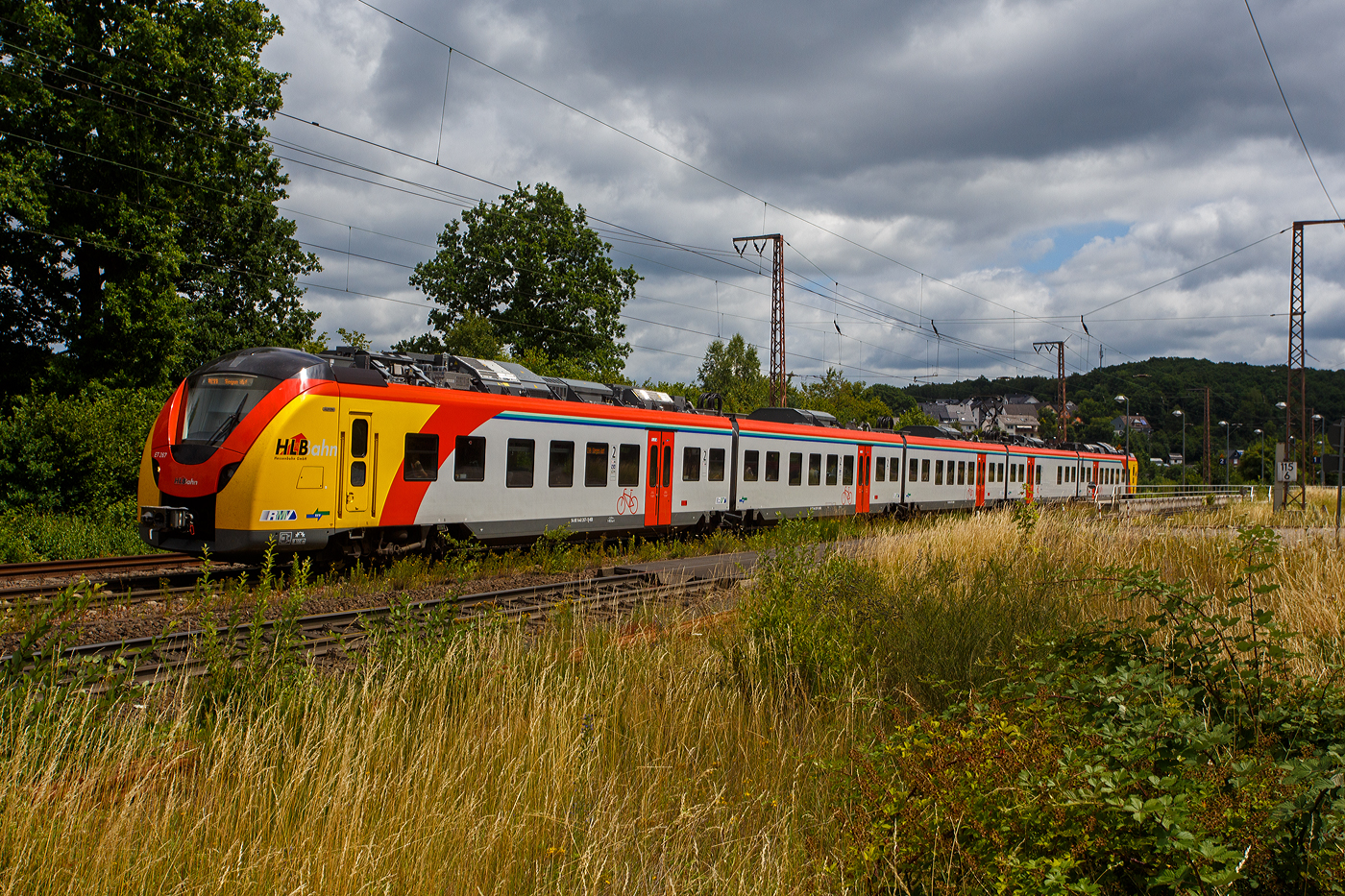 Der ET 267 (1440 267 / 1441 267 / 1841 267 / 1441 767 und 1440 767), ein fünfteiliger Niederflur-Elektrotriebwagen vom Typ Alstom CORADIA Continental 2 (XCC MHX) der HLB (Hessische Landesbahn GmbH), rauscht am 11 Juli 2025, als RE 99 „Main-Sieg-Express“ (Frankfurt/Main - Gießen - Siegen) Umlauf HLB24512, durch Wilnsdorf-Rudersdorf (Kreis Siegen) in Richtung Siegen. 

Der Elektrotriebzug wurden 2023 von der Alstom Transport Deutschland GmbH (vormals LHB) in Salzgitter-Watenstedt unter der Fabriknummer D041545-014 gebaut und an die HLB geliefert. Die Coradia Continental benötigten wegen einer neuen Steuerungssoftware eine neue Zulassung, nach Problemen mit dieser, hatte ALSTOM erst Ende April 2024 die Zulassung für die neuen Coradia Continental für die Hessische Landesbahn (HLB) erhalten und so erfolgte die Abnahme erst zum 30. April 2024.