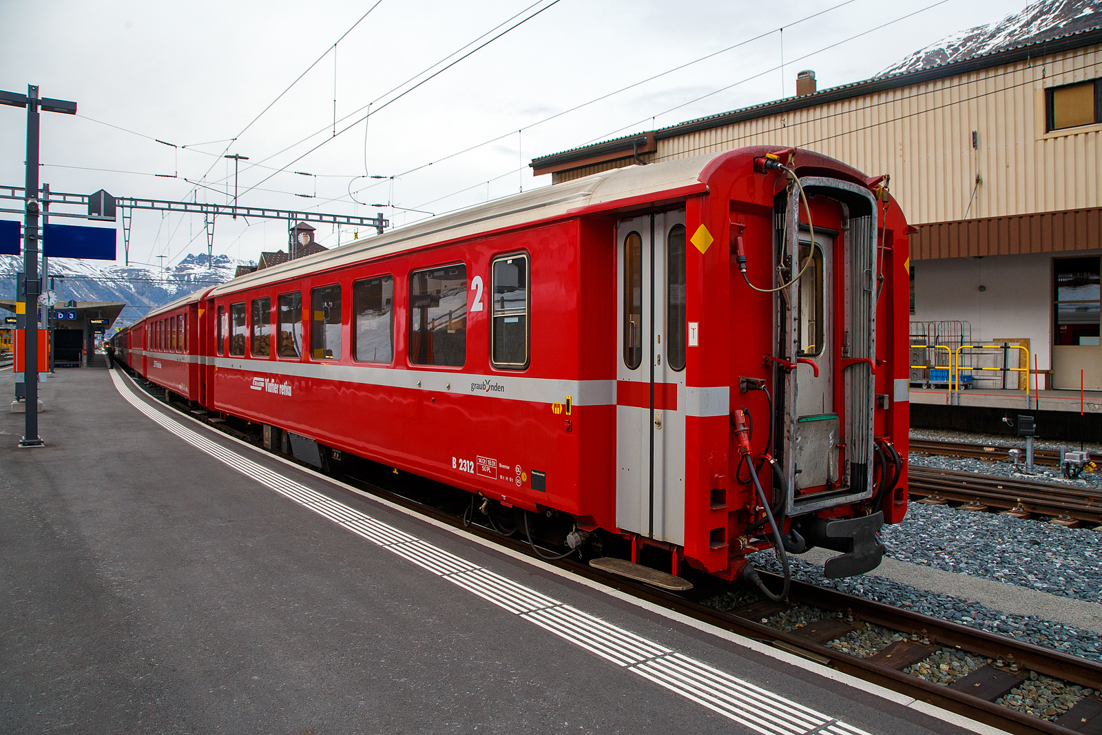 Der f�r die Berninabahn verk�rzte Einheitswagen I - 2.Klasse Reisezugwagen RhB B 2312 am 21.03.2023 im Zugverband im Bahnhof
Pontresina.

Mit mehr als 100 Fahrzeugen bilden die als Einheitswagen I bezeichneten Personenwagen bis heute die gr��te Serie im Rollmaterialbestand der RhB. Das Fahrzeugkonzept wurde Anfang der sechziger Jahre in enger Zusammenarbeit zwischen Industrie und RhB entwickelt. Als Neuheit galten damals die Einstiegsbereiche mit WC und Stauraum f�r sperriges Gep�ck an den Wagen�berg�ngen. Folglich weicht das Konzept deutlich von den Mitteleinstiegswagen aus den vierziger Jahren ab.

Die ersten von FFA und SIG gebauten Einheitswagen I wurden Ende 1963 in Betrieb genommen. In einem Zeitraum von etwa zehn Jahren wuchs der Bestand an EW I kontinuierlich. Neben den 18,42 m langen Wagen, die haupts�chlich auf dem Stammnetz eingesetzt werden, kamen auch Sonderbauformen mit Aluminiumwagenkasten hinzu. Zu diesen z�hlen auch diese auf 14,19 m verk�rzten Fahrzeuge f�r den Einsatz auf der Berninabahn.

TECHNISCHE DATEN (2.Klasse EW I, verk�rzt):
Hersteller Wagenkasten: FFA
Hersteller Drehgestelle: SWP
Inbetriebsetzung: 1968-72
Betriebsnummern: B 2307-2314 und B 2451-2460
Anzahl Fahrzeuge: 18
Spurweite: 1.000 mm
L�nge �ber Kupplung:14.910 mm
Breite: 2.650 mm
Achsabstand im Drehgestell: 1.800 mm
Drehzapfenabstand: 9.240
Gewicht: 14.000 kg
Sitzpl�tze: 50
zul. H�chstgeschwindigkeit: 90 km/h
Lauff�hig: StN (Stammnetz) / BB (Berniabahn) / MGB (Matterhorn Gotthard Bahn)
