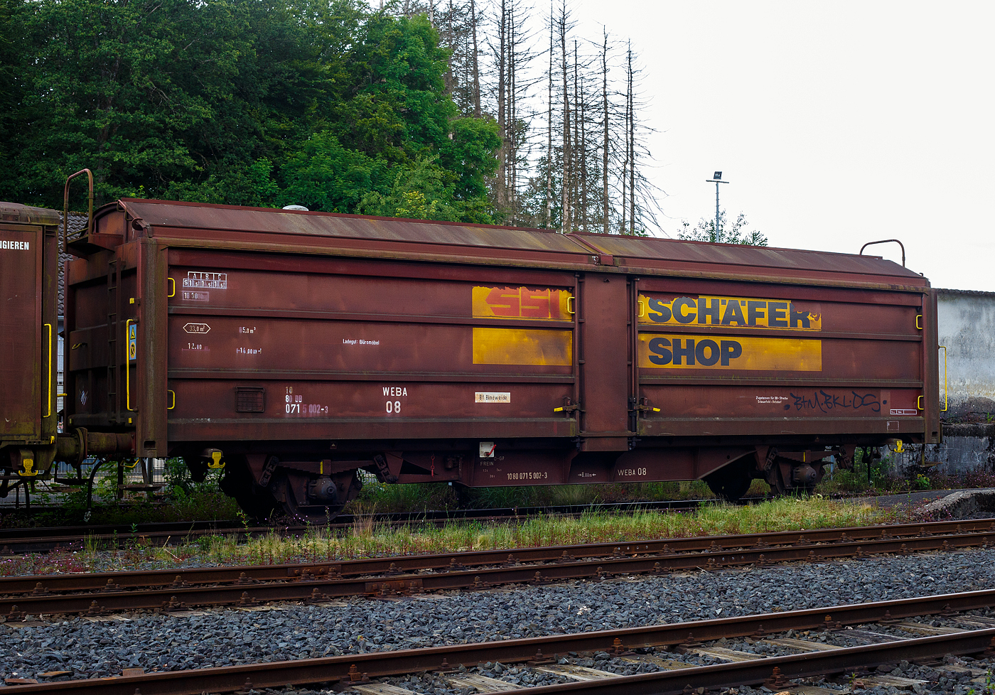 Der gedeckte zweiachsige Schiebewand-/Schiebedachwagen WEBA 08 - 10 80 0715 002-3 D-WEBA (ex 10 80 071 5 002-3 D-DB) der Gattung Tbis 869 - Bauform A (für Büromöbel der SSI Schaefer Shop GmbH) der WEBA (Westerwaldbahn des Kreises Altenkirchen GmbH) abgestellt am 16 Juni 2024 auf dem Betriebshof der Westerwaldbahn (WEBA) auf der Bindweide bei Steinebach/Sieg. Der Wagen ist auf DB-Strecke Scheuerfeld – Betzdorf(Sieg) zugelassen. 
Beschreibung:
Die Beschaffung erster Hubschiebedachwagen begann bereits 1949. Die Wagen verfügten über ein zweiteiliges Dach, von denen ein Teil über das andere geschoben werden konnte. In der Mitte des Wagens war ein der Dachform angepasstes Querjoch angebracht, um einerseits die Spur der Dachlaufwerke halten zu können, andererseits das Dach dicht verschließen zu können. Betätigt wurde das Dach durch ein an den Kopfendenden angebrachte hoch liegende Bühne, die über Leitern erreicht wurden.

Ab 1966 wurden von der DB bei der Waggonunion Siegen (eigentlich Dreis-Tiefenbach, zuvor Siegener Eisenbahnbedarf A.G.) die ersten Wagen der Gattung Tbis 869 der Bauform A beschafft. Bei dieser Bauform konnte das Dach auch nur von einer kleinen oben liegenden Bühne an den Stirnwänden geöffnet werden. Zwei Jahre später wurde die Bauform B dieser Gattung gefertigt. Hierbei war es nun möglich das Dach mittels Handräder an einer Stirnseite der Waggons zu öffnen. Es war nun nicht mehr nötig auf das Dach zu steigen und verminderte somit auch die Unfallgefahr.

Eingesetzt wurden diese Waggons für den Transport von großen nässeempfindlichen Stückgütern (bei diesem Wagen waren es später Büromöbel), durch das öffnungsfähige Dach könnte die Ladung auch mittels Kranen schnell be- und entladen werden. Von den ca. 2.000 beschafften Fahrzeugen gelangten noch gut 1.400 zur DB AG, dort wurden sie aber zügig ausgemustert und durch neuere Bauarten ersetzt. 

TECHNISCHE DATEN:
Spurweite: 1.435 mm (Normalspur)
Anzahl der Achsen: 2
Länge über Puffer :14.000 mm
Achsabstand: 8.000 mm
Eigengewicht: 18.300 kg
Ladelänge:12.800 mm
Ladefläche: 33,0 m²
Rauminhalt: 85,0 m³
Seitenwand-Türöffnung (B × H): 5.660 × 2.100 mm
Lichte Öffnung bei geöffnetem Dach: 6.000 × 2.530 mm
Fußbodenhöhe über SO: 1.200 mm
Höchstgeschwindigkeit: 100  km/h 
Maximales Ladegewicht: 18,5 t (Streckenklasse C oder höher)
Kleinster bef. Gleisbogenradius:  35 m
Bremse: Frein O-GP 
Intern. Verwendungsfähigkeit: RIV (ursprünglich)
