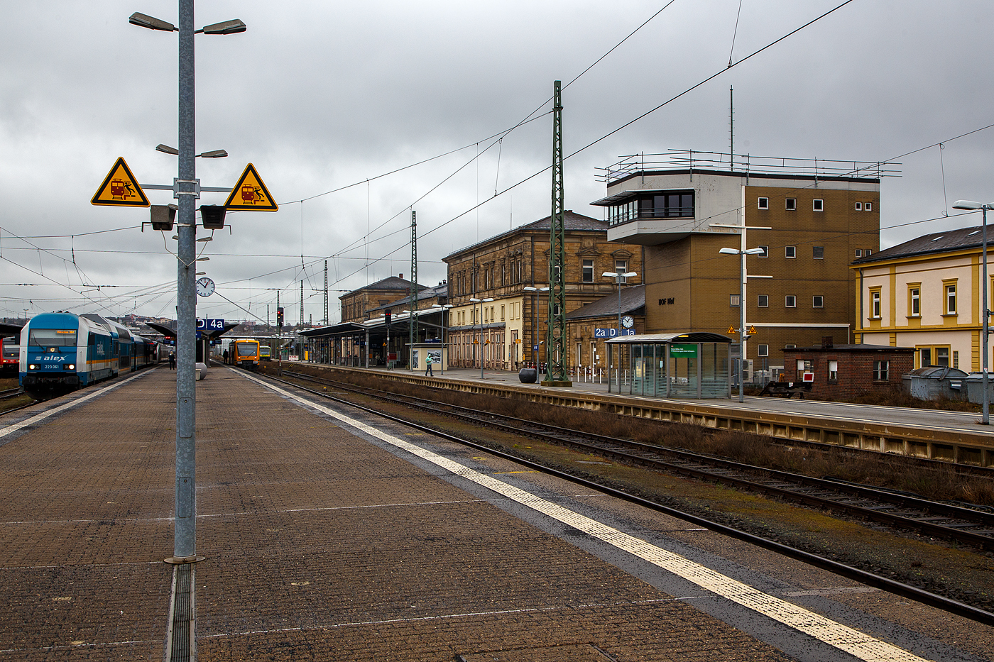 Der Hauptbahnhof Hof (offiziell Hof Hbf) am 17.04.2023, rechts das Fdl.-Stellwerk Hof Hbf. 

Der Hauptbahnhof ist der wichtigste Bahnhof der oberfr�nkischen Stadt Hof. Der Bahnhof ist seit jeher ein Eisenbahnknoten zwischen Bayern, Th�ringen, Sachsen und dem Nachbarland Tschechien. 2013 war er mit t�glich 7000 bis 8000 umsteigenden Reisenden der f�nftgr��te Umsteigebahnhof Bayerns.

Der Hauptbahnhof liegt am Schnittpunkt der Sachsen-Franken-Magistrale Dresden–Hof–N�rnberg und der Strecke Berlin–Leipzig–Hof–Regensburg–M�nchen. Bei seiner Er�ffnung 1880 war er Gemeinschaftsbahnhof an der Grenze zwischen bayerischer und s�chsischer Staatsbahn. Dies ist heute noch an der gro�en Ausdehnung der Bahnanlagen und dem imposanten Empfangsgeb�ude zu erkennen. Nach der Gr�ndung der Deutschen Reichsbahn wurde der Bahnhof etwa 25 Jahre lang zum Durchgangsbahnhof. Von 1945 bis 1990 war der Hofer Bahnhof wieder Grenzbahnhof, diesmal zwischen der Sowjetischer Besatzungszone/Deutsche Demokratische Republik und Amerikanischer Besatzungszone/Bundesrepublik Deutschland, bevor die Grenze durch die Deutsche Wiedervereinigung wegfiel. Bis 2006 war der Hauptbahnhof ein Teil des Fernverkehrsnetz der DB, ab 2030 soll es wieder eine Fernverkehrsverbindung geben.

Zum Bahnhof geh�ren ein Zentralstellwerk, ein Container-Terminal, eine Zolldienststelle und ein Bahnbetriebswerk. Fr�her gab es G�terabfertigung und einen Paketbahnhof.

Der Bahnhof bestand fr�her aus zwei Teilen, in denen jeweils alle Betriebsanlagen (Lokschuppen, Kohlenbunker, Betriebswerk, Abstellgruppen usw.) vorhanden waren. Die s�dliche Seite geh�rte den K�niglich Bayerischen Staats-Eisenbahnen, die n�rdliche Seite den K�niglich S�chsischen Staatseisenbahnen. 

Das Empfangsgeb�ude wurde durch den seit 1856 bei den K�niglich Bayerischen Staats-Eisenbahnen angestellten Architekten Georg Friedrich Seidel (1823–1895) entworfen. Es war spiegelsymmetrisch angelegt, wie der gesamte Bahnhof. Die Grenze zwischen beiden Eisenbahnverwaltungen verlief durch die Mitte des Empfangsgeb�udes. Im Empfangsgeb�ude wurde ein prunkvoller K�nigssaal eingerichtet.

Nach dem Zweiten Weltkrieg war Hof lange wieder Grenzbahnhof, n�rdlich und �stlich von Hof befand sich die innerdeutsche Grenze, die Stadt war wieder zur Schnittstelle zwischen zwei Bahngesellschaften geworden. Die H�llentalbahn wurde unterbrochen, die Bahnstrecke Hof–Eger nur noch im G�terverkehr genutzt, von der Bahnstrecke Hof–Plauen wurde als Reparationsleistung eines der beiden Streckengleise demontiert. Alle Z�ge der Deutschen Bundesbahn (mit Ausnahme der Interzonenz�ge von M�nchen und N�rnberg nach Leipzig und Dresden sowie der Transitz�ge nach Berlin) begannen und endeten in Hof. Bei den Interzonen- und Transitz�gen wurde in Hof ein Lokwechsel durchgef�hrt: In Hof wurden die Z�ge in die DDR mit Triebfahrzeugen der Deutschen Reichsbahn, Z�ge aus der DDR mit Triebfahrzeugen der Deutschen Bundesbahn bespannt. Es wurden in Hof keine Grenzkontrollen durchgef�hrt, diese fanden im Zug oder am Grenzbahnhof Gutenf�rst statt.