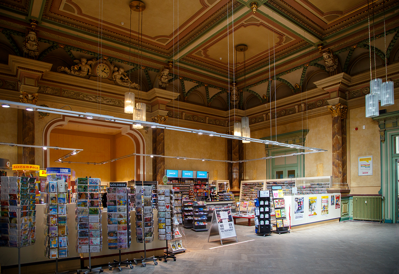 Der imposanten prunkvolle (ehemalige) K�nigssaal in der Mitte des Empfangsgeb�udes vom Hbf Hof am 21.04.2023, hier hat man Denkmalschutz und Nutzung sehr gut umgesetzt. 

Der Bahnhof bestand aus zwei Teilen, in denen jeweils alle Betriebsanlagen (Lokschuppen, Kohlenbunker, Betriebswerk, Abstellgruppen usw.) vorhanden waren. Die s�dliche Seite geh�rte den K�niglich Bayerischen Staats-Eisenbahnen, die n�rdliche Seite den K�niglich S�chsischen Staatseisenbahnen. 

Das Empfangsgeb�ude wurde durch den seit 1856 bei den K�niglich Bayerischen Staats-Eisenbahnen angestellten Architekten Georg Friedrich Seidel (1823–1895) entworfen. Es war spiegelsymmetrisch angelegt, wie der gesamte Bahnhof. Die Grenze zwischen beiden Eisenbahnverwaltungen verlief durch die Mitte des Empfangsgeb�udes. Im Empfangsgeb�ude wurde ein prunkvoller K�nigssaal eingerichtet.

Nach dem Zweiten Weltkrieg war Hof lange wieder Grenzbahnhof.