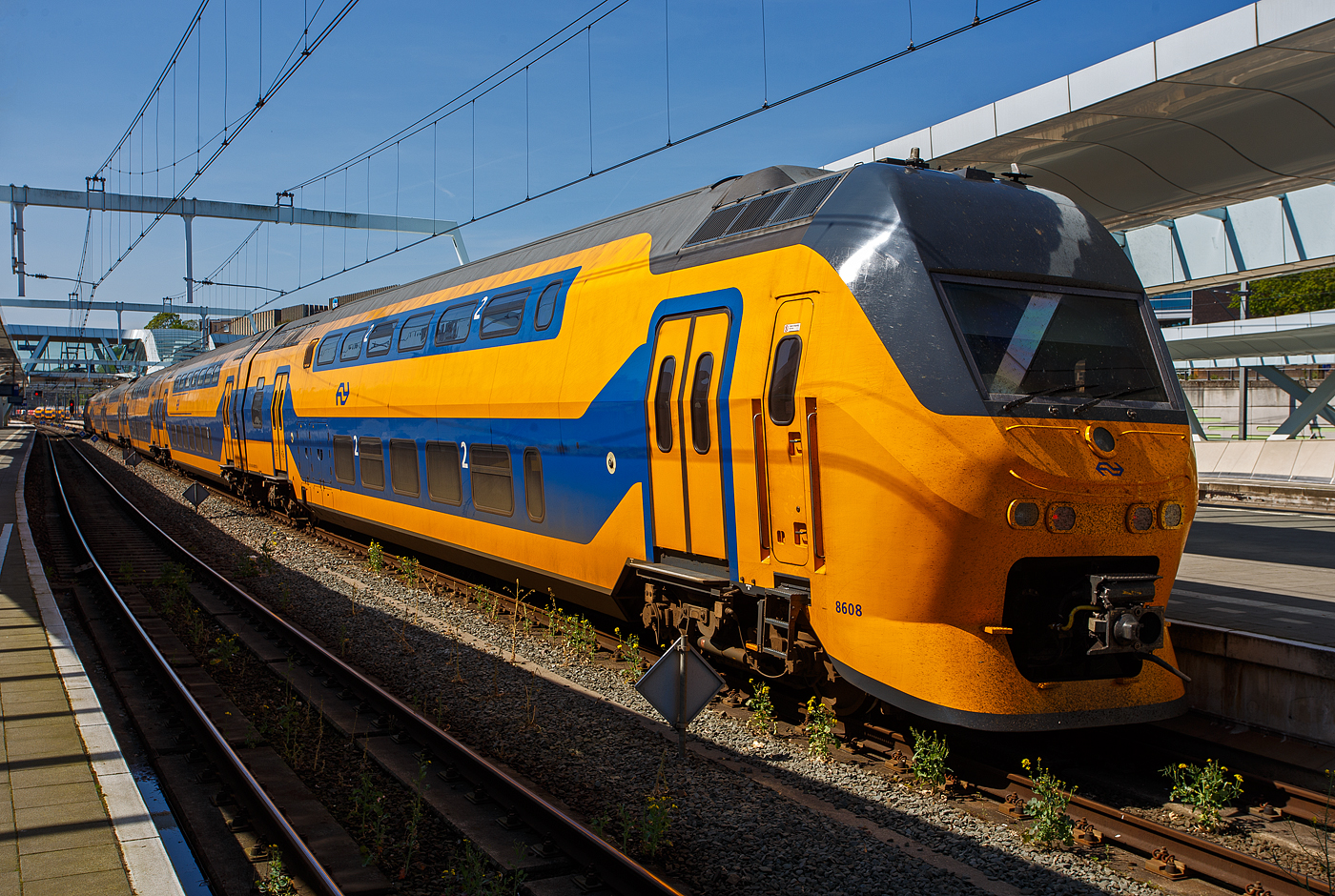 Der sechsteilige NS VIRM Regiorunner (VIRM-VI) 8608 der Nederlandse Spoorwegen N.V. (Niederl�ndische Eisenbahn AG), ex DD-IRM IV NS 8408, am 29 April 2025 im Bahnhof Arnhem Centraal (Arnheim Hbf). VIRM steht f�r Verlengd InterRegio Materieel (verl�ngerte IRM). 

In den 1980er Jahren plante die NS eine radikale Vereinfachung des Personenverkehrs-Angebots: Die bestehenden Zuggattungen sollten zu drei Gattungen, n�mlich Regionalzug (stoptrein), Interregio und Intercity zusammengef�hrt werden. F�r den Interregio sollte das erforderliche Rollmaterial neu entwickelt werden. Das Resultat war die Baureihe DD-IRM. Nach einer weiteren Vereinfachung, bei welcher die Gattung Interregio im Intercity aufging, wurde der DD-IRM zum typischen niederl�ndischen Intercity-Zug.

1994 begann die Auslieferung der neuen IRM-Z�ge. Hersteller waren die Waggonfabrik Talbot in Aachen (1995 von Bombardier Transportation aufgekauft) 34 dreiteilige und 47 vierteilige Z�ge wurden gebaut. Weil Talbot nicht gen�gend Kapazit�t hatte wurde die Fertigung von 47 Wagen Typ ABv5 bei De Dietrich Ferroviaire aus Reichshoffen (Elsass) ausgelagert. Die Drehgestelle wurden von Schweizerische Industrie-Gesellschaft (SIG) in Neuhausen am Rheinfall (CH) und Stork RMO (NL) geliefert.

Weil die Transportkapazit�ten insbesondere der dreiteiligen Z�ge bald nicht mehr ausreichten, entstand die erste Serie (VIRM-1) durch die Erweiterung des DD-IRM, der interregionalen Doppelstockausr�stung ( Regiorunner“). Umbauprogramm startete 2002 alle Dreiteiler bekamen einen zweiten Zwischenwagen verpasst und so zu vierteiligen Z�gen verl�ngert, die bisherigen Vierteiler wurden mit zwei Zwischenwagen (davon einem angetriebenen) zu Sechsteiligen Z�gen gestreckt. Bombardier fertigte die Aufbauten in seinem G�rlitzer Werk die Drehgestelle im Werk Siegen, die Umbauten fanden im ehemaligen Talbot Werk in Aachen statt. Die so umgebauten Z�ge hie�en ab nun Verlengd InterRegioMaterieel (verl�ngerte IRM): VIRM-IV als Vierteiler, VIRM-VI als Sechsteiler.

Zu den Umbauten wurden auch weitere „neue“ komplette vier- und sechsteilige VIRM-Triebz�ge gebaut. Die NS hat so nun insgesamt 178 elektrische Doppelstock-Triebz�ge VIRM, davon 98 des vierteiligen Zugtyps (VIRM-IV) und 80 des sechsteiligen Zugtyps (VIRM-VI). 

TECHNISCHE DATEN der VIRM-VI (Sechsteiler der Series 8600/8700)
Hersteller (mechanischer Teil): Bombardier Transportation, ex Talbot, Aachen Hersteller (elektrische Ausr�stung): Holec, heute Eaton Industries GmbH
Baujahre: 1994 bis 1996 (als vierteilige ET)
Umbau (Verl�ngerung) in sechsteilig: 2002 bis 2005 (dieser 2003)
Spurweite: 1.435 mm (Normalspur)
Achsformel: 2'Bo' + 2'2' + 2'Bo' + 2'2' + 2'2' + Bo'2'
Konfiguration (Serie 8600): mBvk1 – ABv5 – mBv7 – ABv6 – ABv4 – mBvk2
L�nge �ber Puffer: 162.060 mm
L�nge der Endwagen: 27.290 mm
L�nge der Mittelwagen: 26.500 mm
Drehzapfenabst�nde: 20.000 mm
Breite: 3.020 mm
H�he: 4.670 mm
Achsabstand in den Triebdrehgestellen: 2.750 mm
Achsabstand in den Laufdrehgestellen: 2.500 mm
Treib- und Laufraddurchmesser: 920 mm (neu) / 840 mm (abgenutzt)
Dienstgewicht: ca. 351 t
H�chstgeschwindigkeit: 160 km/h (Planm��ig 140 km/h) 
Stundenleistung: 6 � 402 kW = 2.412 kW
Stromsystem: 1,5 kV DC
Sitzpl�tze: 	1. Klasse 129–132 / 2. Klasse 438–442 / Klappsitze 26
Kupplung: Scharfenberg
