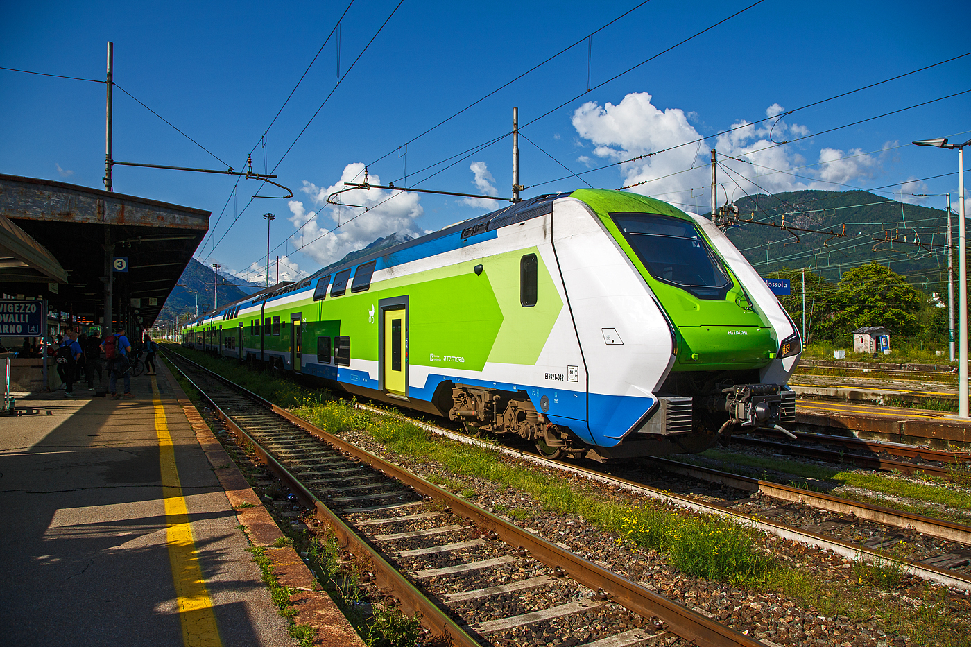 Der Trenord „Caravaggio“ ETR 421-042 (94 83 4441 842-5 I-TN / 94 83 4441 042-0 I-TN) ein vierteilige Hitachi Caravaggio am 25 Mai 2023 im Bahnhof Domodossola. 

Diese Doppelstock-Elektrotriebzüge vom Typ Hitachi Caravaggio heißen bekanntlich bei der Trenitalia „Rock“, aber bei der Trenord heißen sie (wie bei Hitachi) „Caravaggio“. Die Züge sind aber sehr ähnlich dem „Rock“ von Trenitalia, der Unterschied liegt wohl in der Innengestaltung. Einige der Züge für Trenord wurden aber aus der Produktionslinie für die Trenitalia entnommen und weisen daher die gleiche Inneneinrichtung auf, während die übrigen das Trenord-Interieur erhalten haben.

Die Trenord hat z.Z. 105 dieser Doppelstock-Elektrozüge vom Typ Hitachi „Caravaggio“, als Baureihe ETR 421, ETR 521 oder ETR 521 S1 (ETR steht für italienisch Elettro Treno Rapido). Der Unterschied zwischen den beiden fünfteiligen ETR 521 und ETR 521 S1 (ursprünglich als ETR 522 vorgesehen) ist mir noch unbekannt.

Caravaggio für die FNM
Die Ferrovie Nord Milano unterzeichnete im September 2018 einen Rahmenvertrag über maximal 120 Züge mit vier oder fünf Wagen. Ein erster Abruf von 2018 umfasst 30 Vierteiler. Diese Fahrzeuge sind bei der Trenord für den Einsatz auf der S-Bahn Mailand vorgesehen. Weitere 10 Fünfteiler wurden für den Malpensa Express zum Mailänder Flughafen und 16 Vierteiler für eine Flughafenverbindung in Bergamo bestellt. Ein dritter Auftrag beinhaltet zusätzliche 10 Vierteiler und 40 Fünfteiler, die ab 2022 ausgeliefert wurden. Insgesamt werden folglich 56 Vierteiler und 50 Fünfteiler ausgeliefert. 

Der Hitachi Caravaggio ist ein elektrischer Doppelstock-Triebzug, der von Hitachi Rail Italia in Reggio di Calabria und Neapel gefertigt wird. Die italienische Trenitalia setzt diesen Typ unter dem Namen „Rock“ im Regionalzugverkehr ein. Ein Folgeauftrag, vier- und fünfteiligen Zügen, wurde von den Ferrovie Nord Milano (Trenord) für den Nahverkehr rund um Mailand bestellt, hier haben sie den Namen „Caravaggio“

Die Züge sind als ETR.421, ETR.521 und ETR.621 im italienischen Baureihenverzeichnis eingereiht, wobei die erste Ziffer die Anzahl der Wagen kennzeichnet. Hitachi nennt die Grundkonstruktion Masaccio. Auf der gleichen Plattform bauen die Blues-Dieseltriebzüge der Trenitalia auf. Diese sind einstöckig und mit Akkus ausrüstbar. Namensgeber für die Zugtypen sind die italienischen Künstler Masaccio und Caravaggio, die im 15. und 16. Jahrhundert herausragende Gemälde schufen.

Der Hersteller Hitachi Rail Italy S.p.A. ist kein unbekannter auf Italiens Schienen, denn Hitachi war bis 2015 noch AnsaldoBreda und war auch an der Entwicklung und Bau der Hochgeschwindigkeitszügen ETR 400 (Frecciarossa 1000) beteiligt. Im Jahr 2015 übernahm der japanische Konzern Hitachi die AnsaldoBreda. Hitachi Rail Italien baut im Werk Pistoia (nördlich von Florenz) die doppelstöckigen Elektrotriebzüge (EMU) vom Typ „Caravaggio“. In Neapel werden die Drehgestelle und Komponenten gebaut.

Bauart / Aufbau
Die Züge bestehen aus vier bis sechs Doppelstockwagen. Jeder Wagen besitzt zwei einflügelige Türen im Unterstock pro Wagenseite. Ein Wagenteil ruht jeweils auf 2 luftgefederten Drehgestellen, die Frontwagen besitzen jeweils 2 Triebdrehgestelle mit je zwei TSA-Gleichstrommotoren, so ergibt sich ein Gesamt-Stundenleistung von 3.400 kW. Die sechsteiligen EMU haben zudem in der Mitte noch ein weiteres Wagenteil mit 2 Triebdrehgestellen, so haben die ETR 621 die Achsfolge Bo′Bo′+2′2′+2′2′+Bo′Bo′+2′2′+Bo′Bo′ und eine Gesamt-Stundenleistung von 4.200 kW (vermutlich gedrosselte Leistung). Die Züge sollen 30 % weniger Energie pro Passagierkilometer verbrauchen und mehr Passagiere pro Wagenlänge befördern können als frühere Modelle.

Jeder Zug wird von einem 3-kV-Gleichstromsystem angetrieben, dass 3.400 kW (4.600 PS) erzeugt und eine Höchstgeschwindigkeit von 160 km/h (99 mph) erreicht. Die Antriebsausrüstung ist größtenteils auf dem Dach montiert, wodurch der Innenraum optimal für die Unterbringung der Passagiere genutzt werden kann. Die Beschleunigung des Zuges beträgt 1,1 m/s², was zu einer verbesserten Pünktlichkeit beiträgt. Der Zug ist mit seitlichen und nach vorne gerichteten Kameras mit Anomalie-Erkennung ausgestattet. Der Wagenkasten besteht hauptsächlich aus Leichtmetalllegierungen, was ein geringes Gewicht pro Passagier und eine hohe Passagierkapazität pro Längeneinheit ermöglicht. Die Passagierkapazität variiert je nach Betreiber.

Ein Zug ist zu einem einzigen durchgängigen barrierefreien Raum, ohne Türen oder Trennwände, angeordnet. Der neue Zug besitzt sehr große Fenster. Die Züge verfügen über Klimaanlagen, die sich an die Anzahl der Fahrgäste an Bord anpasst, um den Energieverbrauch zu senken. Jeder fünfteilige hat zehn Türen/Seite (vierteilige 8) und zwei Toiletten (eine Standardtoilette und eine für Personen mit eingeschränkter Mobilität). Zwei Bereiche in der Nähe der barrierefreien Toiletten sind für Rollstühle reserviert und verfügen über Andockmöglichkeiten und Serviceruftasten. Der Caravaggio verfügt über Gepäckablagebereiche und spezielle Stellplätze für Fahrräder und Kinderwaagen, sowie Steckdosen zum Aufladen von Elektrofahrrädern. Die Züge sind mit LED-Beleuchtung, WLAN, USB-Anschlüssen, einem Fahrgastinformationssystem, Energiezählern und einem Fahrgastzähler ausgestattet. Treppen über den Drehgestellen ermöglichen den Zugang zum Oberdeck. Die Türen sind mit Schiebetritten ausgestattet, um den Spalt zwischen Bahnsteig und Fahrzeug zu überbrücken, wenn der Zug steht. Für Fahrgäste mit eingeschränkter Mobilität steht zudem eine manuell bedienbare Rampe zur Verfügung.

TECHNISCHE DATEN der ETR 421 (4-Teiler):
Typ: Hitachi Caravaggio
BR / Bezeichnungen: ETR 421, bei TN „Caravaggio“ und bei Trenitalia „Rock“
Baujahre: ab 2017
Spurweite: 	1.435 mm (Normalspur)
Fahrzeugbegrenzungslinie: GB
Achsfolge: Bo'Bo '+ 2'2' + 2'2 '+ Bo'Bo' 
Länge über Puffer: 109.600 mm 
Breite: 2.800 mm
Höhe über SO (ohne Stromabnehmer): 4.300 mm
Drehzapfenabstände (je Wagen): 19.100 mm
Achsabstand im Drehgestell: 2.650 mm
Treib- und Laufraddurchmesser: 920 mm (neu)
Höchstgeschwindigkeit: 160 km/h
Eigengewicht: ca. 204,0 t
Max. Achslast: 18,5 t
Beschleunigung:  1,10 m/s²
Anzahl der Motoren: 8 luftgekühlte TSA-Gleichstrommotore
Traktionsmotoren: Typ TME 59A-22-4 von TSA - Traktionssysteme Austria GmbH (Wiener Neudorf)
Stundenleistung: 3.400 kW (4.622 PS)
Stromsystem: 3.000 V DC (=)
Sitzplätze: ca. 479 
Toiletten: 2 geschlossenes System, davon 1 Rollstuhlgerecht
Türen je Längsseite: 8
Kupplung: Scharfenbergkupplung (SCHAKU) Typ 10
Bremse: KB R-E-A (D)

Abweichende TECHNISCHE DATEN der ETR 521 (5-Teiler):
BR / Bezeichnungen: ETR 521, bei TN „Caravaggio“ und bei Trenitalia „Rock“
Achsfolge: Bo'Bo '+ 2'2' + 2'2 '+ 2'2 '+ Bo'Bo' 
Länge über Puffer: 136.800 mm
Sitzplätze: ca. 600
Türen je Längsseite: 10

Abweichende TECHNISCHE DATEN der ETR 621 (6-Teiler):
BR / Bezeichnungen: ETR 621, bei Trenitalia „Rock“
Achsfolge: Bo'Bo '+ 2'2' + 2'2 '+ Bo'Bo' + 2'2 '+ Bo'Bo' 
Länge über Puffer: 163.400 mm
Anzahl der Motoren: 12 luftgekühlte TSA-Gleichstrommotore
Stundenleistung: 4.200 kW (5.710 PS), gedrosselt
Sitzplätze: ca. 720
Türen je Längsseite: 12

Quellen: Trenord, Trenitalia, Hitachi, TSA, Anschriften an den ETR, Wikipedia (D und I) 
Stand: September 2025
