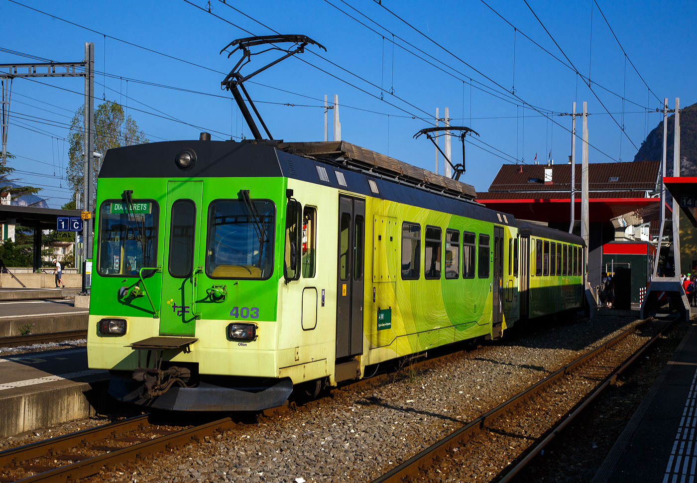Der Triebwagen tpc ASD BDe 4/4 403 „Ollon” mit dem Steuerwagen tpc ASD Bt 431 haben am 10 September 2023, als ASD (Aigle–Sépey–Diablerets) Regionalzug R 24 von Les Diablerets via Le Sépey, nun den Bahnhof Aigle erreicht. Die 23,3 Kilometer lange Strecke der ASD (Aigle–Sépey–Diablerets) ist eine reine Adhäsionsbahn und führt von Aigle über Le Sépey nach Les Diablerets.

Der elektrische Personen-Triebwagen mit Gepäckabteil wurde 1987 von Vevey ACMV (Ateliers de constructions mécaniques de Vevey) in Vevey gebaut, die elektrische Ausrüstung ist von der BBC (Brown, Boveri & Cie.). Er ist ein sogenannter ACMV Westschweizer Meterspurtriebwagen der zweiten Generation. 

Die Westschweizer Meterspurtriebwagen sind elektrische Triebwagen, die 1985 bis 1992 von den Ateliers de constructions mécaniques de Vevey ACMV und 1996 von Vevey Technologies an sechs Westschweizer Privatbahnen für verschiedene Stromsysteme und zum Teil mit gemischtem Adhäsions- und Zahnradantrieb geliefert wurden. Die Fahrzeugfamilie ist modular aufgebaut und ließ sich bezüglich ihrer Größe und Ausstattung an die Erfordernisse der jeweiligen Bahngesellschaft anpassen. Die Triebwagen wurden elf Jahre produziert und während dieser Zeit der technischen Entwicklung angepasst.

Die Fahrzeuge sind in leichter Stahlbauart konstruiert und 2,65 Meter breit. Die Schürzen, der Unterteil des Kastens, wurden aus Aluminium-Stangpressprofilen hergestellt, die nach einer Kollision mit Kraftfahrzeugen ausgewechselt werden können. An den Stirnwänden wurden bei weniger beanspruchten Elementen Formteile aus glasfaserverstärktem Kunststoff verwendet. Die Wagenkästen der Triebwagen sind für die Aufnahme der elektrischen Ausrüstung verstärkt und mit Befestigungspunkten versehen. Für die Laufdrehgestelle wurde eine Bauart übernommen, die schon bei Steuerwagen der Chemin de fer Bière–Apples–Morges und Chemin de fer Yverdon–Ste-Croix verwendet wurde. Die Triebdrehgestelle verfügen über einen Rolldrehkranz und zwei längs angeordnete Fahrmotoren, die je eine Achse über Kardanwellen antreiben.

Neben einer Rekuperations- und einer Widerstandsbremse sind die Triebwagen mit einer selbsttätigen Druckluftbremse ausgerüstet. Weil deren Hauptleitung durch die Elektronik gesteuert wird, kann der Zug einhändig mit dem Fahrschalter bedient werden.

Die Aigle–Sépey–Diablerets-Bahn (ASD), seit 1999 Teil der Transports Publics du Chablais (TPC), konnten 1987 neues Rollmaterial beschaffen, so auch vier dieser Triebwagen BDe 4/4 (401 bis 404). Wegen ihrer engen Kurven dienten die kurzen NStCM-Triebwagen als Basisfahrzeug. Als Steuerwagen dienen der ASD Fahrzeuge der ehemaligen Birsigthalbahn, die sie von der Baselland Transport (BLT) erworben werden konnte. Für den Einsatz auf der ASD wurde der Führerstand, bei den ex BTB-Steuerwagen neu aufgebaut.

Auch die AOMC (Aigle-Ollon-Monthey-Champéry-Bahn) hat drei solcher Triebwagen (BDeh 4/4 501 bis 503) beschafft, diese waren aber durch den Zahnradbetrieb und das andere Stromsystem der AOMC doch anders ausgeführt, u.a. auch in besonderer Leichtbauweise. Um die technischen Normalien ihrer Strecken zu vereinheitlichen, bauten die TPC im Jahr 2016 die Linie von Aigle nach Champéry um. Sie ersetzten das bisherige Zahnstangensystem Strub durch eine Abt-Zahnstange und erhöhten die Fahrleitungsspannung auf 1500 Volt. Damit verloren diese BDeh 4/4 501–503 und die zugehörigen Steuerwagen ihr Einsatzgebiet.

TECHNISCHE DATEN:
Baujahr: 1987 (4 Stück)
Spurweite: 1.000 mm
Achsformel: Bo’Bo’
Wagenkastenmaterial: Stahl
Länge über Puffer:18.800 mm
Breite: 2.650 mm
Gewicht: 32,4 t
Höchstgeschwindigkeit: 65 km/h (ursprünglich 25 km/h)
Leistung: 820 kW
Stromsystem: 1500 Volt DC (Gleichstrom)
Elektrische Ausrüstung: Schützensteuerung
Sitzplätze: 32
Kupplungstyp: BSi -Kompaktkupplung 

Die BSI-Kompaktkupplung ist eine mechanische Vorrichtung zum Verbinden zweier Schienenfahrzeuge zu einem Zug. Sie überträgt die Zug- und Druckkräfte innerhalb eines Zugverbandes und lässt sich automatisch kuppeln und entkuppeln. Sie findet überwiegend bei Straßenbahnwagen und Regionaltriebwagen der Eisenbahn Verwendung. Die Kupplung wurde vom ehemaligen Unternehmen Bergische Stahl-Industrie-Gesellschaft in Remscheid entwickelt, inzwischen Teil der Wabtec-Gruppe.


Der Steuerwagen tpc ASD Bt 431,  ex BTB/BLT (Bt 26):
Die Geschichte:
Anlässlich der Modernisierung des BTB-Rollmaterials und für die Bildung von die Betriebsabwicklung stark vereinfachenden Pendelzügen wurden 1966 auch sieben Steuerwagen Bt 21 bis 27 beschafft. Diese standen jedoch lediglich sechs neuen Triebwagen ABe 4/4 11 bis 16 gegenüber. Der zusätzliche Steuerwagen wurde ab 1977 für einen Pendelzug mit den entsprechend angepassten Be 4/4 der Serie 8 bis 9 aus dem Jahre 1951 benötigt.

Die Steuerwagen entsprachen bezüglich des wagenbaulichen Teils so weit als möglich den Motorwagen. Es waren zwei Fahrgastabteile (Raucher/Nichtraucher) vorhanden. Auf der führerstandslosen Seite befanden sich die Plattformen mit den beidseitigen, pneumatisch betätigten Falttüren ganz am Wagenende, um im Wageninnern möglichst viele Sitzplätze anordnen zu können. Als Drehgestelle kamen solche elastischer Bauart mit Flexicoil-Lagerung und Gummi-Zusatzfedern sowie Klotzbremse zum Einbau.

Der Führerstand entsprach jenem der Motorwagen (ABe 4/4). Er war von Anfang an so ausgelegt, dass auch die entsprechend angepassten Be 4/4 8 und 9 ferngesteuert werden konnten. Eine Stirnwandtüre ermöglichte das Mitführen von Zusatzwagen oder das Einreihen eines Steuerwagens in der Zugsmitte. 1972 wurde der Zugfunk nachgerüstet.

Mit der Fusion der Basler Vorortsbahnen 1974 gingen alle sieben Steuerwagen, welche immer Seite Rodersdorf an die Züge gestellt wurden, an die neugegründete Baselland Transport AG (BLT) über ,so wurde dieser zum BLT Bt 26.

Nach der Betriebsumstellung im Herbst 1984 verkaufte die BLT alle sieben Fahrzeuge in die Westschweiz. Die Bt 22, 23, 24 und 25 kamen als Bt 132, 133, 134 und 131 zur Schmalspurbahn Aigle–Ollon–Monthey–Champéry (AOMC).

Die Bt 21 sowie 26 und 27 fanden den Weg zur Aigle–Sépey–Diablerets-Bahn (ASD). Ab September 1985 wurden sie bei ACMV in Vevey für den Betrieb mit den für 1987 bestellten Triebwagen BDe 4/4 401 bis 404 hergerichtet. Die Anpassungen umfassten im Wesentlichen:
• Neuanstrich
• Verschließen der vorderen Stirnwandtüren
• Einbau eines neuen Führertisches
• Anpassungen an den Steuerstromkreisen
• Anpassungen der elektrischen, pneumatischen und mechanischen Kupplungen (BSi)
• Einbau von Schienenbremsmagneten in beide Drehgestelle

Die Inbetriebsetzung erfolgte ab Juni 1987 als Bt 431 bis 433.

TECHNISCCHE DATEN bei Inbetriebsetzung (1966):
Spurweite: 1.000 mm
Typenbezeichnung: Bt
Anzahl Wagen: 7
Länge über alles: 17.212 mm
Größte Breite: 2.500 mm
Höhe über Dach: 3.450 mm
Drehzapfenabstand: 11.000 mm
Achsabstand im Drehgestell: 1.800 mm
Eigengewicht: 17.000 kg
Sitz-/Stehplätze: 64 / 66 (zusätzlich 2 Klappsitze)
Höchstgeschwindigkeit: 65 km/h
Anschaffungskosten/Wg.: CHF 356.205,–

Abweichende heutige Daten:
Eigengewicht: 18 t 
Sitz-/Stehplätze: 56/ 60 
Max. Ladegewicht: 2,5 t (so müsste er eigentlich BDt 431 heißen)

Als vierter Steuerwagen stieß 2000 der jahrelang abgestellte und nie in Betrieb genommene Bt 131 der AOMC (ex BTB/BLT Bt 25) hinzu. Dieses Fahrzeug erfuhr dieselben Anpassungen wie die Bt 431 bis 433,  wobei jedoch in Abweichung dazu die Stirnwandtüre belassen wurde.