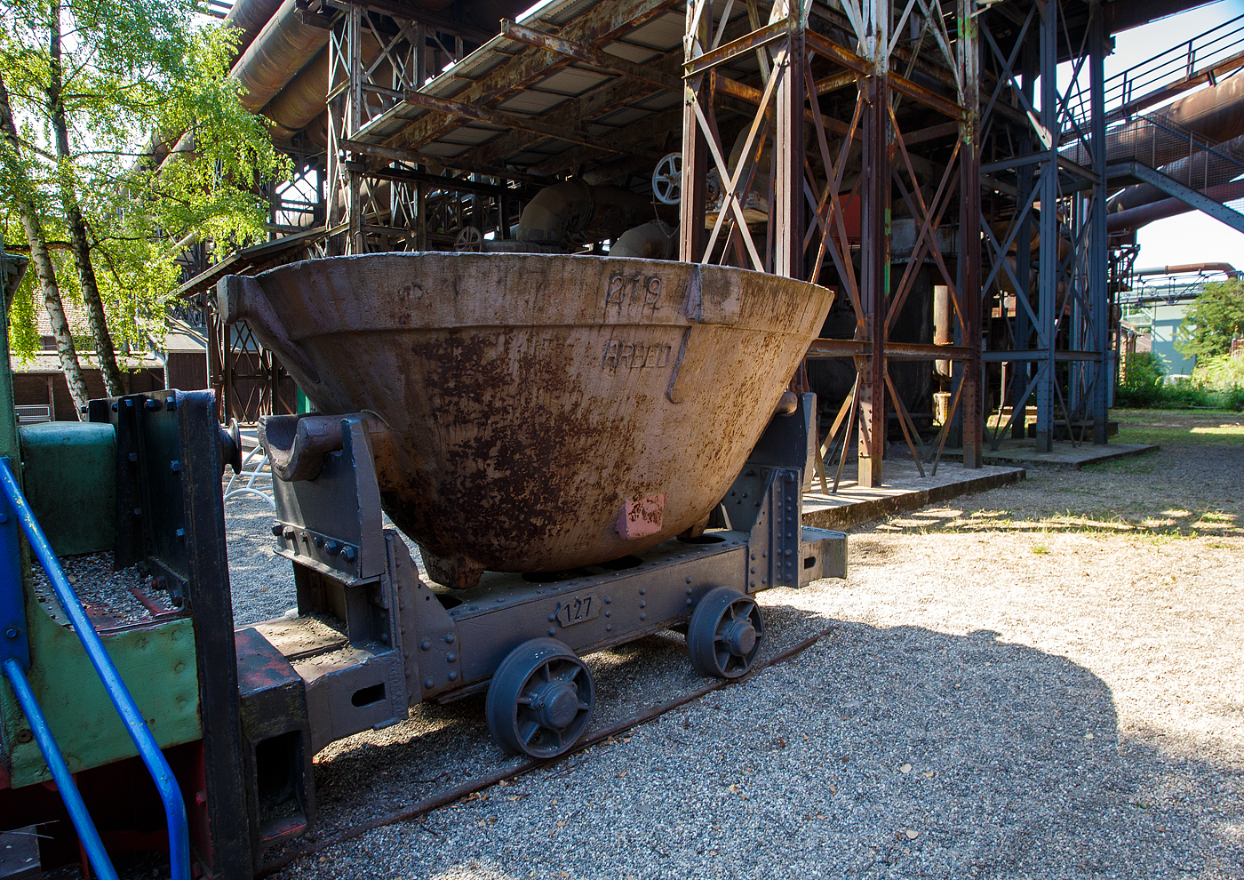 Der zweiachsige 785 mm Schmalspur Schlackewagen 127 mit dem K�bel ARBED 219, hinter Dampflokomotive Nr. 20 der V�lklinger H�tte (ehem. R�chling'schen Eisen- und Stahlwerke GmbH in V�lklingen/Saar, ab 1982 ARBED-Saarstahl GmbH, ab 1986 Saarstahl V�lklingen GmbH) hier am 01 Juli 2025 als Denkmal beim Biergarten V�lklinger H�tte. Heutiger Eigent�mer ist die Initiative V�lklinger H�tte e.V..