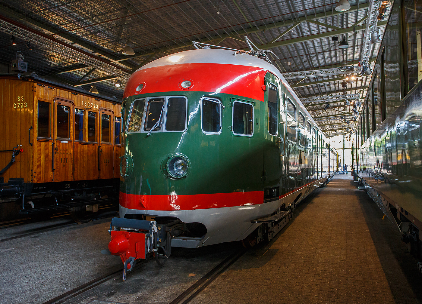Der zweiteilige Elektrotriebwagenzug Mat '36 – NS 252, am 29 April 2025 im Het Spoorwegmuseum (bis 2005 NSM - Nederlands Spoorwegmuseum / Niederländischen Eisenbahnmuseum) in Utrecht im Bahnhof Maliebaanstation. Ein sehr schönes Eisenbahnmuseum das zum Verweilen einlädt, leider fehlte uns dieses Mal die Zeit dafür. 

Der ET Mat '36 – NS 252 wurde 1938 von Werkspoor N.V. in Utrecht gebaut für die NS - Nederlandse Spoorwegen (Niederländischen Staatsbahnen) gebaut. Die elektrische Ausrüstung war von Heemaf. Während des Zweiten Weltkrieges wurde er um einen Mittelwagen erweitert. Der Triebzug 252 (ehemals Zug 418) wurde 1970von STIBANS vor dem Abriss gerettet, auf den ursprünglichen zweiteiligen Zug gekürzt, wieder mit der Nummer 252 neu nummeriert und konserviert. Im Jahr 2009 wurde er dem Eisenbahnmuseum übergeben. 

Die NS-Baureihe Mat ’36 oder Materieel ’36 war eine Serie von 90 Elektrotriebzügen, die von der NS - Niederländischen Staatsbahnen ab 1936 eingesetzt wurde. Das technische Konzept der Triebzüge beruht auf der zwei Jahre zuvor beschafften Baureihe Mat ’34 mit dieselelektrischem Antrieb. Merkmale waren Stromlinienform, Faltenbälge an den Wagenübergängen, Schürzenbleche an den Unterseiten und eine glatte Schweißkonstruktion der Wagenkästen. Trotz Stromabnehmern nannte die Öffentlichkeit sie weiterhin „Diesels“.

Das Design des Mat '36 aus den späten 1930er Jahren ist etwas Besonderes. Vor dieser Zeit war es üblich, mit Dampflokomotiven und Einzelwaggons zu fahren. Schon früh setzte man in den Niederlade auf die Elektrifizierung. Die Hauptstrecken zwischen den größeren Städten der Niederlande waren zu der Zeit bereits weitgehend elektrifiziert. Auf diesen Verbindungen wurden die Triebzüge der Baureihe Mat ’36 eingesetzt. Das Design des Zuges baut auf der ersten Stromlinienbauart Mat ’34 (DE3 - „Dieseldrie“) auf und war technologisch und konstruktiv fortschrittlich.

Beschreibung und Einsatz:
Der Lieferung vorausgegangen war eine Prototypenserie von acht Zügen mit der Bezeichnung Mat ’35, Seriennummer NS 201 – 208. Die Baureihenbezifferung bei den Triebzügen der NS bezieht sich stets auf das erste Jahr der Indienststellung. Die Vorserie wurde auf der Verbindung von Rotterdam nach Hoek van Holland eingesetzt, daraus ergab sich der Spitzname die „Hoek van Hollanders“. Die Hauptserie wurde nur leicht verändert, es gab Schiebetüren anstelle von Schwingtüren und der Gepäckraum wurde verkleinert.

Die Mat ’36-Serie bestand zunächst aus 53 zweigliedrigen Zügen (Typ EI2) mit den Nummern 211 – 263 und 37 dreigliedrigen Zügen (Typ EID3) mit den Nummern 601 – 637. Die zweiteiligen Garnituren hatten Jakobs-Drehgestelle in der Mitte, die dreiteiligen Garnituren hatten eine klassische Abstützung mit zwei separaten Drehgestellen für jeden Wagenkasten. Ab 1942 wurden 29 zweiteilige und alle dreiteiligen Züge um einen mittleren Wagenkasten verlängert. Die neuen Dreiteiler erhielten die Nummerierung 401 – 429, während die neuen Vierteiler ihre Nummerierung behielten. Nach 1952 wurden weitere 13 Triebzüge zu dreigliedrigen Zügen umgebaut, sie erhielten die Nummern 441 – 453.

Die Hauptstrecken zwischen den größeren Städten der Niederlande waren zu der Zeit bereits weitgehend elektrifiziert. Auf diesen Verbindungen wurden die Triebzüge der Baureihe Mat ’36 eingesetzt.

1940 erfolgte eine weitere Lieferung der Baureihe mit der Bezeichnung Mat ’40. Sie bestand aus 15 zweigliedrigen und 25 fünfgliedrigen Zügen. Im Vergleich zur Vorgängerserie wurde die Größe der Frontfenster leicht verändert, und die Züge erhielten auch eine 1. Klasse. Während des Zweiten Weltkriegs gingen mehrere Züge verloren. Danach war der Bedarf an Transportkapazitäten hoch, soweit wie möglich wurden beschädigte Züge wieder instandgesetzt und es wurde eine weitere Serie von 144 Zügen mit der Bezeichnung Mat ’46 bestellt. Davon waren 79 Züge zweigliedrig und 65 viergliedrig. Auch diese Züge unterschieden sich nur geringfügig von den Vorkriegsausführungen. In der Summe ergeben sich 282 weitgehend ähnliche Triebzüge mit elektrischem Antrieb, die auf der Konstruktion der Baureihe Mat ’36 beruhen.

Die Mat-36-Serie mit 217 Wagen war die größte Bestellung von Schienenfahrzeugen, die die NS jemals aufgegeben hat.

Technik der zweiteiligen ET (El2):
Die zweiteiligen Zuggarnituren sind 43.48 Meter lang und wogen bei der Anlieferung 79 Tonnen. Der Triebzug ist mit 4 Elektromotoren des Herstellers Heemaf vom Typ TM-712 ausgestattet. Jeder Motor leistet 165,5 kW (225 PS) bei bis zu 1.690 U/min.. Insgesamt verfügt ein Triebzug über eine Leistung von 662 kW (900 PS). Die Aufhängung dieser Motoren entspricht der Aufhängung einer Straßenbahn. Der Fahrmotor ist einseitig gleitgelagert auf der Achse gelagert. Der Antrieb der Motorwelle erfolgt über ein Ritzel, dass das Zahnrad auf der Radsatzwelle antreibt. Der Zug ist für eine Geschwindigkeit von 125 km/h. Im normalen Zugbetrieb wurde eine Geschwindigkeit von 110 km/h gefahren. Der ET verfügt über 24 Sitzplätze in der zweiten Klasse und 96 Sitzplätze in der dritten Klasse. 

Die Pressluft für die Druckluftbremse und verschiedene elektropneumatische Geräte wird von zwei Kompressoren, sind unter dem Ck-Wagen (3. Klasse Wagen) befinden, erzeugt. Sie liefern bis zu 280 Liter Luft pro Minute. Zur Stromversorgung des Steuerstroms und der Beleuchtung ist unter dem Wagen ein Motorgenerator von Heemaf vom Typ GM32/30, installiert. Dieser wandelt die 1.500 Volt Oberleitungsspannung in 100 Volt Spannung für den Steuerstrom und 145 Volt für die Beleuchtung um. Der Motorgenerator liefert eine Leistung von 5 kW. Unter dem BCk-Wagen befinden sich die Schaltschränke und Relaiskästen. Auch die Anfahrwiderstände, Fahrschalter und die Folgerolle finden unter dem BCk-Wagen ihren Platz. Beide Wagen sind mit einem Scherenstromabnehmer ausgestattet. Um zu verhindern, dass zu viel Strom durch den Zug fließt, wurde auf dem Dach eine 1.000-Ampere-Sicherung angebracht.

Die zweiteiligen Züge, die 1941 und 1942 zu dreiteiligen Zügen erweitert wurden, haben eine Länge von 62,2 Metern und wiegen 105 Tonnen. Die Gesamtzahl der Sitzplätze erhöht sich in der dritten Klasse um 32, so dass insgesamt 24 Passagiere der zweiten Klasse und 128 Passagiere der dritten Klasse Platz finden. Die seit 1949 verlängerten dreizehn Züge haben eine Länge von 62,1 Metern und ein Gewicht von 106 Tonnen. Die Gesamtzahl der Sitzplätze erhöht sich in der dritten Klasse um 56, so dass insgesamt 24 Passagiere der zweiten Klasse und 152 Passagiere der dritten Klasse Platz finden.

Technik der dreiteiligen ET (ElD3):
Die dreiteiligen Zuggarnituren sind 72,2 Meter lang und wogen bei der Anlieferung 143 Tonnen. Auch der Triebzug ist mit Elektromotoren des Herstellers Heemaf vom Typ TM-712 ausgestattet, nur sind es hier 8 Stück. So habe diese die doppelte Traktionsleistung von 1.324 kW (1.800 PS), gegenüber den zweiteiligen, Antriebsart und Höchstgeschwindigkeit entsprechen der El2 (s.o.). Diese dreiteiligen ET verfügen über 48 Sitzplätze der zweiten Klasse und 144 Sitzplätze der dritten Klasse.

Nach der Verlängerung der dreiteiligen Züge betrug die Länge der vierteiligen Züge 95,6 Meter und ihr Gewicht betrug 181 Tonnen. Die Gesamtzahl der Sitzplätze erhöht sich in der dritten Klasse um 80, so dass insgesamt 48 Passagiere der zweiten Klasse und 224 Passagiere der dritten Klasse Platz finden.

Um ein schnelles Kuppeln zu ermöglichen, sind die Züge mit automatischen Kupplungen von Scharfenberg ausgestattet. Dies führte dazu, dass die Züge nicht an Züge mit Schraubkupplung und Puffern gekoppelt werden konnten.

TECHNISCHE DATEN:
Gebaute Anzahl: 90, davon ursprünglich EI2 zweigliedrig 53 und (EID3 dreigliedrig 37)
Hersteller:Werkspoor, Beijnes, Allan
Baujahre: ab 1936
Ausmusterung: bis 1970
Spurweite: 1.435 mm (Normalspur)
Achsfolge: Bo'(2')Bo' / (Bo' Bo'+2'2'+ Bo'Bo')
Länge über Kupplung: 43.48	0 mm / (72.200 mm)
Leergewicht: 79 t / (143 t)	
Höchstgeschwindigkeit: 125 km/h (Im Plandienst 110 km/h)
Kapazität: siehe Beschreibung oben
Motorentyp: 4 bzw. 8 Heemaf vom Typ TM-712 je 165,5 kW
Leistung: 662 kW / (1.324 kW)
Übersetzung: 21 : 61
Stromsystem: 1,5 kV Gleichstrom
