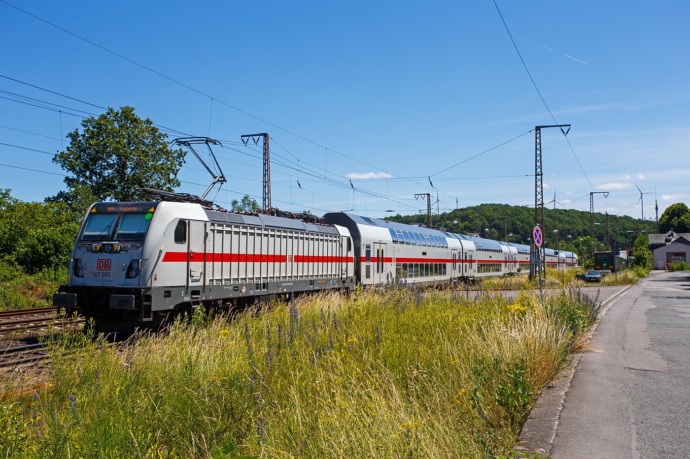 Die 147 580-5 (91 80 6147 580-5 D-DB - IC 4877) schiebt am 28 Juni 2024 die IC2-Garnitur 4877 der DB Fernverkehr AG Steuerwagen voraus, als IC 2229 / RE 34 - Umlauf RE 52229 (Dortmund Hbf – Siegen – Dillenburg - Frankfurt/Main Hbf), durch Wilnsdorf-Rudersdorf (Kreis Siegen) in Richtung Frankfurt/Main. Zwischen Dortmund Hbf und Dillenburg wird der Zug auch als RE 34 (hier Umlauf 52229) geführt und hat in diesem Abschnitt die Freigabe für alle Nahverkehr Tickets.

Die TRAXX P160 AC3 wurde 2020 von Bombardier in Kassel unter der Fabriknummer 35663 gebaut und an die DB Fernverkehr AG ausgeliefert. Sie hat die Zulassungen für Deutschland und die Schweiz, daher hat sie auch vier Stromabnehmer. Der Bahnstrom (15.000 V 16 ⅔ Hz) ist ja derselbe, aber die Palettenbreite (Wippe) ist 1.450 mm im SBB-Netz und somit 500 mm schmaler als die Wippen fürs DB Netz (1.900 mm breit). Das Schleifleistenmaterial ist bei beiden aus Graphit.