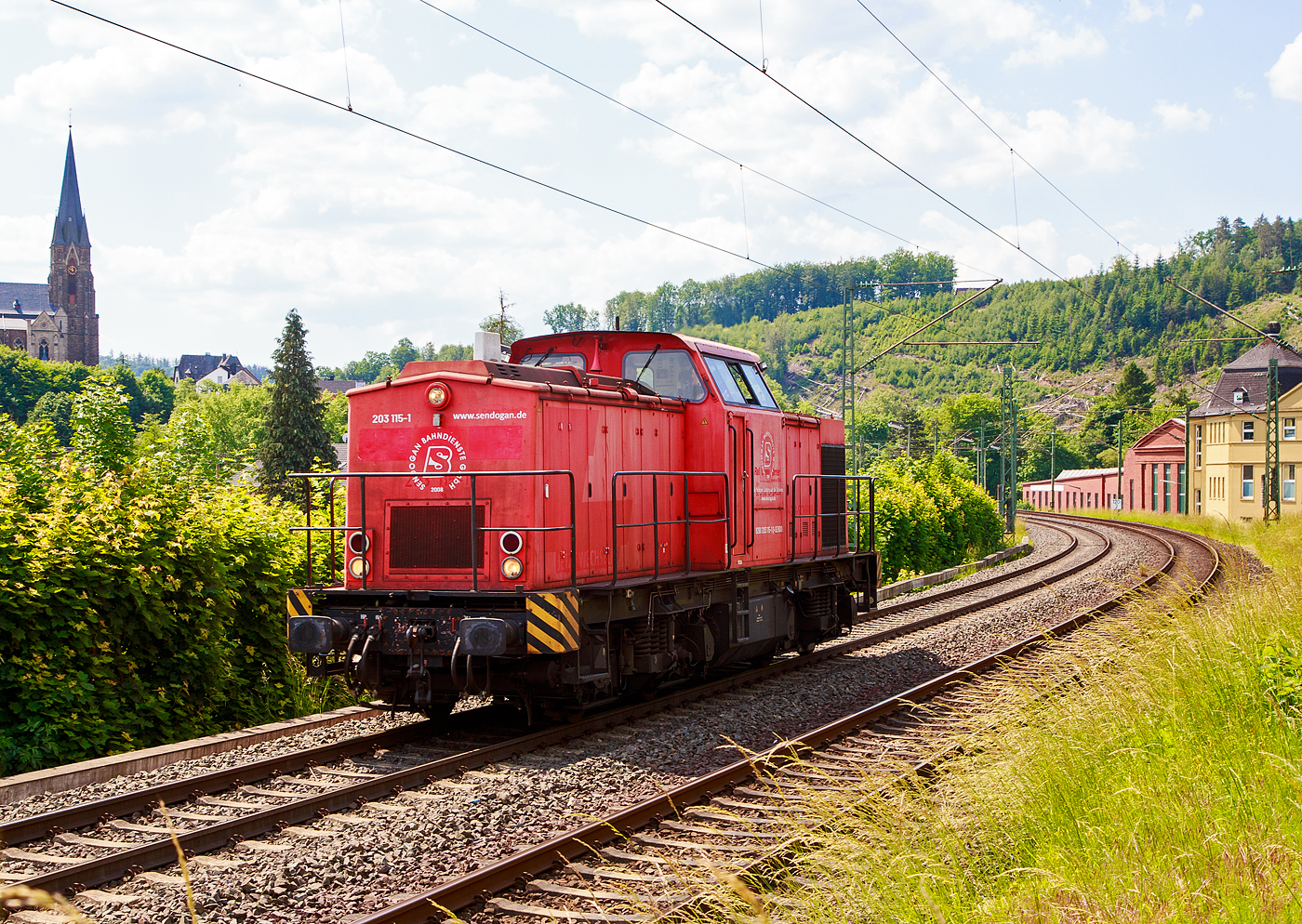 Die 203 115-1 (92 80 1203 115-1 D-SENDO) der Sendogan Bahndienste GmbH (Recklinghausen), ex DB 202 450-3, fährt am 06.06.2023 als Lz (Lokzug) bzw. auf Tfzf (Triebfahrzeugfahrt) Kirchen an der Sieg in Richtung Siegen. Übrigens recht in den Fabrikhallen wurde früher auch Loks gebaut, es ist die Lokfabrik Arnold Jung in Jungenthal bei Kirchen an der Sieg.

Die V 100.1 wurde 1972 bei LEW (VEB Lokomotivbau Elektrotechnische Werke „Hans Beimler“, Hennigsdorf) unter der Fabriknummer 13489 gebaut und als DR 110 450-4 an die DR ausgeliefert. 1984 erfolgte der Umbau in DR 112 450-2, die Umzeichnung in DR 202 450-3 erfolgte 1992, die Ausmusterung bei der DB erfolgte 1998. Im Jahre 2002 erfolgte durch ALSTOM Lokomotiven Service GmbH, Stendal der Umbau gemäß Umbaukonzept  BR 203.1  in die heutige 203 115-1, die Inbetriebnahme war im Jahr 2005. Von 2005 bis Dezember 2010 war die Lok von ALSTOM Lokomotiven Service GmbH wieder an die DB (DB Regio bzw. DB Schenker) vermietet, bis sie Anfang 2011 an die EBM verkauft wurde. 2015 wurde die EBM Cargo GmbH von der Rail Cargo Carrier - Germany GmbH (zur ÖBB) übernommen, somit wurde die Lok zur 92 80 1203 115-1 D-RCCDE. Im Mai 2021 ging sie an die Sendogan Bahndienste GmbH in Recklinghausen.

TECHNISCHE DATEN:
Spurweite: 1.435 mm (Normalspur)
Achsanordnung: B'B'
Länge über Puffer: 14.240mm
Radsatzabstand im Drehgestell: 2.300mm
Drehzapfenabstand: 7.000mm
Höhe über SO: 4.255mm
Dienstgewicht: 69 t

Motor: 12-Zylinder CATERPILLAR-Dieselmotor mit Direkteinspritzung, Abgasturbolader und Ladeluftkühlung, vom Typ CAT 3512 DI-TA
Motorleistung: 1.305 kW (1.774 PS)
Nenndrehzahl: 1.800 U/min
Hubraum: 51,8 Liter (Bohrung-Ø 170 x Hub 190 mm)
Motorgewicht: 6.537 kg

Getriebe: Voith Strömungsgetriebe GSR 30/5,7
Leistungsübertragung: dieselhydraulisch
Anfahrzugkraft: 207 kN
Höchstgeschwindigkeit: 100 km/h
Kleinste Dauerfahrgeschwindigkeit: 11,1 km/h
Kleinster befahrbarer Gleisbogenradius: 80m
