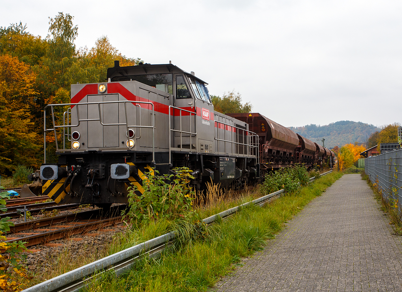 Die 277 809-0  Elmi“ (92 80 1277 809-0 D-KAF), eine Vossloh MaK G 1700 BB der KAF - Falkenhahn Bau AG (Kreuztal), steht am 12 Oktober 2025 mit einem Schotterzug im Bahnhof Herdorf. Mit dem Zug werden später die neuen Weichen 25 und 26 eingeschottert. 

Die Vossloh MaK G 1700 BB wurde 2001 von Vossloh in Kiel 2001 unter der Fabriknummer 1001113 gebaut und an die NE - Neusser Eisenbahn geliefert. Nach dem Zusammenschluss der HGK und der NE zur RheinCargo GmbH & Co. KG, fuhr sie noch als RHC 277 809-0. Anfang 2014 ging sie an die Vossloh Locomotives GmbH (92 80 1277 809-0 D-VL) und war 1 ½ Jahre als Mietlok unterwegs, bis sie im Juni 2015 an die Michael Bugdoll Bau- und Sicherungsarbeiten e. K in Dorsten ging, als diese konnte ich sie auch mal ablichten. Seit 01.01.2021 ist die Lok nun bei der KAF - Falkenhahn Bau AG (Kreuztal), hier hat sie aber ihren Namen  Elmi“ behalten. 

TECHNISCHE DATEN:
Baujahr: 2001 - 2003
gebaute Stückzahl: 6
Spurweite: 1.435 mm (Normalspur)
Achsfolge: B´B´
Länge über Puffer: 14.700 mm
Drehzapfenabstand: 7.400 mm
Achsabstand im Drehgestell: 2.400 mm
größte Breite: 3.080 mm
größte Höhe über Schienenoberkante: 4.220 mm
Raddurchmesser: 1.000 mm (neu)
kleinster befahrbarer Gleisbogen: 60 m
Dienstgewicht 87,3 t
Kraftstoffvorrat 3.500 l
Motor: MTU-12-Zylinder-Dieselmotor, vom Typ 12V 4000 R20
Leistung: 1.500 kW bei 1800 U/min
Getriebe: Voith L 5r4 zU2
Anfahrzugkraft: 249 kN
Höchstgeschwindigkeit: 100 km/h

Die Vossloh Lokomotive MaK G 1700 BB ist eine dieselhydraulische Lokomotive. Bei der Überarbeitung der Typenpalette nach der Übernahme der MaK durch Vossloh 1998 wurde im 4. Typenprogramm unter der Bezeichnung G 1700 BB der Bau einer vierachsigen Streckenlokomotive mit Mittelführerhaus vorgesehen. Tatsächlich handelte sich zunächst um eine Weiterentwicklung der G 1206. Die Maschine wurde in einigen Details an die Lokomotiven des 4. Typenprogramms angepasst. Dies betraf in erster Linie den Rahmen, der so geändert wurde, dass die neuen Standarddrehgestelle verwendet werden konnten. Dabei wurden die Rahmenenden so umgestaltet, dass die Lokomotiven die im 4. Typenprogramm üblichen Komfortaufstiege erhielten. Ebenfalls geändert wurde der Dieselmotor. Zum Einsatz kam der schon bei den G 1206 für die Dortmunder Eisenbahn verwendete MTU 12V 4000 R20 mit einer unveränderten Leistung von 1.500 kW bei 1.800 U/min. Die übrigen Komponenten der G 1700 BB blieben gegenüber der G 1206 weitgehend unverändert.

Der Dieselmotor ist ein wassergekühlter MTU 90°-V12-Zylinder-Viertakt-Dieselmotor mit Common-Rail-Einspritzung, OHV-Ventilsteuerung, Registeraufladung mit Ladeluftkühlung. Der Hubraum beträgt 57.199 cm³ (57,2 Liter), die Zylinder haben eine Bohrung von Ø 170 mm × 210 mm Hub. Die Motorabmessungen (LxBxH) sind 2.670 x 1.696 x 2.001 mm, das Gewicht (trocken) beträgt 7.700 kg.

Die ersten beiden Lokomotiven dieses Typs (die KSW Lok 42 und diese hier) wurden im Jahr 2001 ausgeliefert. Ende 2002 bis Anfang 2003 folgten weitere vier Lokomotiven aus Vorratsbauten. Nach diesen sechs Lokomotiven wurde der Bau der G 1700 BB zugunsten der technisch sehr ähnlichen und bereits weiter verbreiteten G 1206 wieder eingestellt.

So ist der Nachfolger die G 1700-2 BB keine Weiteentwicklung der G 1700 BB, sondern um eine komplette Neuentwicklung. 