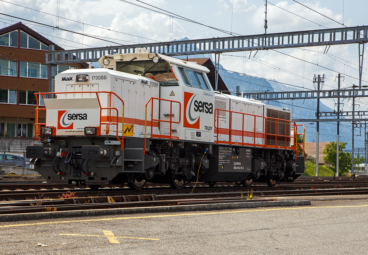 Die Am 843 151 „Trudy“ (98 85 5843 151-2 CH-SERSA) der Sersa (Rhomberg Sersa Rail Group), eine Schweizer Version der MaK G 1700-2 BB, ist am 28.05. 2023 beim Bahnhof Spiez abgestellt.

Die Am 843 wurde 2004 von Vossloh in Kiel (ehem. MaK) unter der Fabriknummer 5001492 gebaut und an die Sersa AG (CH) geliefert. Die angeschriebene Bezeichnung „MaK G 1700 BB“ ist eigentlich nicht ganz richtig, denn die Schweizer Version Am 843 unterscheidet sich etwas von der MaK G 1700 BB.

Die Schweizerischen Bundesbahnen (SBB) bestellten bei Vossloh zunächst 59 Lokomotiven der Baureihe Am 843. Diese Lokomotiven werden im schweren Rangier- und leichten Streckendienst eingesetzt. Dazu gehört neben dem Rangierdienst in den größeren Rangierbahnhöfen und auf Stationen auch der Zustelldienst mit Streckenfahrten im Nahbereich. Ein weiteres Einsatzgebiet für die Lokomotiven besteht im Bau- und Interventionsdienst.

Um die Am 843 für diese sehr unterschiedlichen Aufgaben möglichst gut anzupassen fiel die Wahl auf eine der G1206 sehr ähnliche Maschinenanlage. Das Turbowendegetriebe L 5r4 z wurde in einer Version als Stufengetriebe verwendet. Es besetzt einen Rangiergang mit 40 km/h Höchstgeschwindigkeit und hohen Zugkräften im unteren Geschwindigkeitsbereich, sowie einen Streckengang mit 100 km/h Höchstgeschwindigkeit. Der Motor bleib dagegen der gleiche und leistet unverändert .1500 kW.

Für die übrigen Komponenten bediente man sich bei der Entwicklung der Am 843 jedoch der wesentlich jüngeren G 1700-2 BB, die den hohen Komfortwünschen der SBB gerecht wurden und deutlich mehr Einbauräume für diversen Sonderausrüstungen, z. B. die schweizerischen Zugsicherungen Integra Signum und ZUB 262 ct bietet. Trotzdem unterscheidet sich die Am 843 durch das Linksführerhaus und die für die Schweiz typischen eckigen Lampen und Geländer mit Schutzblechen schon äußerlich deutlich von ihr. Eine weitere Besonderheit ist der Partikelfilter zur Reduzierung des Rußausstoßes, die erstmals bei einer Lokmotive dieser Leistungsklasse in Serie eingebaut wurde.

Im Herbst 2003 begann die Lieferung die ersten Loks. Weitere Lokomotiven der Baureihe Am 843 konnten an andere Bahnen in der Schweiz verkauft werden. Zunächst erhielt das Bauunternehmen Sersa AG im Sommer 2004 drei Lokomotiven, die bei der Ausrüstung des Lötschberg-Basistunnels eingesetzt wurden. Für den gleichen Tunnel, jedoch für den Bau- und Interventionsdienst im regulären Betrieb erhielt die BLS zwei Jahre später ebenfalls drei Am 843. Als Besonderheit erhielten die BLS-Loks die europäische Zugsicherung ETCS, die im neuen Tunnel verwendet wird.

Der Lokrahmen besteht aus Walzträgern und massiven Blechen, welche in Schweißkonstruktion miteinander verbunden wurden. Dadurch entsteht ein stabiler und robuster Grundaufbau, welcher der Lok die notwendigen Festigkeiten verleiht. Im Lokrahmen wurde eine so genannte Umweltwanne montiert, welche aus dem Fahrmotor austretenden Flüssigkeiten (Mineralölen und Wasseremulsionen) auffängt, diese können mit Hilfe eines Ablasshahnes entleert und fachmännisch entsorgt werden.

Der vordere längere Vorbau beinhaltet neben dem Dieselmotor auch die notwendige Kühlanlage und das Antriebsgetriebe. Der kürzere hintere Vorbau enthält neben der Druckluftanlage auch die elektrischen Komponenten wie die Batterieladung.

Zwischen den beiden Vorbauten befindet sich das Mittelführerhaus, welches über die zwei diagonal gegenüberliegenden Eingangstüren betreten werden kann. In ihm sind alle für den Lokführer notwendigen Einbauten vorhanden. Ein Führersitz je Fahrpult und Fahrrichtung, welcher mit Arm- und Rückenlehnen ausgerüstet ist, erlaubt die sitzende Bedienung der Lokomotive. Dieser Führersitz ist drehbar gelagert und kann zusammengeklappt und unter den Führertisch verschoben werden. Dadurch ist auch die stehende Bedienung der Lokomotive ohne Behinderung möglich. Zur Entlastung der Füße sind auch verstellbare Fußstützen montiert. Der Fußboden ist mit einem Profilgummibelag belegt worden, der eine einfache Reinigung und dennoch einen guten Stand erlaubt.

Angetrieben wird die Lokomotive von einem 12-Zylinder-4Takt-Dieselmotor vom Typ Caterpillar 3512 B DI-TA-SCAC, dieser erbringt mit Hilfe der beiden Abgasturbolader und der Ladeluftkühlung eine maximale Leistung von 1.500 KW (2.040 PS). Seine höchste Drehzahl beträgt 1.800 U/min. Er wird mit Hilfe eines elektrischen Anlassers gestartet und ist elektronisch geregelt. Dadurch ist es möglich, den Motor bestmöglich im optimalen Leistungsbereich zu betreiben. Sein Gewicht beträgt mit 322 Liter Schmieröl und 134 Liter Kühlwasser 7.700 kg.

Die vom Dieselmotor erzeugte Leistung wird mittels einer Gelenkwelle auf das hydrodynamische Getriebe (Turbowendegetriebe), vom Typ Voith L5r4zseU2, übertragen. Das Getriebe hat eine maximale Leistung von 1.400 kW. Es beschränkt somit die Leistung der Lokomotive und verhindert zugleich, dass der Fahrmotor überlastet werden kann. Seine maximale Drehzahl ist gleich groß, wie jene des Fahrmotors.

Das Turbowendegetriebe besitzt für jede Fahrrichtung zwei Drehmomentwandler. Dem eigentlichen Wandlergetriebe ist eine mechanische Getriebe nachgeschaltet, das eine niedrige für den Rangierbetrieb bestimmte Schaltung und eine höhere für den Streckenbetrieb bestimmte Schaltung zur Verfügung zu stellen. Diese Umschaltung darf jedoch erst im Stillstand erfolgen.

Die Achsen in den Drehgestellen werden über Gelenkwellen vom Turbowendegetriebe angetrieben. Die Übertragung auf die Achsen erfolgt mit Hilfe von Stirnradgetrieben mit Kegelradvorgelege.

Technische Daten:
Gebaute Anzahl: 79
Spurweite: 1.435 mm (Normalspur)
Achsformel: B'B'
Länge über Puffer: 15.200 mm
Höhe: 4.220 mm
Breite: 3.080 mm
Drehzapfenabstand: 7.700 mm
Achsstand im Drehgestell: 2.400 mm
Dienstgewicht: 80 t
Höchstgeschwindigkeit: 100 km/h (40 km im Rangiergang)
Installierte Leistung: 1.500 kW (2.040 PS)
Anfahrzugkraft: 249 kN
Treibraddurchmesser: 1.000 mm
Motorentyp: Caterpillar 3512B DI-TA-SCAC
Nenndrehzahl: 1.800/min
Getriebe:  Voith Typ L 5r4 zseU2 	
Kleinster bef. Halbmesser: 60 m
Tankinhalt: 3.500 l
