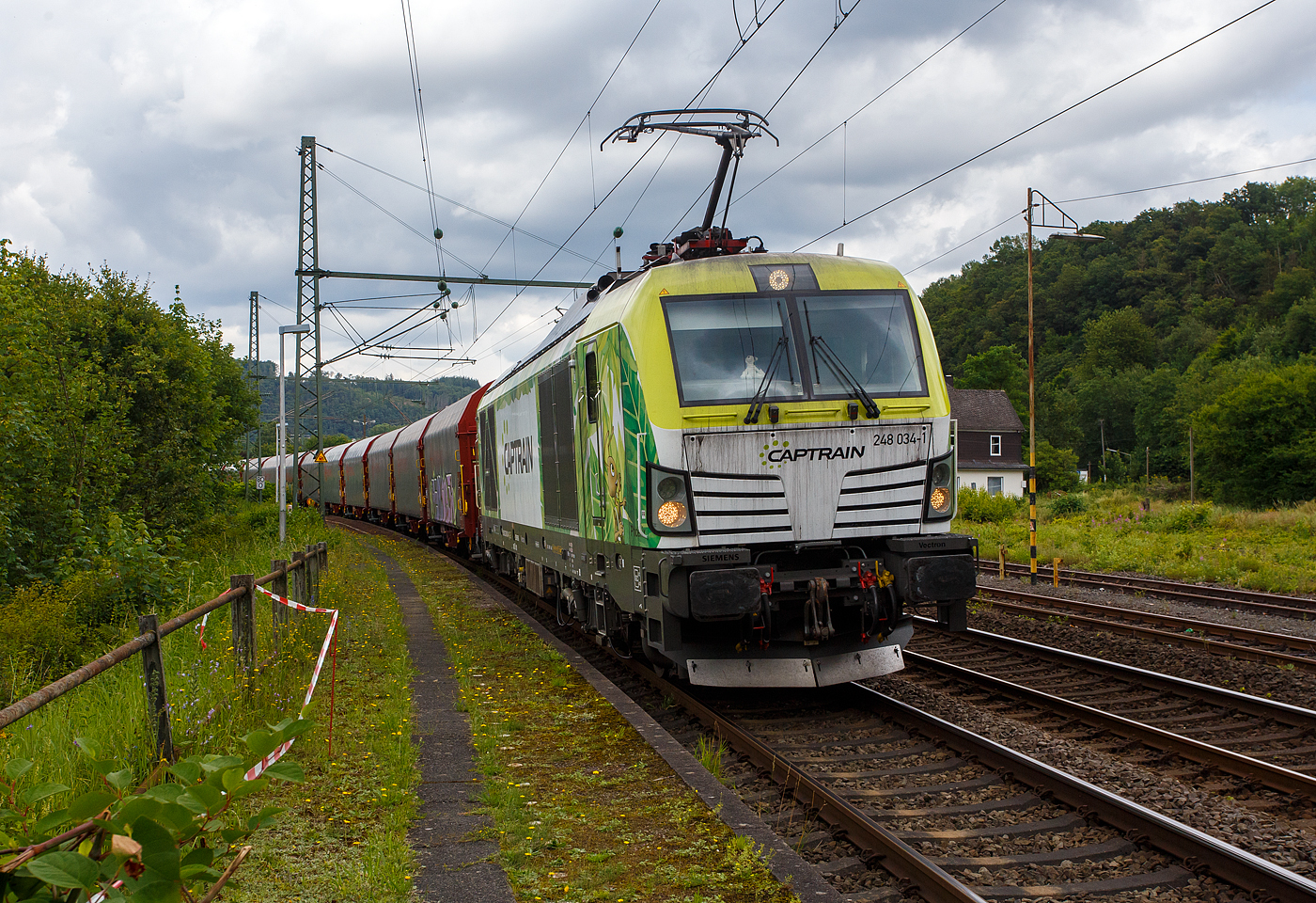 Die an die Dortmunder Eisenbahn GmbH (DE) vermietete SIEMENS Vectron Dual Mode 248 034-1  Phoenix  (90 80 2248 034-1 D-DE) der Captrain Deutschland GmbH fährt am 01 Juli 2024, mit einem Coilzug (Wagen der Gattung Shimmnis-ttu der Ermewa) durch Scheuerfeld/Sieg in Richtung Köln. 

Die SIEMENS Vectron DM wurde 2022 von Siemens Mobility GmbH in München-Allach unter der Fabriknummer 23185 gebaut und im Februar 2023 an die Captrain ausgeliefert. Die Lok hat die Zulassung für Deutschland und eine Höchstgeschwindigkeit von 160 km/h. Die Hybridlok (Vectron Dual Mode) kann die Antriebsenergie aus der Fahrleitung beziehen (2.400 kW Leistungen am Rad), oder mittels eines MTU 16V 4000 R84 V16-Zylinder-Dieselmotors (2.400 kW Motorleistung, 2.000 kW Leistungen am Rad) erzeugen.

Die Dortmunder Eisenbahn GmbH (DE) ist eine private Eisenbahngesellschaft aus Dortmund. Die Dortmunder Eisenbahn GmbH ist ein gemeinsames Tochterunternehmen der Dortmunder Hafen GmbH und der Captrain Deutschland GmbH. Sie ist zu 65 Prozent im Besitz der Captrain Deutschland GmbH (deutsche Tochter der SNCF) und 35 Prozent der Anteile hält die Dortmunder Hafen AG. Die DE Infrastruktur GmbH, mit ca. 50 Kilometern Gleislänge, gehört zu 81 Prozent der Dortmunder Hafen AG und zu 19 Prozent der Captrain Deutschland GmbH.