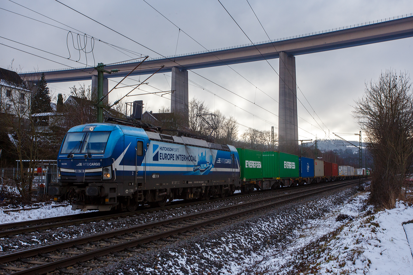 Die an die RTB Cargo vermietete Siemens Vectron MS - 6193 945-3 (91 80 6193 945-3 D-ELOC) der ELL - European Locomotive Leasing (Wien) fährt am 30 Januar 2026 mit einem Containerzug durch Eiserfeld in Richtung Siegen. Im Hintergrund die 105 m hohe Siegtalbrücke der A45 (Sauerlandlinie).

Die SIEMENS Vectron MS - 6.4 MW wurde 2022 von Siemens in München-Allach unter der Fabriknummer 22989 gebaut. Sie ist in der Variante A10-7i ausgeführt und hat so die Zulassungen für Deutschland, Österreich, Polen, Tschechien, Slowakei, Ungarn, Niederlande und Rumänien (D / A / PL / CZ / SK / H / NL und RO).

So besitzt die Variante MS A10 folgende Zugsicherungssysteme: ETCS BaseLine 3, sowie für Deutschland (PZB90 / LZB80 (CIR-ELKE I)), für Österreich (ETCS Level 1 mit Euroloop, ETCS Level 2, PZB90 / LZB80), für Polen (SHP), für Tschechien und die Slowakei (LS (Mirel)), für Ungarn (ETCS Level 1, EVM (Mirel)) für die Niederlande (ETCS Level 1, ETCS Level 2, ATB-EGvV) und für Rumänien (PZB90).
