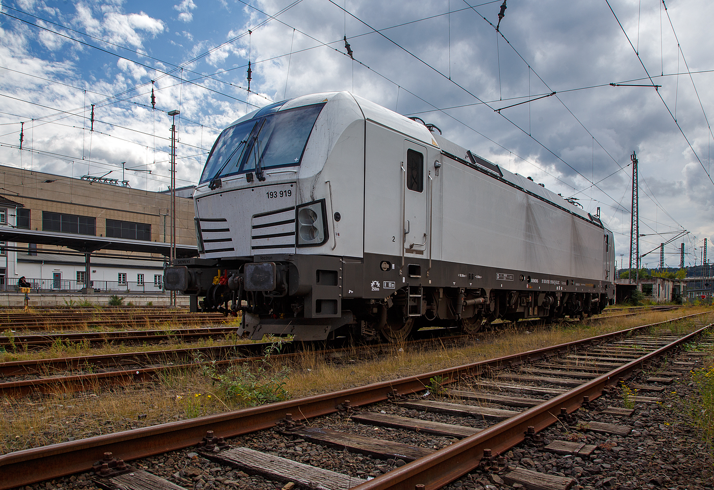 Die an die SETG - Salzburger Eisenbahn TransportLogistik GmbH vermietete weiße SIEMENS Vectron AC DPM 193 919 (91 80 6193 919-8 D-ELOC) der ELL - European Locomotive Leasing ist am 28.08.2023 beim Hbf Siegen abgestellt.

Die SIEMENS Vectron AC DPM mit Diesel Power Modul  bzw. mit LM (Last Mile Diesel) wurde 2022 von Siemens Mobilitiy in München-Allach unter der Fabriknummer 22968 gebaut. Diese Vectron Lokomotive ist als AC DPM – Lokomotive (Wechselstrom-Variante mit Dieselmodul für Rangieren ohne Fahrdraht) mit 6.400 kW konzipiert und zugelassen für Deutschland, Österreich, Bulgarien, Slowakei, Rumänien, Tschechien und Ungarn (D/A/BG/SK/RO/CZ/H), im Dieselbetrieb beträgt die Leistung lediglich 180 kW (160 kW am Rad). 

Diese topmodernen Lokomotiven weisen eine Leistung von 6.400 kW (8.700 PS) auf. Das eingebaute Diesel-Power-Modul ermöglicht das Rangieren ohne Fahrdraht. Zusätzlich sind die Vectron-Lokomotiven von Siemens mit einer Funkfernsteuerung und einer halbautomatischen Bremsprobe ausgerüstet. 

Die Entwicklung der Siemens Lokomotive Vectron basiert auf den Erfahrungen der erfolgreichen EuroSprinter beziehungsweise deren Weiterentwicklung Siemens ES 2007 (NMBS/SNCB-Reihe 18/19) ersetzt. Ausgereifte und bewährte Technik ist mit Flexibilität und Modularität kombiniert. Die Vectron Lokomotive ist für die vielfältigsten Verkehrsaufgaben konzipiert. Ob im nationalen oder grenzüberschreitenden Verkehr, ob im Personen- oder Güterverkehr. Es werden vier elektrische Versionen und eine dieselelektrische Version der Lokomotivplattform angeboten. Die hier gezeigten Vectron Lokomotiven sind als AC – Lokomotiven (Wechselstromlok) mit 6.400 kW Leistung) konzipiert und haben ein Diesel Power Modules (DPM) / Rangiermodul bzw. Last Mile (LM).

Die äußere Gestaltung der Vectron-Lokomotiven unterscheidet sich nur wenig von der der Siemens ES 2007; insbesondere wird das der Crashnorm entsprechende Kopfmodul bis auf einige Detailänderungen, etwa Rückblickkamera statt Seitenfenster, übernommen. Innen ist der neue Typ hingegen komplett anders aufgebaut. Der Maschinenraum besitzt im Gegensatz zur Bombardier TRAXX einen geraden Mittelgang, an dessen Seiten alle Komponenten einen festen Platz haben. In einem unter dem Boden verlaufenden Kanal verlaufen die Steuerleitungen und Druckluftrohre. Die Radsätze werden über gefederte Ritzel-Hohlwellen angetrieben.

Der Vectron unterstützt mit einer optimierten Systemauslegung und vielfältigen Funktionen für energieoptimales Abstellen. Der elektrische Vectron ermöglicht eine erhöhte elektrische Bremskraft von 240 kN. Die rückgewonnene Energie wird hocheffizient für die Versorgung von Hilfsbetrieben genutzt bzw. und wo möglich ins Netz zurückgespeist.

TECHNISCHE DATEN der Vectron AC DPM:
Spurweite: 1.435 mm
Achsformel: Bo'Bo'
Länge über Puffer: 18.980 mm
Drehzapfenabstand: 9.500 mm
Achsabstand im Drehgestell: 3.000 mm
Breite: 3.012 mm
Höhe: 4.248 mm
Raddurchmesser : 1.250 mm (neu) / 1.160 mm (abgenutzt)
Gewicht: 90 t
Spannungssysteme: 15 kV, 16,7 Hz AC (Wechselstrom)
Max. Leistung am Rad: 6.400 kW
Leistungsfaktor: nahe 1
Höchstgeschwindigkeit: 160 km/h
Anfahrzugskraft: 300 kN
Dauerzugkraft: 250 kN
Elektrische Bremskraft: 240 kN
Kraftübertragung: Ritzelhohlwellenantrieb
Lichtraumprofil: UIC 505-1

Leistungsdaten DPM (Diesel Power Modul):
Max. Geschwindigkeit : 40 km/h
Leistung: 180 kW (160 kW am Rad)
Tankvolumen der DPM:  350 l (Diesel)
