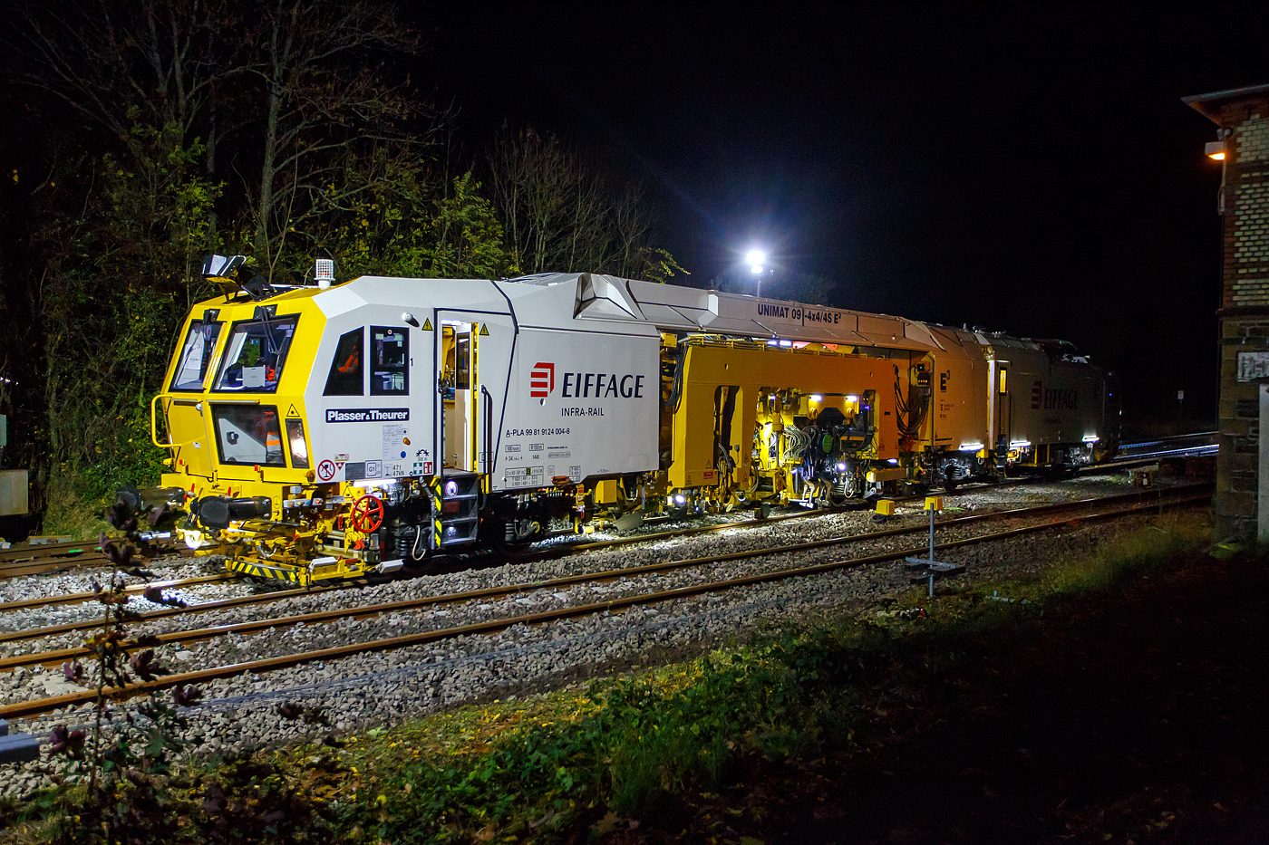 Die Baustelle Bahnhof Herdorf am Abend des 26 Oktober 2025, nun ab 20:40 Uhr wird die neue Weiche 3, beim Bahnhof/Stellwerk Herdorf Fahrdienstleiter (Hf), gestopft. Hier kam die recht neue Plasser & Theurer UNIMAT 09-4x4/4S E� (A-PLA 99 81 9124 004-8), eine Universal-Weichenstopfmaschine mit Hybrid-Antriebstechnik, der Firma Eiffage Infra-Rail GmbH (Herne) zum Einsatz. Ob die Maschine nur von Eiffage Infra-Rail gemietet oder nun gekaut wurde ist mir nicht klar, aber eingestellt ist sie in �sterreich �ber Franz Plasser Vermietung von Bahnbaumaschinen GmbH. 

Die Maschine wurde 2017 von Plasser & Theurer in Linz unter der Fabriknummer 6557/58 gebaut. Diese Maschine mit der neuen E�-Antriebstechnologie von Plasser & Theurer wurde erstmals 2017 auf der iaf 2017 in M�nster pr�sentiert, wo ich sie am 01.06.2017 auch ablichten und sogar in ihr Platz nehmen konnte. Siehe u.a.:
http://hellertal.startbilder.de/bild/oesterreich~bahndienstfahrzeuge~stopfmaschinen/572409/neues-maschinendesign-und-neue-e179-antriebstechnologie-von.html
und
http://hellertal.startbilder.de/bild/oesterreich~bahndienstfahrzeuge~stopfmaschinen/572406/der-blick-des-maschinenfuehrers-auf-das.html

Leider ist die Helltalbahn nicht elektrifiziert, somit konnte die Maschine den Bahnhof Herdorf nur mit Dieselantrieb (diesel-elektrisch) anfahren und nur im Dieselbetrieb arbeiten. Wenn aber eine Oberleitung vorhanden ist, dann kann die Maschine auch rein elektrisch arbeiten. 

Die Fahrantriebe sind elektrisch im Dieselbetrieb diesel-elektrisch. Im Arbeitsmodus werden alle Drehbewegungen elektrisch, Linearbewegungen hydraulisch. Zudem wir im Dieselbetrieb �bersch�ssige elektrische Energie ins Netz zur�ck gespeist. 

Der diesel-elektrisch angetriebener Fahrmodus und Arbeitsmodus:
Ein Dieselmotor mit einer Leistung von 600 kW liefert die Energie f�r die elektrische Versorgung der Antriebskomponenten �ber den Trafo und Stromrichter. Er wirkt dabei als Generator. Im Arbeitsbetrieb funktionieren die Aggregate gleicherma�en wie im elektrischen Modus. Wichtigster Vorteil ist die Reduktion von der CO2-Emission und von L�rm (10 dBA L�rmreduzierung). Weniger Triebstoffverbrauch, h�here Energieeffizienz im Diesel-elektrischen Betrieb. Ich konnte pers�nlich feststellen, dass die Maschine (auch beim Stopfen) erheblich leiser ist, als andere klassische Maschinen. 

TECHNISCHE DATEN:
Fahrzeugbegrenzungsprofil: G1
Spurweite: 1.435 mm (Normalspur)
Anzahl der Achsen: 8 (in 4 Drehgesten)
L�nge �ber Puffer:  34.140 mm
Drehzapfenabst�nde: 11.250 mm / 4.550 mm / 10.300 mm
Achsabstand im Drehgestell: 1.800 mm
Raddurchmesser (neu): 920 mm
Eigengewicht: 142.000 kg
Kleister befahrbarer Gleisbogen: R = 150 m 
Zugelassen f�r Streckenklasse: C2 und h�her
H�chstgeschwindigkeit: 100 km (eigen und geschleppt)
Kraftstofftank: max. 2.580 l (Diesel)
Wirkungsgrad: bis zu 94 %
Bremse:2 x KE-GP mZ (K)
Bremssohle: J 816 M