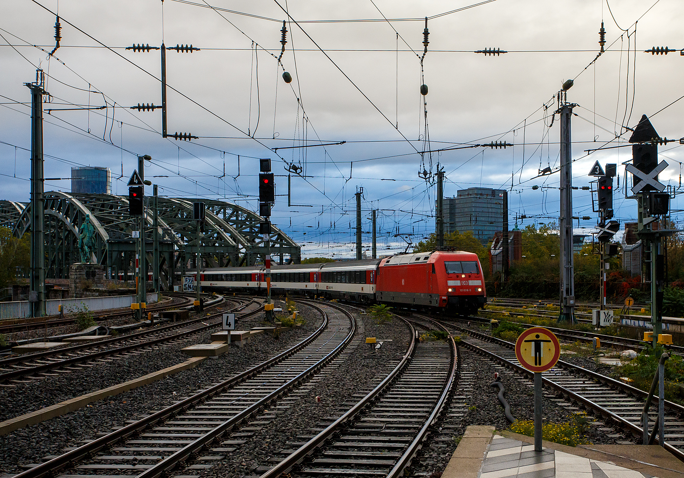 Die DB 101 018-0 (91 80 6101 018-0 D-DB) der DB Fernverkehr AG, kommt am 21 Oktober 2025, mit dem EC 7 (Hamburg-Altona - K�ln - Mainz - Basel SBB) [ehem. weiter �ber Bern nach Interlaken Ost], �ber Hohenzollernbr�cke und erreicht so nun den Hauptbahnhof K�ln. Hinter der DB 101 sind SBB EuroCity-Wagen. Die EuroCity-Wagen (Apm EC und Bpm EC) der SBB sind zwar nach �hnlichen Prinzipien aufgebaut worden, werden aber in der Schweiz nicht als Einheitswagen bezeichnet. Eine Ausnahme ist der eingereihte Speisewagen (WRm 61 85 88-94 113-7 CH-SBB), diese sind Einheitswagen IV. 

Die Lok wurde 1996 von ADtranz (ABB Daimler-Benz Transportation GmbH) in Kassel unter der Fabriknummer 33128 gebaut.

Aufgrund der gro�en Versp�tungen des EC 7 von Hamburg-Altona nach Interlaken Ost und des EC 9 von Dortmund Hbf nach Z�rich HB verkehren beide Linien ab dem 29. April 2025 fahrplanm��ig nur noch bis Basel SBB. Wobei dieser Zug in K�ln p�nktlich war.

F�r den Schweizer Linienabschnitt ab Basel SBB nach Z�rich HB und Interlaken Ost kommen Ersatzz�ge zum Einsatz. Reisende von Deutschland aus dem EC 7 und dem EC 9 in Richtung Schweiz steigen in Basel SBB um. Diese Ma�nahme wurde bei gro�en Versp�tungen bereits in Vergangenheit umgesetzt.

Nicht betroffen sind der EC 6 von Interlaken Ost nach Dortmund Hbf und der EC 8 von Z�rich HB nach Hamburg-Altona. Diese Z�ge verkehren weiterhin grenz�berschreitend.
