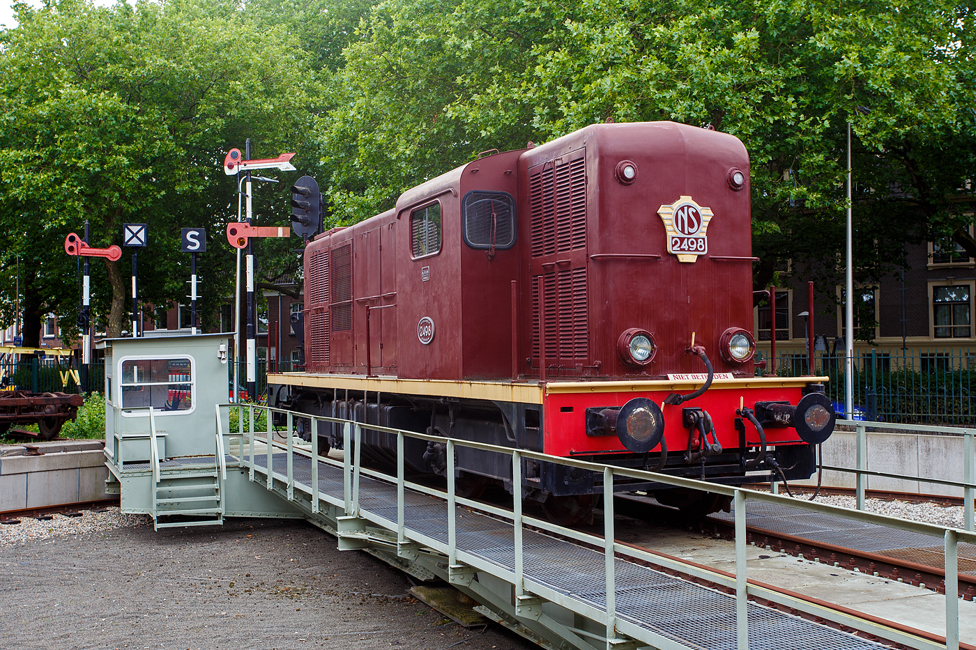 Die Dieselelektrische Lokomotive NS № 2498 der NS-Serie (Baureihe) 2400 am 24 Juni 2025 auf der Drehscheibe im Het Spoorwegmuseum (bis 2005 NSM - Nederlands Spoorwegmuseum / Niederländischen Eisenbahnmuseum) in Utrecht im ehemaligen Bahnhof Maliebaanstation.

Die NS-Baureihe 2400 (2401 – 2530) ist eine Reihe von 130 Stück der leichteren Version dieselelektrischer Lokomotiven, die zwischen 1954 und 1991 von der NS - Nederlandse Spoorwegen (Niederländischen Staatsbahnen, heute Niederländische Eisenbahnen AG), für den Güterverkehr auf Nebenstrecken, eingesetzt wurden. Gebaut wurden die Loks zwischen 1954-1957 (diese 1956) von Alsthom in Belfort in Frankreich. 

Anfang der 1950er Jahre entschied die NS, dass die verbleibenden Dampflokomotiven innerhalb weniger Jahre ersetzt werden müssten. Zu diesem Zweck wurden 280 Diesellokomotiven bestellt, die, aufgeteilt auf die Baureihen NS 2200 und die leichtere NS 2400, dazu beitrugen, dass im Januar 1958 die letzte Dampflokomotive außer Betrieb genommen werden konnte. 

Es wurden Lokomotiven in bewährter Bauart angeschafft. 130 Lokomotiven (Baureihe 2400) wurden bei Alsthom in Frankreich bestellt und weitere 150 Lokomotiven amerikanischer Bauart (Baureihe 2200) bei verschiedenen Herstellern in den Niederlanden und Frankreich.

Die Serie 2400 wurde nicht speziell für die NS entwickelt. Lokomotiven dieses Modells wurden bereits in den 1950er Jahren von Alsthom im französischen Belfort an Eisenbahnen in den damaligen französischen Kolonien und in eine Reihe anderer Länder geliefert. Die 2401-2530 wurden zwischen 1954 und 1957 gebaut. Im gleichen Zeitraum wurde auch die Serie 2200 ausgeliefert.

Von 1954 bis 1991 verkehrten sie von Zwolle im Norden des Landes aus, zunächst auch für Personenzüge, später nur noch für Güterzüge. 1976 wurden sieben Lokomotiven an den Bauunternehmer Volkers für den Bau eines Handelshafens in Saudi-Arabien verkauft. Ab 1980 befanden sich alle 113 verbliebenen Lokomotiven im Depot in Zwolle. Die Lokomotiven konnten auch in Mehrfachtraktion verkehren, zunächst mit zwei Lokomotiven, ab 1970 waren jedoch auch drei Lokomotiven üblich.

In den Jahren 1982 und 1983 wurden die ersten 22 Lokomotiven wegen abgelaufener Überholungsfrist ausgemustert, darunter auch die 2498. Die restlichen folgten von 1987 bis 1991. Im Jahr 1985 wurde die 2498 für die Aufstellung im NINT in Amsterdam (Nemo Science Museum Amsterdam) vorbereitet, die Lokomotive war jedoch noch immer eine Nummer zu groß.

Am 10. Dezember 1987 wurde die 2498 dem Nederlands Spoorwegmuseum übergeben. 1992 wurde die Lokomotive in Tilburg wieder mit einer Motoranlage ausgestattet, die nach ihrer Abstellung entfernt worden war. Schließlich ging der 2498 Anfang 2009 zurück zum Überholungsbetrieb nach Tilburg, um braun neu lackiert zu werden. Die Lokomotive ist jedoch nicht im Betrieb.

Die 2530 „Bisschop“ (Bischof):
Da die Sicht aus dem Führerstand einer 2400 insbesondere im Zugbetrieb nicht besonders gut war, wurde die letzte, 1957 ausgelieferte Lokomotive probeweise mit niedrigeren Motorhauben und einem anderen (Mittel-)Führerstand ausgestattet. Der Führerstand ist höher und länger und bietet besseren Komfort und bessere Sicht als bei den Serienmodelle. Die 2530 wurde in einer anderen Farbe in Dienst gestellt: Lila mit schwarzem Fahrgestell, was der Lokomotive den Spitznamen „der Bischof“ einbrachte. Diese besondere Farbe wurde von der Frau des Präsidenten der NS Franciscus Querien (Frans) den Hollander ausgewählt. Im Jahr 1963 erhielt die Lokomotive, wie auch die übrige Serie, einen rotbraunen Anstrich. Der Lokführer hat tatsächlich eine viel bessere Sicht und aus diesem Grund wurde die Lokomotive oft an der Spitze von Arbeitszügen eingesetzt, insbesondere 1964 bis 1989 beim „Unkrautbekämpfungszug“. 

Allgemeiner Aufbau:
Alsthom baute die gesamte Lokomotive nach dem Aufbau einer Rangierlokomotive mit zwei Hauben, die den Motor und die verschiedenen Geräte umschließen und durch einen Führerstand mit der gleichen Höhe wie die Hauben getrennt sind.

Bei dem von SACM, Mulhouse (Société alsacienne de constructions mécaniques, früher auch Elsässische Maschinenbau-Gesellschaft Grafenstaden) gelieferten Motor handelt es sich um den Typ MGO V12. Es ist ein V12-Zylinder 4-Takt Dieselmotor mit Turbolader und Ladeluftkühler, diese Motoren kamen in Frankreich unter anderem in der CC 65000 und einigen BB 63500 zum Einsatz. Mit einer Leistung von 625 kW (850 PS) treibt der Dieselmotor einen Generator an, der die vier Fahrmotoren (einen für jede Achse) mit Gleichstrom mit einer Spannung von 1,5 kV versorgt. Die Lokomotiven mit einem Gesamtgewicht von 60 t sind auf 80 km/h begrenzt. Sie können in Mehrfacheinheiten aus zwei Lokomotiven eingesetzt werden, deren Anzahl auf drei und dann auf vier erhöht werden kann. Einige Lokomotiven sind mit einem dritten Spitzensignal ausgestattet, um den Betrieb auf den deutschen Grenzstrecken zu ermöglichen, wo diese Ausrüstung vorgeschrieben ist. Aufgrund der Bauweise der Lokomotive hat der Lokführer keine gute Sicht auf die Gleise. 

TECHNISCHE DATEN:
Hersteller: Alsthom, Belfort (Frankreich)
Gebaute Anzahl: 130 (NS 2401 bis 2530)
Baujahre: 1954–1957 
Ausmusterung: 1991
Spurweite: 1.435 mm (Normalspur)
Achsfolge: Bo'Bo'
Länge über Puffer: 12.520 mm (2530: 13,3 m)
Max. Breite: 2.900 mm
Höhe: 3.800 mm
Drehzapfenabstand: 6.800 mm
Achsabstand im Drehgestell: 2.400 mm
Treibraddurchmesser: 1.000 mm (neu)
Dienstgewicht: 60 t
Dieselmotor: SACM V12-Zylinder 4-Takt Dieselmotor mit Turbolader und Ladeluftkühler vom Typ MGO V12
Dieselmotorleistung: 625 kW (850 PS) bei 1.500 U/min.
Motorhubraum: 52 Liter (Ø 175 mm x 180 mm Hub)
Generator:  Alsthom GP 830 A mit einer Leistung von 672 kW (730 V, 920 A)
Fahrmotoren: 4 Stück Alsthom TA 637 VF (1,5 kV)
Leistung der Fahrmotoren: 4 x 168 kW = 672 kW 
Getriebeübersetzung: 15:78
Antrieb: SLM-Universalantrieb
Höchstgeschwindigkeit: 80 km/h 
Anfahrzugkraft: 161,8 kN
Max. Tankinhalt: 3.100 Liter 
Kleister befahrbarer Gleisbogen: R 80 m
