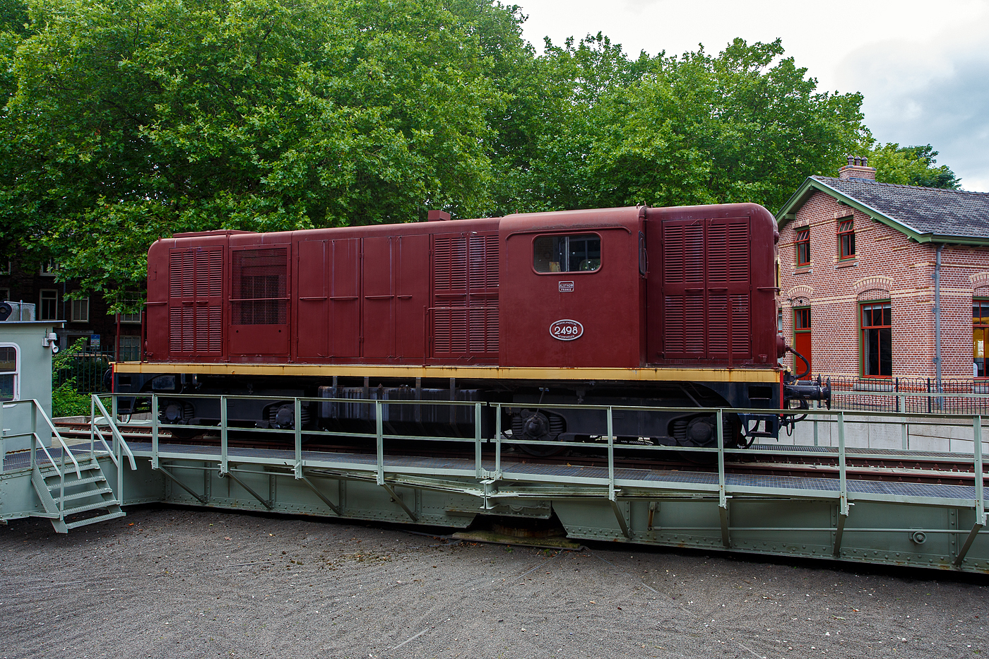 Die Dieselelektrische Lokomotive NS № 2498 der NS-Serie (Baureihe) 2400 am 24 Juni 2025 auf der Drehscheibe im Het Spoorwegmuseum (bis 2005 NSM - Nederlands Spoorwegmuseum / Niederländischen Eisenbahnmuseum) in Utrecht im ehemaligen Bahnhof Maliebaanstation.

Die NS-Baureihe 2400 (2401 – 2530) ist eine Reihe von 130 Stück der leichteren Version dieselelektrischer Lokomotiven, die zwischen 1954 und 1991 von der NS - Nederlandse Spoorwegen (Niederländischen Staatsbahnen, heute Niederländische Eisenbahnen AG), für den Güterverkehr auf Nebenstrecken, eingesetzt wurden. Gebaut wurden die Loks zwischen 1954-1957 (diese 1956) von Alsthom in Belfort in Frankreich. 

Anfang der 1950er Jahre entschied die NS, dass die verbleibenden Dampflokomotiven innerhalb weniger Jahre ersetzt werden müssten. Zu diesem Zweck wurden 280 Diesellokomotiven bestellt, die, aufgeteilt auf die Baureihen NS 2200 und die leichtere NS 2400, dazu beitrugen, dass im Januar 1958 die letzte Dampflokomotive außer Betrieb genommen werden konnte. 

Es wurden Lokomotiven in bewährter Bauart angeschafft. 130 Lokomotiven (Baureihe 2400) wurden bei Alsthom in Frankreich bestellt und weitere 150 Lokomotiven amerikanischer Bauart (Baureihe 2200) bei verschiedenen Herstellern in den Niederlanden und Frankreich.

Die Serie 2400 wurde nicht speziell für die NS entwickelt. Lokomotiven dieses Modells wurden bereits in den 1950er Jahren von Alsthom im französischen Belfort an Eisenbahnen in den damaligen französischen Kolonien und in eine Reihe anderer Länder geliefert. Die 2401-2530 wurden zwischen 1954 und 1957 gebaut. Im gleichen Zeitraum wurde auch die Serie 2200 ausgeliefert.

Von 1954 bis 1991 verkehrten sie von Zwolle im Norden des Landes aus, zunächst auch für Personenzüge, später nur noch für Güterzüge. 1976 wurden sieben Lokomotiven an den Bauunternehmer Volkers für den Bau eines Handelshafens in Saudi-Arabien verkauft. Ab 1980 befanden sich alle 113 verbliebenen Lokomotiven im Depot in Zwolle. Die Lokomotiven konnten auch in Mehrfachtraktion verkehren, zunächst mit zwei Lokomotiven, ab 1970 waren jedoch auch drei Lokomotiven üblich.

In den Jahren 1982 und 1983 wurden die ersten 22 Lokomotiven wegen abgelaufener Überholungsfrist ausgemustert, darunter auch die 2498. Die restlichen folgten von 1987 bis 1991. Im Jahr 1985 wurde die 2498 für die Aufstellung im NINT in Amsterdam (Nemo Science Museum Amsterdam) vorbereitet, die Lokomotive war jedoch noch immer eine Nummer zu groß.

Am 10. Dezember 1987 wurde die 2498 dem Nederlands Spoorwegmuseum übergeben. 1992 wurde die Lokomotive in Tilburg wieder mit einer Motoranlage ausgestattet, die nach ihrer Abstellung entfernt worden war. Schließlich ging der 2498 Anfang 2009 zurück zum Überholungsbetrieb nach Tilburg, um braun neu lackiert zu werden. Die Lokomotive ist jedoch nicht im Betrieb.

Die 2530 „Bisschop“ (Bischof):
Da die Sicht aus dem Führerstand einer 2400 insbesondere im Zugbetrieb nicht besonders gut war, wurde die letzte, 1957 ausgelieferte Lokomotive probeweise mit niedrigeren Motorhauben und einem anderen (Mittel-)Führerstand ausgestattet. Der Führerstand ist höher und länger und bietet besseren Komfort und bessere Sicht als bei den Serienmodelle. Die 2530 wurde in einer anderen Farbe in Dienst gestellt: Lila mit schwarzem Fahrgestell, was der Lokomotive den Spitznamen „der Bischof“ einbrachte. Diese besondere Farbe wurde von der Frau des Präsidenten der NS Franciscus Querien (Frans) den Hollander ausgewählt. Im Jahr 1963 erhielt die Lokomotive, wie auch die übrige Serie, einen rotbraunen Anstrich. Der Lokführer hat tatsächlich eine viel bessere Sicht und aus diesem Grund wurde die Lokomotive oft an der Spitze von Arbeitszügen eingesetzt, insbesondere 1964 bis 1989 beim „Unkrautbekämpfungszug“. 

Allgemeiner Aufbau:
Alsthom baute die gesamte Lokomotive nach dem Aufbau einer Rangierlokomotive mit zwei Hauben, die den Motor und die verschiedenen Geräte umschließen und durch einen Führerstand mit der gleichen Höhe wie die Hauben getrennt sind.

Bei dem von SACM, Mulhouse (Société alsacienne de constructions mécaniques, früher auch Elsässische Maschinenbau-Gesellschaft Grafenstaden) gelieferten Motor handelt es sich um den Typ MGO V12. Es ist ein V12-Zylinder 4-Takt Dieselmotor mit Turbolader und Ladeluftkühler, diese Motoren kamen in Frankreich unter anderem in der CC 65000 und einigen BB 63500 zum Einsatz. Mit einer Leistung von 625 kW (850 PS) treibt der Dieselmotor einen Generator an, der die vier Fahrmotoren (einen für jede Achse) mit Gleichstrom mit einer Spannung von 1,5 kV versorgt. Die Lokomotiven mit einem Gesamtgewicht von 60 t sind auf 80 km/h begrenzt. Sie können in Mehrfacheinheiten aus zwei Lokomotiven eingesetzt werden, deren Anzahl auf drei und dann auf vier erhöht werden kann. Einige Lokomotiven sind mit einem dritten Spitzensignal ausgestattet, um den Betrieb auf den deutschen Grenzstrecken zu ermöglichen, wo diese Ausrüstung vorgeschrieben ist. Aufgrund der Bauweise der Lokomotive hat der Lokführer keine gute Sicht auf die Gleise. 

TECHNISCHE DATEN:
Hersteller: Alsthom, Belfort (Frankreich)
Gebaute Anzahl: 130 (NS 2401 bis 2530)
Baujahre: 1954–1957 
Ausmusterung: 1991
Spurweite: 1.435 mm (Normalspur)
Achsfolge: Bo'Bo'
Länge über Puffer: 12.520 mm (2530: 13,3 m)
Max. Breite: 2.900 mm
Höhe: 3.800 mm
Drehzapfenabstand: 6.800 mm
Achsabstand im Drehgestell: 2.400 mm
Treibraddurchmesser: 1.000 mm (neu)
Dienstgewicht: 60 t
Dieselmotor: SACM V12-Zylinder 4-Takt Dieselmotor mit Turbolader und Ladeluftkühler vom Typ MGO V12
Dieselmotorleistung: 625 kW (850 PS) bei 1.500 U/min.
Motorhubraum: 52 Liter (Ø 175 mm x 180 mm Hub)
Generator:  Alsthom GP 830 A mit einer Leistung von 672 kW (730 V, 920 A)
Fahrmotoren: 4 Stück Alsthom TA 637 VF (1,5 kV)
Leistung der Fahrmotoren: 4 x 168 kW = 672 kW 
Getriebeübersetzung: 15:78
Antrieb: SLM-Universalantrieb
Höchstgeschwindigkeit: 80 km/h 
Anfahrzugkraft: 161,8 kN
Max. Tankinhalt: 3.100 Liter 
Kleister befahrbarer Gleisbogen: R 80 m
