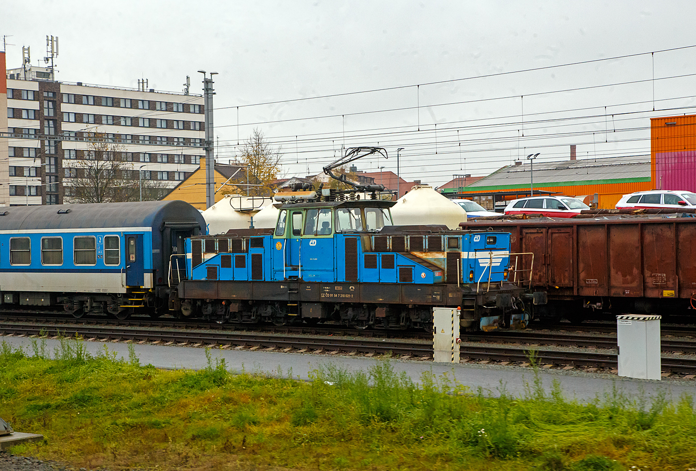 Die elektrische AC-Rangierlokomotive ČD 210 021-2 (CZ ČD 91 54 7 210 021-2) der České dráhy (ČD) steht am 24.11.2022 bei Pilsen (Plzeň) mit einem Personenzug (aufgenommen aus einem alex-Zug).

Die ČD Baureihe 210, ex ČSD-Baureihe S 458.0 (ab 1988 Baureihe 210) ist eine elektrische Rangierlokomotive für 25 kV 50 Hz Wechselstrom.  Sie wurde gleichzeitig mit der Gleichstromlok E 458.0 (heute BR 110) entwickelt, um auf größeren Personen- sowie Güterbahnhöfen den Verschub sowie die Beförderung von Übergabefahrten durchzuführen. Der mechanische Teil ist identisch mit dem der E 458.0, nur im elektrischen Aufbau hat die Lokomotive einen Trafo und eine andere Steuerung. Eine minimale Geschwindigkeit bis zu 5 km/h ist möglich. Die Lokomotiven sind mit einem speziellen Trafo für die Beheizung des Zuges mit 1,5 kV bzw. 3 kV 50 Hz ausgerüstet, und können somit auch im Personenzugdienst eingesetzt werden. Das Übersetzungsverhältnis zwischen Fahrmotorritzel und Großrad beträgt 1:4,055, was der Lokomotive eine Höchstgeschwindigkeit von 80 km/h ermöglicht. Für den Betrieb auf nicht elektrifizierten Streckenteilen besitzt die Lok Akkumulatoren.

TECHNISCHE DATEN:
Gebaute Stück: 74
Spurweite: 1.435 mm (Normalspur)
Achsformel: Bo’Bo’
Länge über Puffer: 14.400 mm
Rahmenlänge:  13.160 mm
Breite: 3.000 mm
Höhe (Pantograph gesenkt):  4.625 mm
Achsstand im Drehgestell : 2.800 mm
Drehzapfenabstand:  6. 300 mm
Treibradraddurchmesser: 1.050 mm (neu) / 980 mm (abgenutzt)
Kleister befahrb. Kurvenradius: R 120 m
Dienstgewicht: 72 t
Max. Achslast : 18 t
Stundenleistung: 984 kW
Dauerleistung: 880 kW
Anfahrzugkraft:  max. 164 kN
Fahrmotoren: 4 Stück Typ TE 006 
Stromsystem: 25 kV 50 Hz AC (Wechselstrom)
