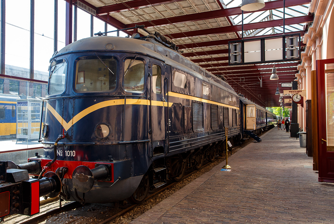 Die Elektrolokomotive NS № 1010 NS-Baureihe 1000 am 29 April 2025 im Het Spoorwegmuseum (bis 2005 NSM - Nederlands Spoorwegmuseum / Niederländischen Eisenbahnmuseum) in Utrecht im ehemaligen Bahnhof Maliebaanstation. Ein Eisenbahnmuseum das zum Verweilen einlädt, leider fehlte uns dieses Mal die Zeit dafür.  

Die NS-Baureihe 1000 war die für das Gleichstromnetz der Niederländischen Staatsbahnen (NS) ausgelegte Version der Wechselstrom-Elektrolokomotive SBB Gotthardlokomotive Ae 4/6 der Schweizerischen Bundesbahnen. Die Fahrzeuge Nr. NS 1001 bis 1003 wurden von der SLM (Schweizerisches Lokomotiv- und Maschinenfabrik) in Winterthur und die Nummern 1004 bis 1010 von der Firma Werkspoor NV (Nederlandsche Fabriek van Werktuigen en Spoorwegmaterieel) in Utrecht produziert. Die elektrische Ausrüstung aller Lok wurde von der Maschinenfabrik Oerlikon (MFO) geliefert.

Ab Sommer 1948 wurden sie zwischen Amsterdam und Eindhoven in Betrieb genommen. Ihre Höchstgeschwindigkeit betrug 160 km/h, die Strecke Amsterdam–Utrecht wurde dafür sogar komplett erneuert. Schnell zeigte sich jedoch, dass die Lokomotiven für 160 km/h nicht geeignet waren. Überhitzte Lager und Haarrisse in den Speichen der Antriebsräder waren die Folge der hohen Geschwindigkeit. Aus diesem Grund wurde die Höchstgeschwindigkeit auf 100 km/h gesenkt, wobei die Schweizer Vorbilder eh nur 125 km/h ausgelegt waren. Ab 1954 bis zur Ausmusterung 1982 wurden sie deshalb fast ausnahmslos im Güterzugdienst eingesetzt. Wie die Originalmuster in der Schweiz waren auch die niederländischen Versionen sehr störanfällig.

Allgemeiner Aufbau:
Der mechanische Teil der Lokomotive wurde von der SLM entworfen. Es handelt sich um eine Rahmenlokomotive, die vier Trieb- und zwei Laufachsen in der Achsfolge (1A)Bo(A1) aufweist. Um die gewünschte Kurvengängigkeit der Lok zu erreichen, wurde jede Laufachse mit der benachbarten Treibachse in ein kombiniertes Drehgestell zusammengefasst, während die beiden mittleren Treibachsen einzeln im Hauptrahen festgelagert sind. Die Laufachsen können jeweils um 2 x 125 und die Drehgestell-Triebachse um je 2 x 6 mm aus ihrer Mittellage ausschwenken (Seitenverschiebbarkeit). Dank dieser Laufwerkanordnung ist es möglich, Kurven mit einem Radius von 110 m bei 30 mm Spurerweiterung noch ohne Zwang zu durchfahren. Bis zu einem Radius von 1.300 m waren 160 km/h möglich.

Wie es auch bei einem gewöhnlichen Drehgestell der Fall ist, dreht sich auch das kombinierte Drehgestell um einen zwischen der Trieb- und Laufachse gelagerten Zapfen. 

Antriebe:
Die Loks hatten den bewährten SLM-Universalantrieb. Jede Treibachse wird durch zwei sich im Lokomotivkasten gegenüberliegende Motoren über ein doppeltes Zahnradgetriebe angetrieben. Die auf den Motorwellen sitzende Zahnritzel sind nicht gefedert. In dem trommelförmigen Antriebszahnrad sind fünf Federelemente eingebaut. 

Als Triebmotoren kamen 8 Stück 6-polige, fremdbelüftete Gleichstrom-Serienmotoren vom Typ 6 MB 620, welche für eine Spannung von 675 V und eine Stundenleistung von 590 PS bei 1.275 U/min ausgelegt wurden, zu Einsatz. Die Kühlluft für je zwei benachbarte Antriebsmotoren wird von einem Radialventilator geliefert, welcher von einem 750 V-Gleichstrommotor von 10 PS Leistung bei 2.400 U/min angetrieben wird. Zwei Ventilatormotoren sind ständig in Reihe geschaltet.

Erhaltenes Exemplar:
Von den zehn hergestellten Exemplaren ist nur eines (dieses) der Nachwelt erhalten geblieben. Die Lokomotive 1010 wurde nach ihrer Ausmusterung in das Eisenbahnmuseum von Utrecht überführt.

TECHNISCHE DATEN:
Spurweite: 1.435 mm
Achsformel: (1A) Bo (A1)
Länge über Puffer: 16.620 mm
Max. Breite: 2.950 mm
Drehzapfenabstand: 8.990 mm
Achsabstand im Drehgestell: 2.600 mm
Achsabstände: 2.600 / 2.230 / 2.230 / 2.230 / 2.600 mm = 11.890 mm
Treibraddurchmesser: 1.550 mm (neu)
Laufraddurchmesser: 1.100 mm (neu)
Dienstgewicht: 100 t
Eigengewicht: mecha. Teil 70,5 t / elektr. Teil 29,1 t
Antriebsmotoren: 8 Stück vom Typ Oerlikon 6 MB 620 mit je 590 PS Leistung
Getriebeübersetzung: 1: 3,56
Antrieb: SLM-Universalantrieb
Höchstgeschwindigkeit: 135 km/h 
Stundenleistung: 3.296 kW (4.480 PS)
Dauerleistung: 2.796 kW (3.800 PS)
Anfahrzugkraft: 177 kN
Stromsystem: 1,5 kV DC
Kleister befahrbarer Gleisbogen: R 110 m

Zum Vergleich (NS 1000 / SBB Ae 4/6) Links zu drei tollen Bildern von Peter Ackermann, der SBB Ae 4/6:
http://igschieneschweiz.startbilder.de/bild/schweiz~e-loks-aeltere-bauarten-und-rangierloks~ae-46-sbb/875212/ae-46-10801-10812-diese-loks-wurden.html

http://igschieneschweiz.startbilder.de/bild/schweiz~e-loks-aeltere-bauarten-und-rangierloks~ae-46-sbb/875209/ae-46-10801-10812-lok-10805-in.html

http://igschieneschweiz.startbilder.de/bild/schweiz~e-loks-aeltere-bauarten-und-rangierloks~ae-46-sbb/875208/ae-46-10801-10812-lok-10805-an.html#tocomment875208

