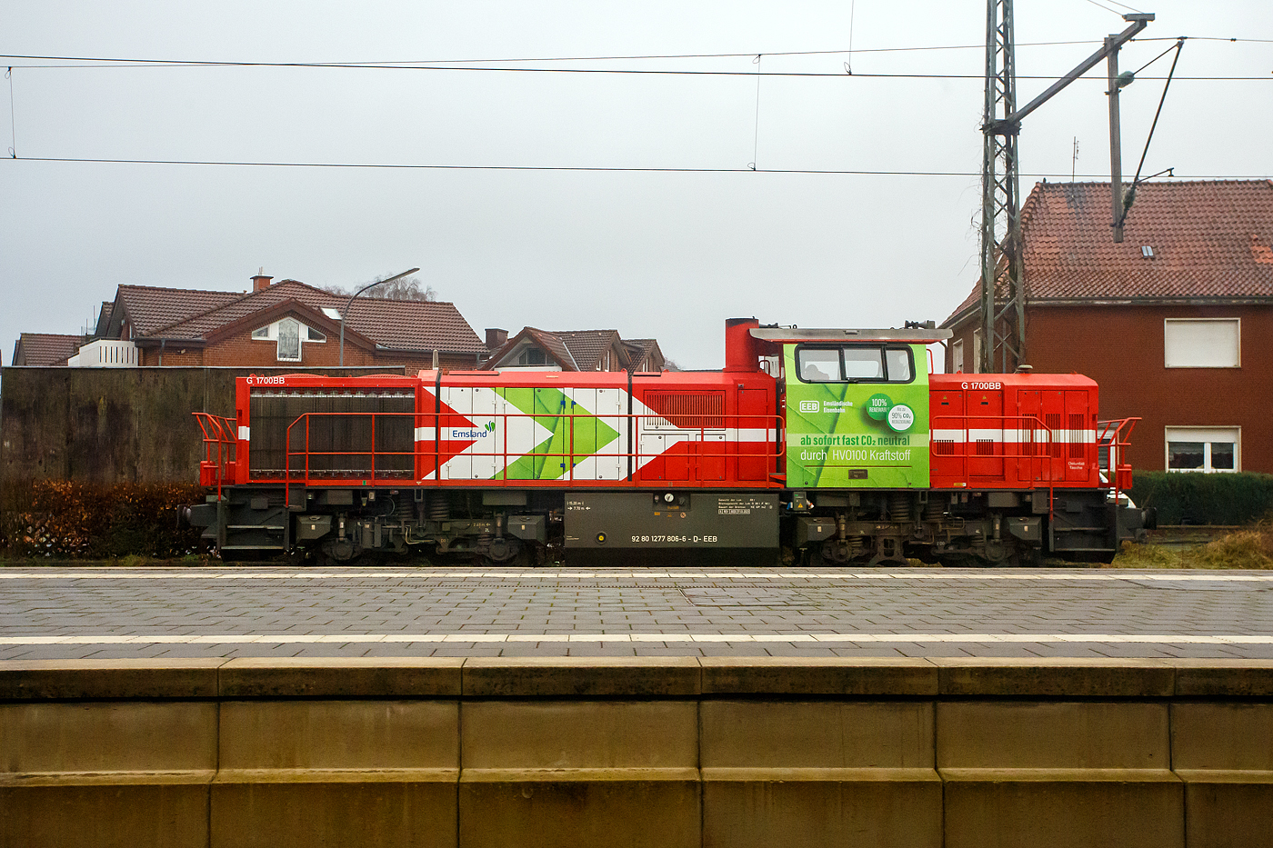 Die Emsland V bzw. 277 806-6 (92 80 1277 806-6 D-EEB) die Vossloh G 1700-2 BB der EEB - Emsländische Eisenbahn GmbH mit Werbung „ab sofort fast CO2 neutral durch HVO 100 Karftstoff“, steht am 14 Februar 2024 beim Bahnhof Meppen (Aufnahme aus einem IC).

Die Lok wurde 2006 von Vossloh in Kiel unter der Fabrik-Nr. 5001594 gebaut und an die HGK - Häfen und Güterverkehr Köln AG in Köln als DH 705 (92 80 1277 806-6 D-HGK) geliefert. Im Februar 2011 ging sie an die EEB - Emsländische Eisenbahn GmbH als Emsland V (92 80 1277 806-6 D-EEB). 

Die Emsländische Eisenbahn (EEB) hat im Oktober 2023 einen Testbetrieb mit einem klimafreundlichen Biokraftstoff gestartet. Der vollsynthetische Biokraftstoff „HVO 100“ soll ein Jahr lang in dieser Lokomotive eingesetzt werden, die normalerweise mit Dieselkraftstoff angetrieben wird. Eine technische Umrüstung der Diesellok ist nicht erforderlich. Der Landkreis unterstützt das Pilotprojekt mit Mitteln aus dem Klimaschutzbudget. Bei geschätzten 200.000 Litern Verbrauch an Dieselkraftstoff im Jahr und einem Mehrpreis von rund 15 Cent pro Liter fallen für den Testzeitraum rund 30.000 Euro Mehrkosten an. Durch den Betrieb mit dem Biokraftstoff können etwa 500 Tonnen CO2 eingespart werden, das sind ca. 90%.

Was ist HVO Diesel?
HVO 100 Diesel ist ein äußerst hochwertiger und klimafreundlicher Hochleistungskraftstoff für Dieselmotoren. Im Gegensatz zu fossilem Dieselkraftstoff wird HVO 100 Diesel aus erneuerbaren Quellen gewonnen und ist damit weitgehend klimaneutral. HVO steht für „hydrotreated vegetable oil“. Es handelt sich also um hydriertes Pflanzenöl aus biologischen Rest- und Abfallstoffen, wie z.B. alte Pflanzenöle, die zum Verzehr nicht mehr geeignet sind. Bei der Hydrierung wird das Pflanzenöl durch eine katalytische Reaktion mit Wasserstoff in Kohlenwasserstoffe umgewandelt und ist aus diesem Grund auch mit herkömmlichen fossilem Diesel in beliebigem Verhältnis mischbar.

HVO 100 Diesel ist nicht zu verwechseln mit dem „Biodiesel“ der ersten Generation, dem Fettsäuremethylester, der bis jetzt zu 7% dem herkömmlichen fossilen Dieselkraftstoff beigemischt wird.

Die Emsländische Eisenbahn GmbH ist ein Eisenbahnunternehmen und Verkehrsunternehmen mit Sitz in Meppen. Sie ist aus einem Eigenbetrieb des Landkreises Emsland hervorgegangen. Dieser war am 1. Januar 1993 durch den Zusammenschluss der Hümmlinger Kreisbahn und der Meppen-Haselünner Eisenbahn entstanden.
