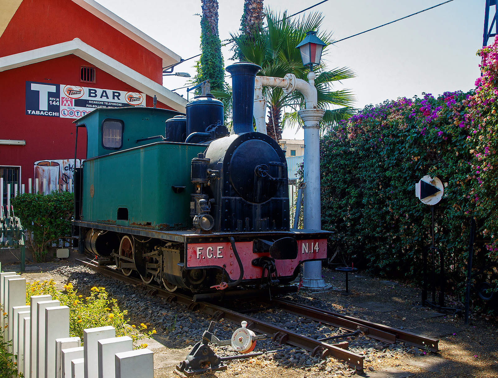 Die F.C.E. N. 14 „LA MEUSE“ der Ferrovia Circumetnea (FCE), ex V 2 der Ferrovia Alifana, steht äußerlich aufgearbeitet, neben einem Wasserkran auf einer Weiche aus der Gründerzeit, neben dem Empfangsgebäude des Bahnhofes Catania-Borgo, hier am 17.07.2022.

Die dreiachsige kohlebefeuerten Schmalspur-Dampflok wurde 1909 von der Société Anonyme des Ateliers de Construction de la Meuse in Liége (Lüttich) unter der Fabriknummer 2224 gebaut und als V 2 an die Ferrovia Alifana in Piedimonte Matese, für ihre 950 mm - Schmalspurbahn von Piedimonte Matese nach Napoli, heute Teil der EAV - Ente Autonomo Volturno S.r.l. (Linie 16). Die Serie bestand aus drei Dampflokomotiven der Gruppo (Gruppe) V 1-3. Die Lok 2 wurde dann 1926 an die Ferrovia Circumetnea (FCE) in Catania verkauft. Bei der Circumetnea sind noch zwei Dampflokomotiven vorhanden, die Nr. 10 (ex. MASCALI) und hier im Bild zu sehende Nr. 14 „LA MEUSE“, ex V 2 der Ferrovia Alifana.

Die 3 belgischen Lokomotiven wurden als Gruppe V 1 bis 3 eingereiht. Sie zeichneten sich durch sehr kleine Räder mit einem Durchmesser von 758 mm (neu) aus. Im Gegensatz zu Circumetnea gab die Ferrovia Alifana ihnen jedoch keinen Namen. Die Lokomotive Nr. 14 ist die einzige der drei, die überlebt hat, und ist als Denkmal im Bahnhof Catania-Borgo ausgestellt. Die anderen beiden Lokomotiven, die Mitte der 1950er Jahre stillgelegt wurden, wurden einige Jahre später abgebrochen.

Die Lokomotiven waren einfach aufgebaute C-Kuppler-Tenderloks (0-3-0 T), mit außenliegenden 2-Zylindern mit Heusinger-Steuerung (oder Walschaerts-Steuerung). Sie waren mit einer Westinghouse-Druckluftbremse und einer Handfeststellbremse ausgestattet.

TECHNISCHE DATEN:
Hersteller: La Meuse in Liége (Lüttich)
Gebaute: 3
Spurweite: 950 mm
Achsfolge: C
Länge: 6.070 mm
Achsabstand: 2 x 1.900 mm = 3.800 mm
Treibraddurchmesser: 758 mm (neu)
Eigengewicht: 17 t
Dienstgewicht: 22 t