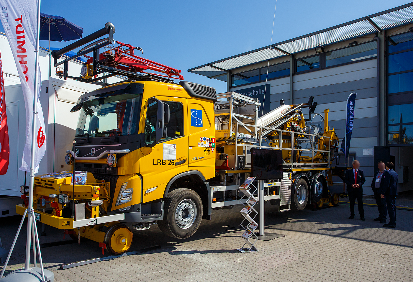 Die Goldschmidt SRS (Smart Rail Solutions) pr�sentierte auf der 29. Internationale Ausstellung Fahrwegtechnik 2025 (iaf) in M�nster (hier am 20 Mai 2025) das bereit im April 2024 an die SPITZKE SE (Gro�beeren) ausgelieferte Zweiwege-Oberleitungsmontagefahrzeug OMF vom Typ LRB26 TC 10-1T2 TS mit Trommelbock, f�r die Fahrleitungsmontage – Oberleitung. Das Fahrzeug ist als Gleisfahrbare Baumaschine Registrier-Nr. G 9931 011 eingestellt. Das Basisfahrzeug/Fahrgestell ist ein Volvo FM 430 Euro 6 (6x2).

Das Zweiwegefahrzeug ist f�r Oberleitungsarbeiten konstruiert und mit einem Goldschmidt hydrostatischen Fahrantrieb f�r Schienen mit drehbarem Eisenbahnfahrgestell f�r den schnellen und einfachen �bergang zwischen Stra�e und Schiene ausgestattet. Auf der Schiene kann man das Fahrzeug von der Kabine oder aus dem Korb bedienen. Das Fahrzeug ist mit einem selbstladenden Trommelgestell ausgestattet. Mit der Teleskop Arbeitsb�hne kann eine Arbeitsh�he von bis zu 13 Metern erreicht werden. Die Spezialfahrzeuge dienen zur Montage von Oberleitungsanlagen der Fern-, Regional- und Industriebahn im Neu- und Umbau. Das OMF ist vom Gleis und vom Planum aus einsetzbar. Ebenso finden die Spezialfahrzeuge Verwendung bei der Montage von Bahnenergieanlagen und beim Verlegen von Kabeln und Leitungen.

Das Fahrzeug verf�gt �ber 3 Achsen (6 x 2), auch auf der Schiene sind es 3, vorne eine und hinten 2 in einem Drehgestell. Der Schienenantrieb erfolgt Hydrostatisch. Das ganze Fahrzeug wird mit dem Schienenantrieb angehoben, die Stra�enr�der sind frei �ber die Schiene angehoben. 

Funktionsmerkmale:
Montage und Demontage von kompletten Oberleitungsanlagen
Montage und Demontage von Bahnenergieanlagen
Wartungs- und Instandhaltungsarbeiten f�r Bestandsanlagen

VORTEILE:
•	Ein- und Ausgleisvorgang in weniger als 2 Minuten
•	Einfaches Eingleisen an 6 Meter breiten Bahn�berg�ngen
•	Eine Neigungskorrektur (TC) der Plattform stellt sicher, dass der Korb immer waagerecht steht, was die Arbeitsbedingungen in Erh�hung erheblich verbessert
•	Das Display im Korb zeigt die Last in Echtzeit, die Position und den zul�ssigen Arbeitsbereich (RTPW) an
•	Selbstladendes Trommelgestell

TECHNISCHE DATEN:
Spurweite: 1.435 mm (Normalspur) 
L�nge �ber Puffer: 11.900 mm
Breite: 2.550 mm (ohne R�ckspiegel)
H�he: 4.000 mm (auf Stra�e) / 4.300 mm (auf den Schienen)
Anzahl der Achsen: je 3 (Stra�e oder Schiene)
Trieb- und Laufraddurchmesser der Schienenr�der: 500 mm (neu)
Dieselmotor: Reihensechszylinder-Dieselmotor vom Typ Volvo D11K430 
Motorleistung: 430 PS (317 kW) bei 1.700 – 1.800 U/min
Max. Drehmoment: 2.050 Nm bei 1000 - 1.400 U/min
Hubraum: 10,8 Liter (Bohrung � 123 mm x 152 mm Hub)
Abgasnorm: Euro 6
H�chstgeschwindigkeit: 90 km/h (Stra�e) / 25 km/h (auf Schiene)
Eigengewicht: 21.800 kg
Max. Nutzlast: 4.200 kg (Trommelbock 2 t, Arbeitskorb 500 kg, Rest Beladung)
	 	 
SPEZIFIKATIONEN DER PLATTFORM:
Hubarbeitsb�hne in Teleskopversion: Typ KLL 10-1T2 mit TC und RTPW 
Korblast 500 kg oder 3 Personen
Korbabmessungen (L x B):  2.000 x 1.100 mm
Arbeitsh�he: 13 m
Neigungskorrektur: 180 mm �berh�hung
Einsatz bis Windgeschwindigkeit: 12,5 m/s
	
Trommelgestell: TB 20 SB, mit hydraulischer Selbstladeeinrichtung 
