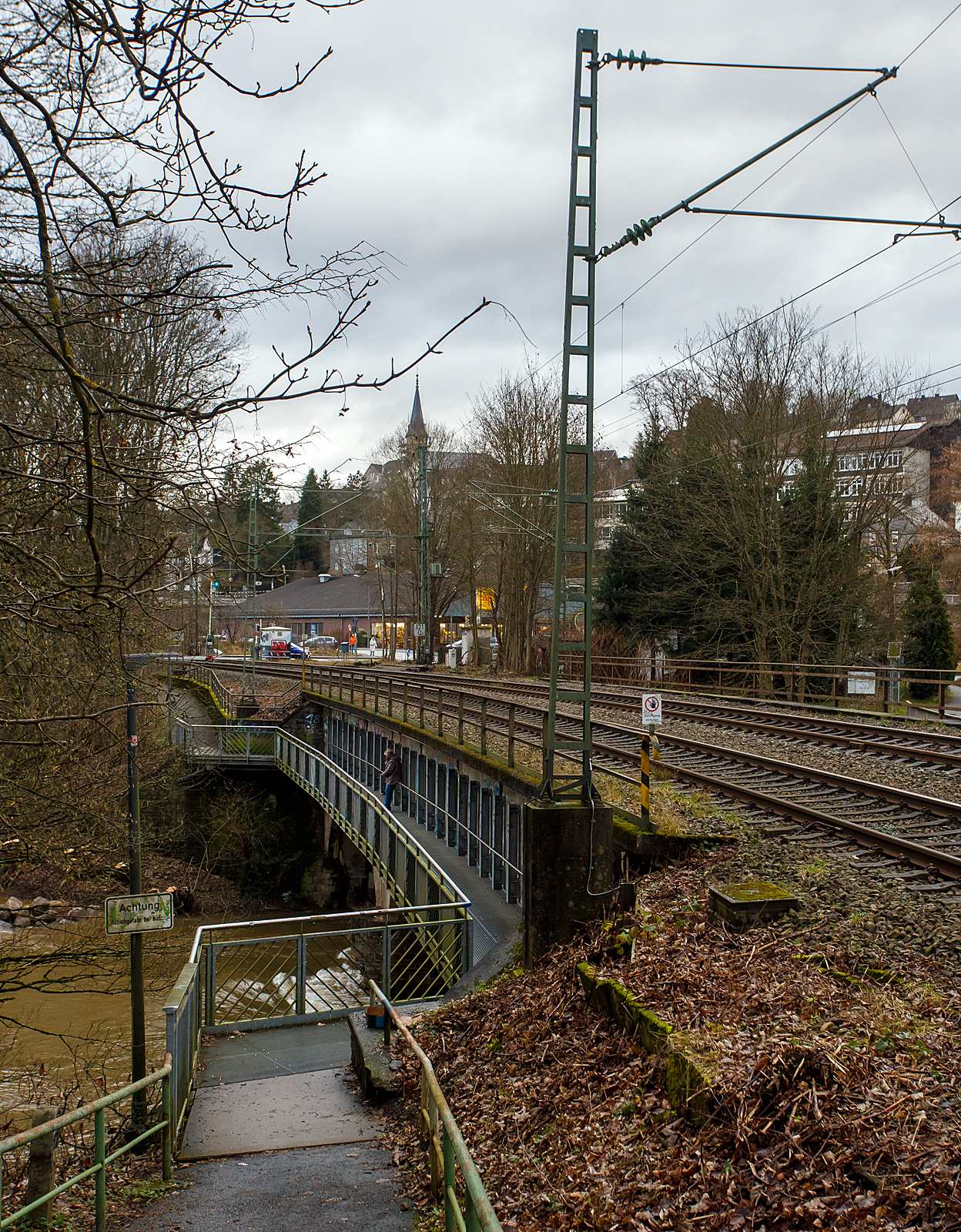 Die vom Hochwasser beschädigte Eisenbahn-Siegbrücke mit Fußgängersteg in Kirchen (Sieg), der Siegstrecke (KBS 460), hier am 03.01.2024.

Die Bahnstrecke Siegen - Köln wird zwischen Kirchen und Betzdorf bis min. Ende nächster Woche gesperrt bleiben. Das hat die Deutsche Bahn Dienstagnachmittag mitgeteilt. Durch das Sieg-Hochwasser gibt es Schäden an einer Eisenbahnbrücke in Kirchen (kurz vorm Bahnhof). Aufgrund der Wetterlage und der weiterhin anhaltenden Regenfälle sei die Sperrung erforderlich, so die Bahn-Pressestelle. Die Züge des RE 9 können wegen der Streckensperrung nur bis Betzdorf fahren. Zwischen Siegen und Kirchen verkehrt die Regionalbahn 90 der Hessischen Landesbahn, leider aber nur wenige und teils mit „kleinen“ LINT 27 Triebwagen. Da wäre wahrhaft mehr möglich und man müsste den SEV nur zwischen Betzdorf und Kirchen betreiben. Aber aufgrund aktuell hoher Krankenstände kommt es auf der Linie RE 9 zudem zu Einschränkungen bis 12.01.2024.

Ich konnte mir den Schaden an einen Brückenpfeiler selbst anschauen (Bilder folgen) und finde die Streckensperrung richtig, darüber ließ ich auch keinen mit Personen besetzten Zug fahren. Was wäre wenn ein Zug darüber fährt und dadurch einbricht. Wer will das verantworten!!! 

Am 29.12.2023 wollten wir mit der Bahn nach Siegen, durch die Reiseauskunft unter www.bahn.de sahen wir bereits das durch wegen einer beschädigten Brücke zwischen Betzdorf (Sieg) und Kirchen (Sieg) ist eine Brücke beschädigt. Die Züge der Linie RE9 aus Richtung Köln enden und beginnen demnach in Betzdorf (Sieg). Die Züge der Linie RE 9 aus Richtung Siegen Hbf enden und beginnen demnach in Kirchen, diese waren aber nicht zu sehen. Bis dahin gab es keine Informationen zur Dauer der Sperrung. Somit fuhren wir mit dem Auto nach Kirchen und fuhren dann mit der RB 90 der HLB (Hessischen Landesbahn) in einem LINT 27, wie die Ölsardinen, nach Siegen Hbf. Auf der Rückfahrt um 14:31 Uhr (ab Siegen) mit RB 90 fuhren wir in einem LINT 41.

Am 30.12.2023 fuhren wir nochmal nach Siegen, das Wetter war besser und unser Ticket war noch gültig. Die Rückfahrt von Siegen machten wir um 13:31 Uhr mit dem HLB RB 90 nach Altenkirchen, dem HLB VT 261 einem LINT 41, dieser war der erste Zug der wieder durchfuhr und die Brücke in langsamer Fahrt befuhr. 

Später hieß es: Die Brücke zwischen Betzdorf und Kirchen ist nach wie vor beschädigt. Die Strecke ist aber wieder befahrbar. Die Züge fahren in dem betroffenen Streckenabschnitt langsamer. Reisende müssen mit Verzögerungen rechnen und sollten ihre Reiseverbindung kurz vor der Abfahrt des Zuges überprüfen.

Nun ist aber der betroffene Streckenabschnitt wieder gesperrt, die Brücke kann nicht mehr befahren werden.