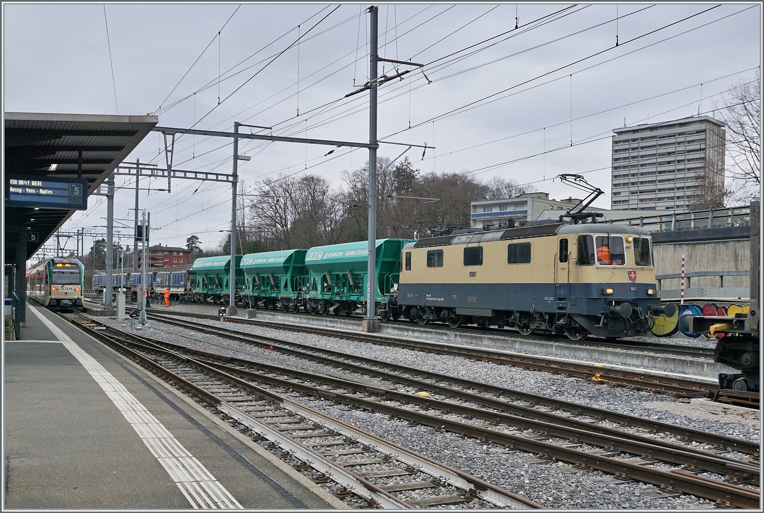Die  IRSI Rheingold Re 4/4 II 11387 (Re 421 387) ist in Morges mit ihrem Kieszug von Gland angekommen und schiebt diesen nun über die Rollbockanlage. 

4. März 2024