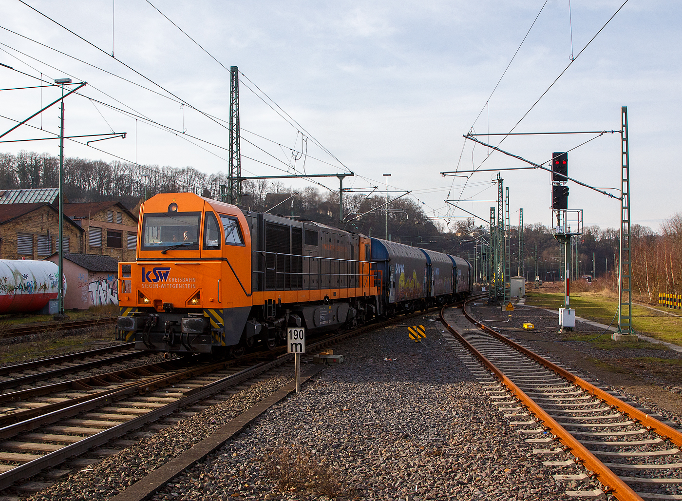 Die KSW 43 (92 80 1273 018-2 D-KSW), die asymmetrische Vossloh G 2000 BB der KSW (Kreisbahn Siegen-Wittgenstein) f�hrt am 09.02.2023, mit ihrem Coilzug (VTG Coilwagen der Gattung Shimmns-ttu), von Betzdorf (Sieg) �ber Siegen, Dillenburg und Haiger nach Herdorf, was einem Umweg von �ber 62 km bedeutet. (Aufnahme vom Bahnsteig 106)

Eigentlich w�rde der Zug hier auf die KBS 462 – Hellertalbahn abbiegen und er w�re in 7,2 km am Ziel. Aber die Hellertalbahn bleibt, nach dem Felssturz am 23.12.2022 in Herdorf bis voraussichtlich zum kleinen Fahrplanwechsel am 09. Juni 2023 gesperrt. Ein weiterer Nachteil ist das die Strecke Haiger – Herdorf nur die Streckenklasse CE hat und zudem sehr Steigungsreich ist. Die 7,2 km lange Strecke Betzdorf – Herdorf hat die Streckenklasse D4, so k�nnen die Coilwagen auch nur abgelastet zugestellt werden.

Nochmal einen lieben Gru� an den netten Lokf�hrer zur�ck.

Zudem habe ich es hier nicht verstanden, warum der KSW-Zug erst auf den Regionalverkehr warten musste bevor es weiter ging. Denn der Zug k�nnte doch ohne Halt durchfahren.
