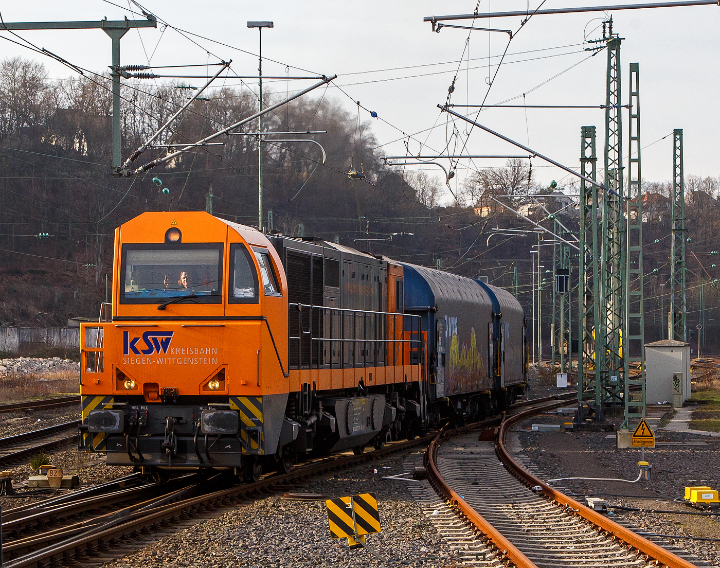 Die KSW 43 (92 80 1273 018-2 D-KSW), die asymmetrische Vossloh G 2000 BB der KSW (Kreisbahn Siegen-Wittgenstein) f�hrt am 09.02.2023, mit ihrem Coilzug (VTG Coilwagen der Gattung Shimmns-ttu), von Betzdorf (Sieg) �ber Siegen, Dillenburg und Haiger nach Herdorf, was einem Umweg von �ber 62 km bedeutet. (Aufnahme vom Bahnsteig 106)

Eigentlich w�rde der Zug hier auf die KBS 462 – Hellertalbahn abbiegen und er w�re in 7,2 km am Ziel. Aber die Hellertalbahn bleibt, nach dem Felssturz am 23.12.2022 in Herdorf bis voraussichtlich zum kleinen Fahrplanwechsel am 09. Juni 2023 gesperrt. Ein weiterer Nachteil ist das die Strecke Haiger – Herdorf nur die Streckenklasse CE hat und zudem sehr Steigungsreich ist. Die 7,2 km lange Strecke Betzdorf – Herdorf hat die Streckenklasse D4, so k�nnen die Coilwagen auch nur abgelastet zugestellt werden.

Nochmal einen lieben Gru� an den netten Lokf�hrer zur�ck.

Zudem habe ich es hier nicht verstanden, warum der KSW-Zug erst auf den Regionalverkehr warten musste bevor es weiter ging. Denn der Zug k�nnte doch ohne Halt durchfahren.
